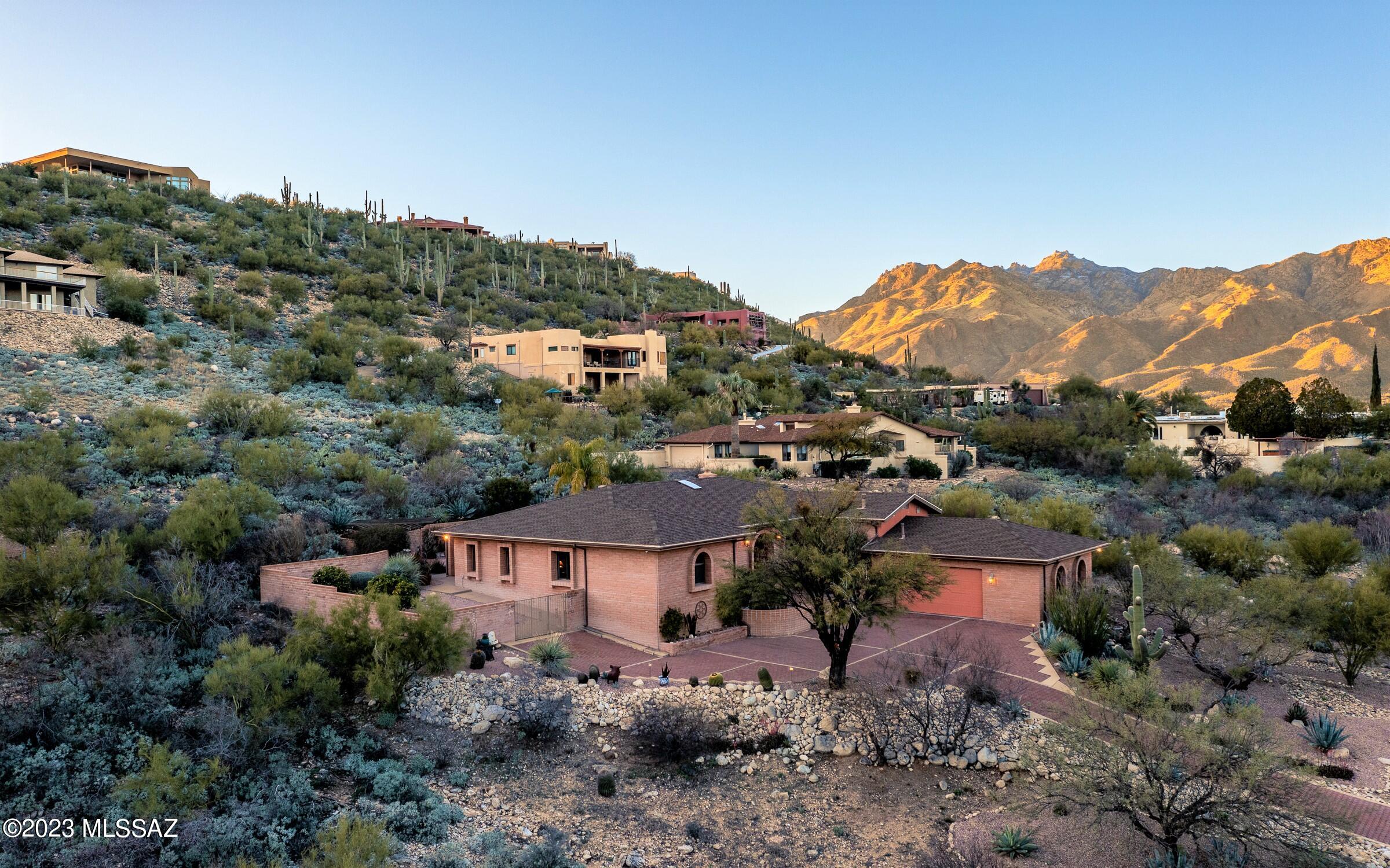 This beautiful custom built masonry home exudes quality from every inch. Located in a gated community on a hillside acre lot & oriented to enjoy wonderful mtn views with a slice of sparkling city lights! It features a Southwest Contemporary architecture that blends well w/Tucson's environment. Arched windows, pitched roof w/varying levels & paver driveway further enhance its appeal. Living space is all on one level w/classic travertine flooring, 4 generous BRs, 2 1/2 baths & oversized 2 car garage. Kitchen has solid cherry wood cabinets w/pull outs, large island & granite counters. The family room picture windows showcase those majestic Mtns, while offering a cozy beehive FP. Primary Bath has a newly remodeled large walk-in tiled shower. Retreat outdoors to a grand backyard oasis. including pool, spa, waterfall and gorgeous mountain views!