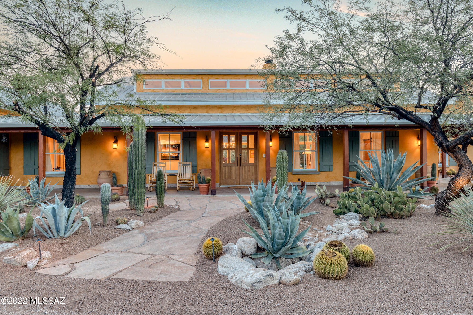 Welcome to Marigold Ranch, a one-of-a-kind property perfectly resting in the
exclusive Tanque Verde Valley.
As you approach this home, your eyes are delighted by the true essence of this
Southern Arizona masterpiece. As Shakespeare is to literature, this home is to
luxury in every aspect. Fashioned after historic, sprawling Texas ranches,
Marigold features a wrap-around porch that brings the desert to your toes.
This home was built with solid block construction walls featuring E-Crete, an
energy-efficient aerated concrete system. The resulting thick exterior walls are
finished with stucco and a natural pigment lime wash, giving a sunny golden-hue
to the exterior. A pitched standing-seam steel roof reminiscent of old ranch
buildings sheds seasonal rains into planting areas around Clerestory windows near the entrance bring more daylight into the interior, along with perimeter upper transom windows and three sets of French doors on the north side. Double-hung windows framed by sage green shutters lend a classic, timeless look to the exterior.

The residence was carefully sited on the three-and-a-half-acre property to avoid disturbing the numerous saguaros and to best-capture the mountain views to the north and east. The grounds are meticulously xeriscaped with unique plantings, relics and sculptures.

Custom Douglas fir double doors greet you as you enter Marigold Ranch and the spectacular floor-to-ceiling double-sided fireplace commands immediate attention. Framed by breathtaking views of the Santa Catalina mountains, this fireplace's style, scale, and charm was inspired by the one in the reading library at the Arizona Inn, a 1930s Spanish Colonial Revival hotel near downtown Tucson. Another prominent feature of the living room area is the set of vintage wooden doors reclaimed from the Tucson Icehouse (circa 1920) that contains the recessed entertainment system. These beautiful features honor our local history with authenticity and anchor the dwelling in Tucson's past.

The craftsmanship of this unique property is showcased through the exposed rough-hewn ceilings and structural beams, which are connected by hand-forged steel bracketry, barrio-style walls, and the solid Montana white pine flooring. The architectural design and flow of the home capture a sense of true peace and tranquility.

The walls feature white hand-troweled diamond plaster, keeping the interior fresh and light. The home has four natural gas fireplaces, creating a wonderfully warm, inviting ambiance - adding comfort to our desert winters. In September 2022, three new HVAC units were installed to keep the house comfortable all year round.

The open kitchen features a tile-clad backsplash with a custom cement range hood, white Calcutta marble across all surfaces - including a Douglas fir island, side pantry, and breakfast nook highlighted with white cabinetry throughout. From the kitchen, one can take their favorite book and a warm beverage to the screened-in porch area to enjoy the morning sunrise.

A wing containing a study and the primary suite angles off one side of the great room, creating a protected courtyard for the north-facing pool terrace. On the opposite side of the great room, another wing includes two guest suites with access to nature's outdoor garden.

Inside and out, this fully furnished and decorated home is filled with many special touches. A mix of contemporary and traditional furnishings and accessories celebrate the colors of the desert and emphasize comfort. The home has two deep Ralph Lauren Home sofas, covered in a hay-colored Manuel Canvas fabric, matching alder-wood low table and sofa bookcase built by local furniture maker Marc Perry, and duck cloth slipcovered armchairs to
anchor the living area.

The pale desert colors of the furnishings and fabrics keep the emphasis on the art. Decorative arts collections, including an assortment of Navajo rugs, antique Indian baskets and pottery, as well as western paintings by California artist Dennis Ziemienski, glasswork by Tom Philibund, and many others, adorn the long
hallways, shelves, and surfaces between the great room and the wings to the east and west.

The thoughtful planning, tasteful eclectic décor, and light-filled layout make this an extremely livable home. Welcome home to Marigold Ranch.
