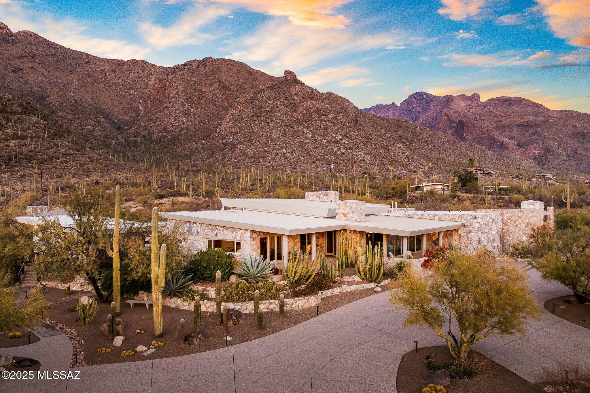 A truly spectacular blend of authentic desert contemporary design and sophisticated modern architecture set on a magical 6.5 acre saguaro studded lot backing to the National Forest. Originally built in 1961 with natural stone quarried from the property, the current stewards of this timeless beauty embarked on a journey to transform and recreate this Frank Lloyd Wright inspired home into a true desert modern masterpiece with none other than Mike Franks, master builder with La Quinta Homes. Armed with exquisite good taste, a dream design team and a healthy budget, the end result is nothing short of amazing. As you enter the private gates and meander up the winding driveway, you are greeted by the most beautiful desert landscaping you've ever seen! The grounds were perfected by Tom Black with Plants of Distinction and showcase some of the most exotic cacti and desert flora which accent the home with vibrant color year round. Natural stone and glass walls are complemented by the use of wood flooring throughout and tongue and groove wood ceilings creating an organic and earthy ambiance. The fusion of the homes simplicity and understated elegance makes for an entertainer's paradise with an open floorplan capturing views from
every window and opening on to deep covered verandas and flagstone patios. To enhance its timeless appeal while preserving its original charm, the property underwent further upgrades in 2021 to include the addition of an art studio/guest house that is unrivaled in Tucson! The natural stone, glass and rusted metal façade blend seamlessly with the main house & features a European designed kitchen, a stunning bathroom w/ handcrafted Zellige tile walls, concrete floors and a workspace that would inspire anyone with its abundant natural light and glass walls that incorporate the beauty of the desert into its modern design. The original stone pool house was also converted to a 1 bed/1 bath guest house that can also serve as a private home office or yoga studio overlooking the pool, beautiful grounds, a new stone Ramada w/fireplace and the dramatic Catalina Mountains & Pima Canyon towering above. With views like this, working from home will prove difficult as your eyes will be drawn to nature and the peaceful surroundings this property affords. Spanning 5,076 sq.ft, the main house features 3 bedrooms & 3 luxurious bathrooms, w/floor to ceiling windows framing views of the city lights and breathtaking sunrises and sunsets. The use of organic
materials creates a seamless connection to the surrounding desert
landscape and the design provides flexible living spaces for guests or creative endeavors. The primary bedroom suite with a private reading area w/fireplace & patio, large walk in closet, sauna and spa like bathroom, embodies comfort and sophistication with a romantic flair. The gourmet kitchen w/honed stone counters, top of the line appliances and large island will leave you speechless, especially after seeing the views from the kitchen sink. The fusion of natural elements and top of the line designer details makes this one of the most beautiful and distinctive homes ever to be offered in Tucson! With its convenient Foothills location - 5 min to Whole Foods or La Encantada, and a stone's throw from Pima Canyon Trailhead, this is truly a rare opportunity to own a piece of Tucson's finest real estate. Horse Property. HOA is Voluntary.