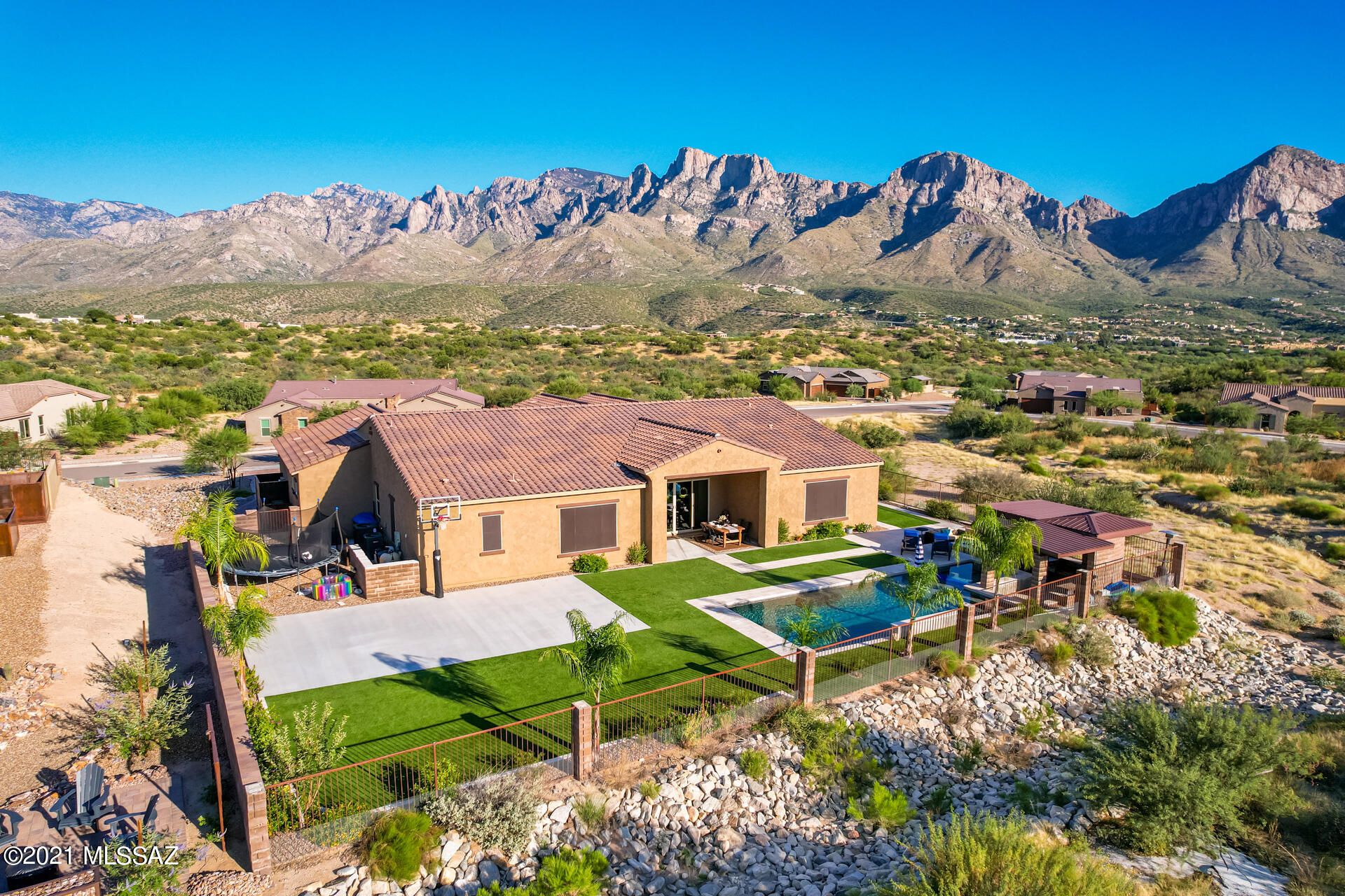 Welcome to one of Oro Valley's most sought after and prestigious gated communities: Sanctuary at Silverhawke.  Nestled on half an acre of lush desert, privacy abounds in this highly upgraded 2-year new home that boasts almost 4300sqft of elegant finishes, soaring ceilings and unobstructed mountain views.  Large entry courtyard showcases the Catalinas and Pusch Ridge and flows to the inside where you enter into a great room that will delight your senses with variegated textures and sumptuous finishes on the walls, stunning light fixtures and a wonderful flow.  

At the heart of the great room is the kitchen arranged around a vast quartz island highlighting double-stacked wall cabinets and a Carrera tile backsplash that climbs to the ceiling.  The gourmand will delight in the Welcome to one of Oro Valley's most sought after and prestigious gated communities: Sanctuary at Silverhawke. Nestled on half an acre of lush desert, privacy abounds in this highly upgraded 2-year new home that boasts almost 4300sqft of elegant finishes, soaring ceilings and unobstructed mountain views. Large entry courtyard showcases the Catalinas and Pusch Ridge and flows to the inside where you enter into a great room that will delight your senses with variegated textures and sumptuous finishes on the walls, stunning light fixtures and a wonderful flow. At the heart of the great room is the kitchen arranged around a vast quartz island highlighting double-stacked wall cabinets and a Carrera tile backsplash that climbs to the ceiling. The gourmand will delight in the professional fridge and freezer, Wolf gas cooktop, double ovens, and easy workflow.  A butler's pantry with ample cabinetry and a built-in icemaker offers passage through a corridor to formal dining room.  Warm hand-scraped wood flooring, custom wainscoting and built-ins with whimsical backsplashes add to the ambience and charm.  Multiple cozy seating areas allow family and guests to be comfortable, whether gathered near the fireplace or seated in the family room to watch a show.  Thoughtful consideration has been given to the use for every space throughout the home.

Private Master Bedroom suite is an oasis for relaxation with stunning mountain views, an oversized spa bathroom with luxurious soaking tub and separate shower with gorgeous tile accents and large walk-in closet. 
 
Designed for multiple generations the generous NextGen suite lies just off the main entrance.  Its spacious living room/rec room features multiple closets  one with W/D hook-ups and a separate bedroom suite with its own walk-in closet and bathroom with mobility friendly shower.    Two additional bedrooms each have their own en-suite provide private luxury for all. The expansive laundry room combines function and beauty with custom built-ins, plentiful storage, and a contemporary tile backsplash.  Nearby 3.5 car garage has plenty of storage and an EV charging station.

The backyard is built to entertain and enjoy!  With no neighbors behind, you can enjoy the privacy and serenity of the desert and panoramic mountain views.  Featuring multiple outdoor living spaces that seamlessly flow from one to another, everyone will find their niche. Artificial turf, travertine pavers, a basketball court, and a large custom swimming pool with shaded sun deck and spa. Swim up to a unique sunken patio adjacent to the pool where the L-shaped ramada incorporates a built-in BBQ, fire pit and dining area, Professional landscaping is just starting to mature and you will enjoy the beauty for years to come! Watch blazing sunsets give way to star-studded skies at the foot of a majestic mountainscape that will continually awe.

Ideally located in Oro Valley, close to shopping, dining, hospitals, and parks, you will love the lifestyle in this quiet gated community.
