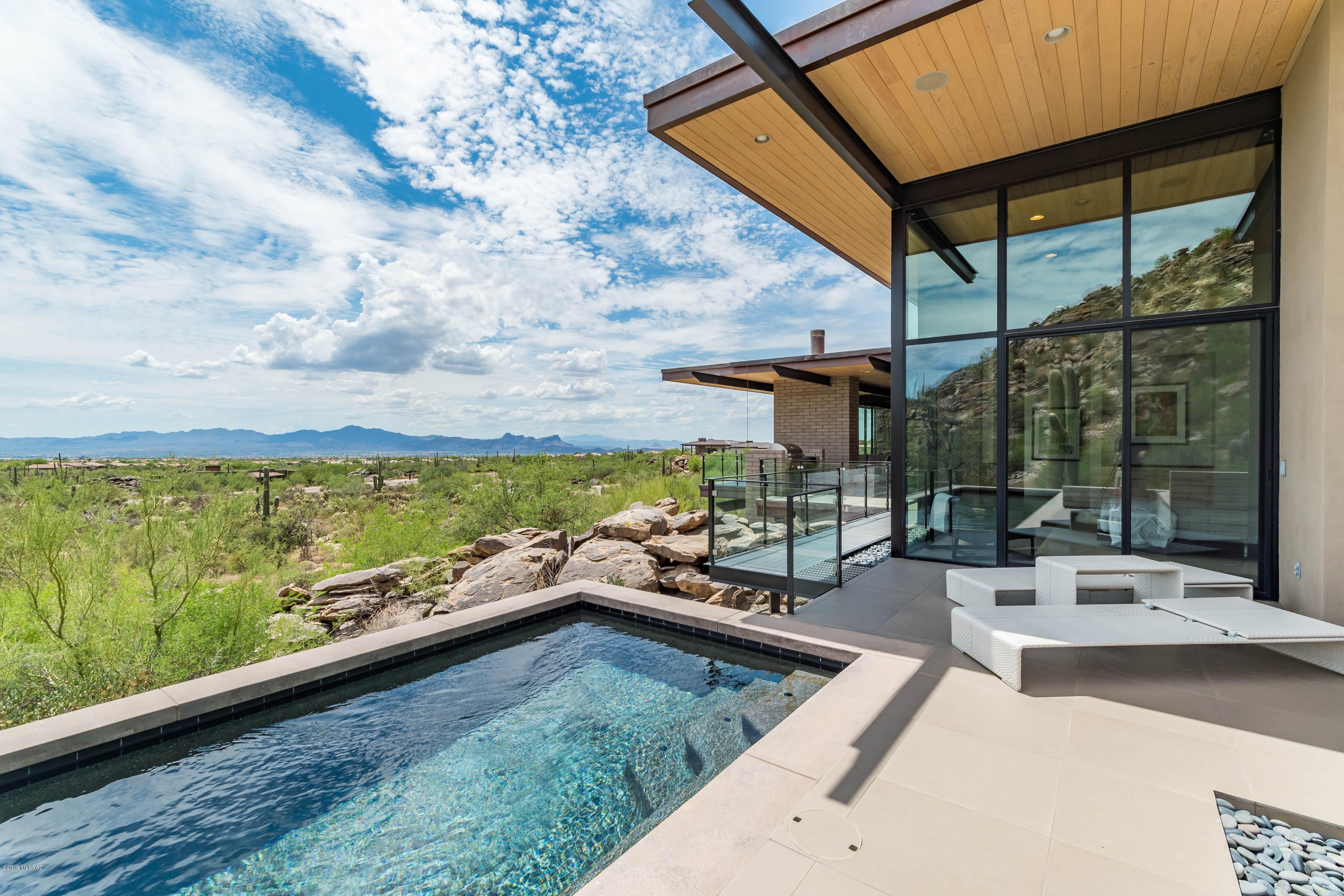An ultra modern glass-ensconced masterpiece - an actual piece of art to live in - with views everywhere! Architect Kevin B Howard meticulously designed all living spaces on the 2nd level, leaving only the garage at ground level, while bringing in modern influences of Frank Lloyd Wright, Mies van der Rohe & Le Corbusier. Very clean lines that integrate with the landscape and capture the mesmerizing Catalina Mountains and city lights. One enters the home from 'underneath' the structure - a unique and stunning  experience. This home maximizes natural light. Inside the home you will find materials such as wood, earth-toned concrete block, gray porcelain tile which flows on the ceilings, walls and floors and continue to the outside.  The open floor plan centers on the stunning  gourmet kitchen. Both the kitchen and adjacent living room use contrasting dark & light tones while splashes of color throughout home come from the owners art collection.  This sprawling home takes advantage of the lovely Arizona climate w/generous outdoor living spaces including a covered loggia with a TV, cooking facility and ample seating for lounging or dining. Just beyond the master bedroom's glass walls are a pool and patio. When waking up in the morning, there is a fabulous view of the sunrise over the Catalina Mountains. It's almost like waking up outdoors - yet comfy and cozy. The master bath is flooded with natural light from large clerestory windows above. Adjacent to the guest bedroom is a large observatory, which was constructed with a retractable roof that allows for optimal stargazing. The space features PlaneWave Instrument's 20-inch reflecting telescope with a mount by Astro-Physics. The desert is truly a part of this glass-ensconced home set into a mountainside.  The home received the AIA Southern Arizona 2015 Citation Award for Architectural Excellence - a very rare award. Home was also featured in LUXE Magazine Arizona Edition Summer of 2014. Copy of LUXE article to read it full in Documents. This home is one of the most specular homes in all of Arizona and could be the most spectacularly designed home in all of Marana/Dove Mountain/Canyon Pass. If you desire an ultra contemporary design - love glass and endless views - love nature & privacy - then call for a private showing of this custom masterpiece. Ive been told that one can see peaks 60 miles away to the south. Come view for yourself - and please view the aerial drone video posted in MLS and YouTube. It's stunning!