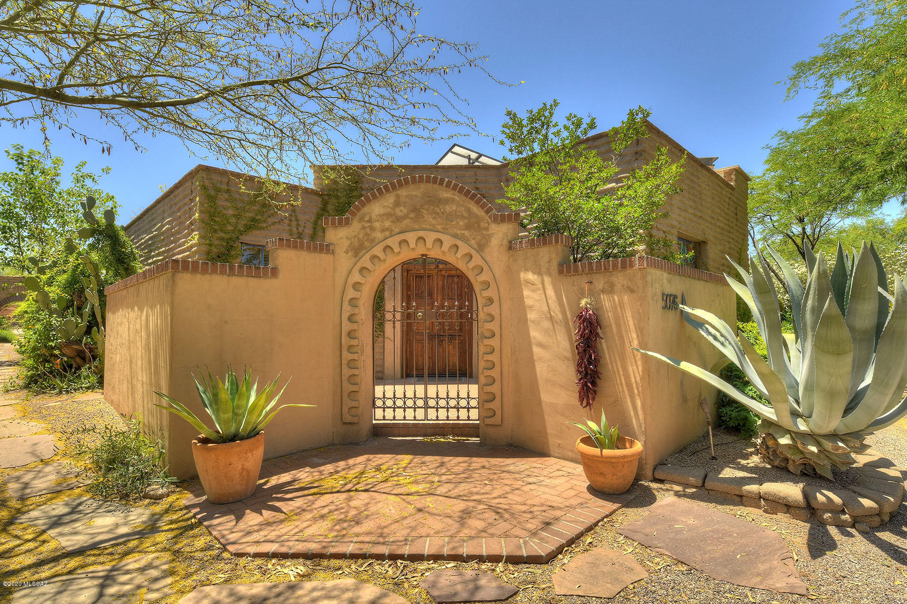Authentic mud adobe hacienda in Ft Lowell Historic District. Tucked away in an enclave of 12 homes amidst a mesquite bosque. This home feels like it is in San Miquel De Allende, Mexico. 3Bd 2Bath. Hi ceilings w/ large viga beams & saguaro ribs thru out. 6 fireplaces-one on patio. Each bdrm has its own fireplace. Trompel'oeil touches thru out. Gourmet kitchen where local renowned chef has entertained, has commercial Wolf stove, sub-zero fridge, farmhouse sink & prep center island 84''x 45'', tile counters, mesquite cabinets & abundant storage. Large great room has triple set tall French doors leading to expansive lush rear yard w/ wall fountain & meditation pond. French doors in Master bdrm suite also open to rear yd. Exceptional design & tile work in master bath. Bedroom 2 & 3 open to small quiet shared patio.  Outdoor kitchen.
Garage has abundant storage and work space.  Courtyard entry.