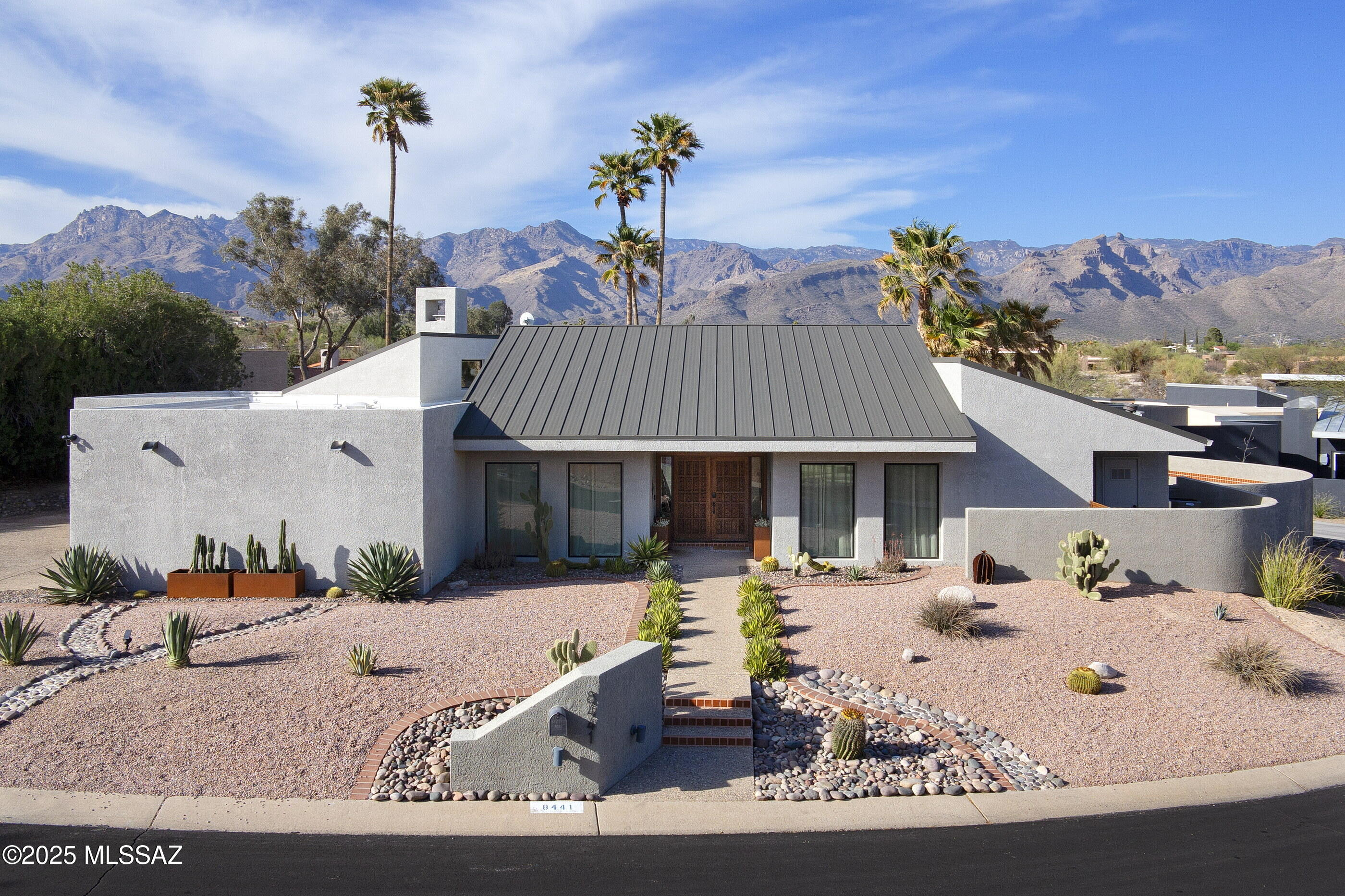 Prepare to be dazzled—and we mean DAZZLED! Designed by architect John Campisano, this stunning 4 bedroom, 3 bath home checks all the boxes—inside and out. All bedrooms have access to outdoor and patio spaces—this home was thoughtfully designed for indoor-outdoor living.  A dramatic sunken living space off the entry with vaulted ceiling and to-the-floor windows is an ideal reading area or game space. With a wall of windows overlooking the back outdoor space, the brand-new kitchen looks like it is out of House Beautiful magazine— soft-close modern Euro cabinetry, concrete counters, handmade Mesquite breakfast bar and floating shelf, coffee station and custom backsplash. Cafe gold-handled appliances which include a gas range with steel hood will thrill the chef in the house —and doi cleanup is a breeze with the large stainless-steel apron sink. The entire kitchen is anchored by a custom oversize kitchen island finished Kintsugi style. The adjacent dining room has a posh mid-century style chandelier, a built-in bar/buffet area is topped by a concrete counter and an artful continuation of the stylish kitchen backsplash tile. Another larger living space off the kitchen features a soaring whitewashed wood ceiling, fireplace, clerestory windows and a modern ceiling fan. 
Self-care, anyone? The primary suite is separated from the rest of the home and is truly a retreat. Prepare to have your mind blown by the bathroom finishesyou won't want to leave! No detail has been sparedthis new bathroom offers mid-century style vanities and lighting, free-form wood framed mirrors, a free-standing soaking tub and an electric wall fireplace. The custom open shower with a river rock waterfall effect seems to spread out and pool into the rest of the space, creating a very natural and cohesive look. This bedroom also offers a soaring ceiling, clerestory windows with electric blinds, built-in journaling desk and a walk-in closet with Sputnik lighting. There are three guest bedrooms, all of which have access to the outdoors. A large bedroom with a walk-in closet and private patio is serviced by a completely renovated hall bath off the main living space. Currently utilized as a gym, this room could also be an ideal home office or guest bedroom. Two matching additional guest bedrooms down a hall share a full hall bath. These bedrooms are connected by catwalk loft areas with custom built airline grade wire rails and an attic space that has been outfitted with a mat flooring. A generous laundry room off the kitchen offers a large sink, cabinets, counterspace and a window. The two-car garage also has a storage roomand the large driveway will accommodate any visitors easily. In addition to the obvious cosmetic improvements, the new owners also heavily invested in the infrastructure of this homenew windows and doors, a new matte metal roof including new gutters and scuppers, whole home in-duct UV air purifier systems, new wood-look ceramic flooring throughout the home, new lighting, fans and much more. Against the backdrop of the Catalina Mountains, the well-designed tiered back outdoor space with desert plantings has grass areas for playtime, pets or just grounding yourself and watching the clouds drift by. Spend sunset in your circular spa and watch the mountains and sky slowly shift to the rich colors the desert Southwest is famous for. A large pool is helmed by a cluster of mature palm trees and offers lots of lounging patio space. The back of the home is lined with covered patio space and an extended paver areaplenty of room to host your guests for year-round entertaining. Get ready to fall in love with this special home!