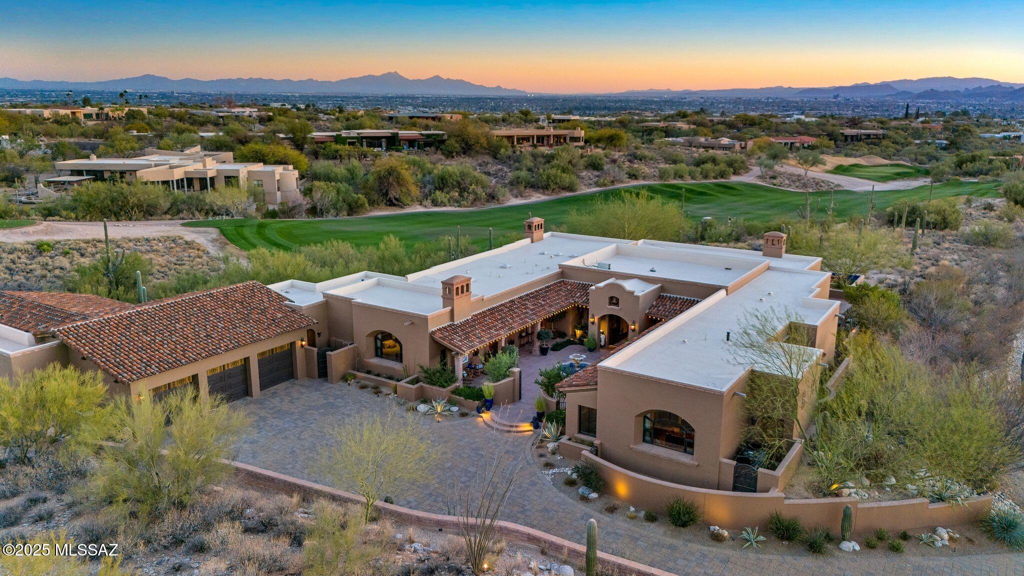 Inspired by world travels, Hacienda De Recuerdos exemplifies the charm and exquisite craftsmanship found in Missions and Haciendas throughout Mexico and Spain.  Set on one of the finest lots in the Catalina Foothills, this 6,300 square foot home has 5 bedrooms plus a guesthouse.  The lot remained protected by the Murphy Trust until Mrs. Murphy's passing in 1997.  It was decidedly the most desirable lot released at her passing for its unobstructed mountain and city views surrounded by open space and golf course on all sides.  The owners then spent the next decade designing and gathering inspiration for what has become the ''Home of Memories''.  
The entry courtyard welcomes you with its Cantera fountain at the center with traditional plantings of Palm (Martyrdom), Cypress (Eternal Life), and Olive (Peace) inspired by the Monastery in Montserrat, Spain.  The custom hand carved front entry doors from Guadalajara are overhung by a bell recovered from Fort Townsend and is an elegant way to announce your arrival.   The Azulejo on the courtyard wall originates from Spain where it was commissioned in Sevilla before finding its home in the courtyard at Hacienda De Recuerdos.

Enter into the large formal living and dining room, allowing your eyes to immediately pass through to the stunning views of the Tucson valley through the 16-foot wall of windows. These windows can vanish into the wall to allow flow from inside to outside.  The large overhead exposed beams are structural, allowing the owners the ability to maximize the ceiling height. 

Before you reach the kitchen, stop by the temperature-controlled 420 bottle wine room noticing the unique vaulted brick ceiling.  Opposite the wine room is the bar with built in beverage fridge and ice maker concealed behind matching cabinet doors.  
The family room and kitchen share space creating an open feel with a unique brick barrel ceiling inspired by those found in Barcelona, Spain.  The kitchen is highly customized with hand carved wood paneling and accents on the island and stove hood and features high end appliances from Sub Zero, Viking Professional, Wolf, and Fisher Paykel.  The primary sink overlooks the golf course. With the additional prep sink on the island there is room for family & friends to help with the holidays in the expansive kitchen. 

Adjacent to the kitchen is the home's laundry room which doubles as a second prep kitchen with a large island, refrigerator and additional dishwasher that is great for catering parties.  In the style of the home, all appliances are hidden by matching cabinet fronts including the washer and dryer.   This space also has a built-in desk and cabinets that line the walls providing ample storage.  From here you have access to the side yard and breezeway to the garage and guest house. 

The living spaces are served by an elegant half bath featuring a special beam and brick ceiling with craftsmanship from across Mexico.  The antique cabinet came from San Miguel De Allende while the copper sink was crafted in Santa Clara Del Cobre.  Like all bathroom tile throughout the home, those featured in this bathroom were imported from Mexico.

A vaulted hallway welcomes you to the spacious master suite that runs along the entry courtyard.  The bedrooms grand window directs your gaze to the Catalina Mountains and Finger Rock.  The suite features beam ceilings and a gas fireplace.  The Master bath is well thought out with separate vanities and two walk in closets with custom closet systems.   The soaking tub and makeup area feature tile reminiscent of the plaster walls at the Alhambra located in Granada Spain.  A pocket door provides privacy in the separate toilet room with a bidet.

The second bedroom in the main house was designed as a guest suite with its own ensuite bath, dual vanities, and large walk-in closet.  There are three additional bedrooms in the main house that can be closed off by a privacy door and currently serve as offices. As you enter the hallway to the guest/office wing you will observe the herringbone brick ceilings and large wood beams.  The custom light fixtures throughout the home were almost exclusively made in Mexico from the owner's designs including those in this hallway.   One office features its own ensuite bath, while the other two share a bath.  Currently closets in bedrooms 4 and 5 are merged to provide a workroom for the office. They could be converted to individual walk-in closets if desired.  El Jefe's office features beamed ceilings and stunning views of the Catalina Mountains though a grand window. 

The guest house has its own entry off the North side of the home and driveway featuring a private patio with a stone cactus fountain and stunning views of the Catalina Mountains.  Enter the guest house to find a lovely living room with a picture window to the mountains and plenty of living space.  The kitchen rivals most homes with ample storage and a large kitchen peninsula.  The generously sized bedroom has views over the golf course.  Your guests may never want to leave.  

The guest house can also be accessed through the garage, making it a short trip into the home. The oversized garage features three individual custom-made garage doors with parking for 3 cars plus space for a golf cart or room for a workout area as currently used. Additionally, there is a large, air-conditioned workshop in the garage, 1 large storage room, and 4 smaller storage closets.  

Access from the garage to the rest of the home is completely flat with no stairs throughout.  Even the backyard features a ramp to the pool level so that the whole home is accessible no matter one's time in life.  The side of the home has a private jacuzzi area that overlooks the golf course.  It also has a yard of artificial turf, great for the dog or a game of bocce ball.

The backyard is a place of tranquility and amazement.  On a clear day you can see multiple mountain ranges looking Southwest all the way to Kitt Peak.  With wide open views, legendary Arizona sunsets abound after a day relaxing by your heated saltwater pool.  The pool is flanked by two stone cactus fountains and multiple lounging areas.   The covered patio starts on the west with a fountain built with reclaimed bricks from Holbrook Arizona and a large sitting area with an outdoor fireplace.   Enjoy al fresco dining while enjoying the twinkling city lights. On the East side of the patio overlooking the golf course is the outdoor kitchen built with the same reclaimed brick featuring a large grill, side stove, sink, and bar seating. 

This one-of-a-kind home is now ready for you to create your own memories.