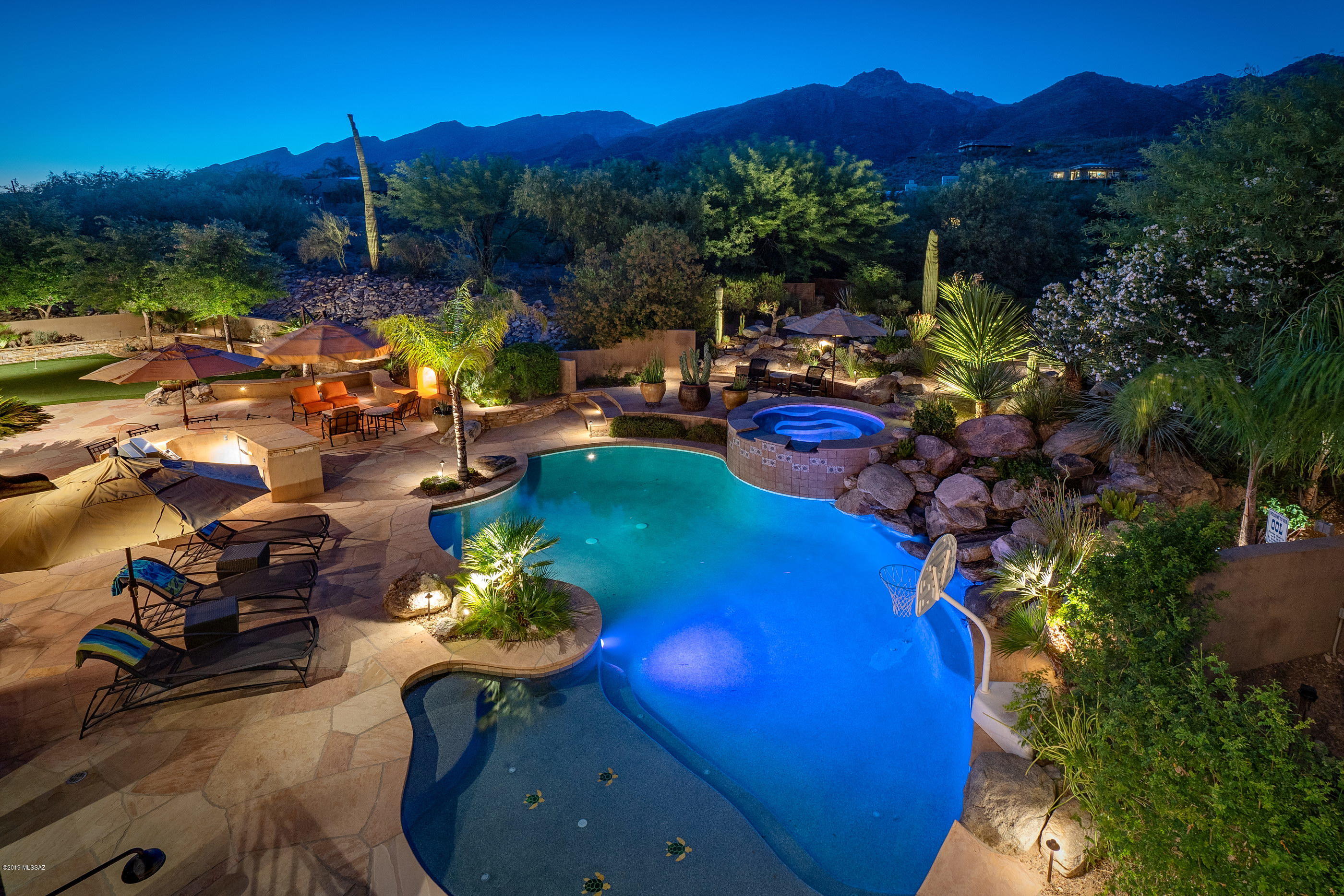 This dramatic hideaway, situated on over an acre, and sited on a North/South axis creates a strong spatial connection between the home and the surrounding landscape. Upon arrival, an air of grandeur pervades this incomparable residence, privately located at the base of the Catalina Mountains and surrounded by sprawling mature desert landscape, adding to the feel of this sophisticated estate. 
Entering the residence, you are greeted by a large foyer with soaring ceilings, acting as the central hall, establishing the main connection point of the home, which opens onto the formal living and dining rooms. Complementing this perfectly executed floor plan, lofty ceilings and French doors open onto the tranquil grounds at every turn. The heart of the home is the fabulous chef's kitchen with gorgeous custom finishes throughout, overlooking the family room, with a fireplace and breakfast dining. 

The main level entertainment (flex) room is designed to substantial scale and comfort, allowing versatility in its use to reflect the activities enjoyed by its owner, while the upper level entertainment space, includes a hand crafted bar, exuding elegance with carved wood cabinetry, granite countertops and a walk-out terrace, overlooking the surrounding verdant gardens and Catalina mountain vistas.

Located on West end of the property is the sumptuously appointed master bedroom, with dressing suite, luxuriously finished master bath and large office/workout space, with one additional bedroom located on the west wing. The balance of four bedrooms are sequestered on the East wing of the residence, each with direct access to an adjoining bath, perfect for families and guests alike. 

An elongated veranda connects the shared living spaces, with a series doors coordinated to tie the interior rooms to the spacious outdoor living environments, resulting in a juxtaposition of private and social spaces. Layers of elevated patios, with various native shrubs cause an explosion of color, light and shadow, creating a framework for the pool and spa, acting as the centerpiece of the rear courtyard. Seamless indoor-outdoor entertaining while out on the sun-drenched terrace, offers al fresco dining, multi-barbecue stations, a putting green with customized green speeds, breaks, fringe and rough, creating the ideal practice surface, all overlooking the resort like pool and spa, with the unobstructed Catalina Mountains beyond.