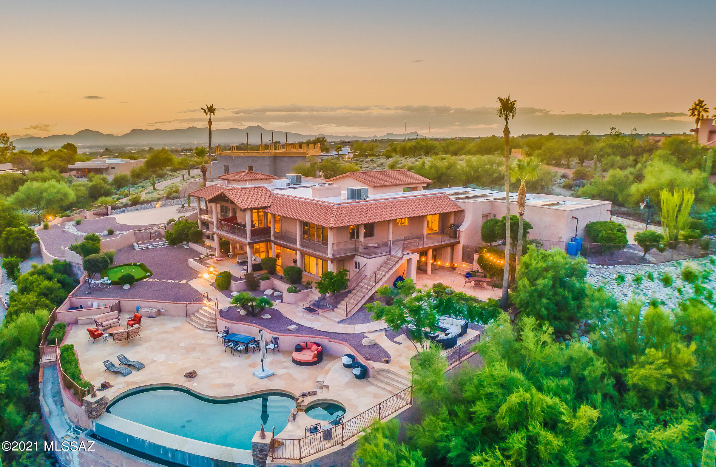 RANGE PRICED: SELLER TO COUNTER OR ACCEPT OFFERS BETWEEN $1,400,000-$1,500,00. Private gated entrance leads to magnificent property on elevated lot at the end of cul-de-sac in highly desirable Catalina Foothills. FIVE BEDROOMS: One Owner's EnSuite on Main Level, Two Jr EnSuite Bedrooms plus Two Additional Bedrooms on Lower Level. FIVE BATHROOMS! TWO OFFICES! Custom Features Throughout! Gourmet Kitchen: SS appliances, Wolf gas stovetop, SubZero refrigerator, breakfast nook, walk-in pantry. Dining Room shares dual sided fireplace with Formal Living. Spacious Owner's EnSuite (main level): Bonus room, private patio, dual vanities, shower, jacuzzi tub, and separate bidet. Breathtaking winding (lighted) staircase leads to lower level to Family Room. Wraparound covered balconies/patios...CONT >>> Private gated entrance leads to palatial property perched on elevated lot at the end of cul-de-sac in highly desirable Catalina Foothills. VIEWS FROM ALMOST EVERY ROOM! Custom Features Throughout! Gourmet kitchen: SS appliances, Wolf gas stovetop, SubZero refrigerator, breakfast nook, walk-in pantry. Dining Room shares dual sided fireplace with Formal Living. Spacious Owner's EnSuite (main level): Bonus room, private patio, dual vanities, shower, jacuzzi tub, and separate bidet. Classic movie worthy circular lighted staircase leads to lower level to Family Room. Two of four lower level bedrooms are en suite. Wraparound covered balconies/patios with breathtaking mountain, sunrise and city night light views. Negative edge pool, spa, putting green, 4-car garage, circular drive, owed solar!!

Upon arrival, you are greeted by the double door entry under a gable roof. The stately grand foyer leads to seamless indoor/outdoor living and entertainment spaces. Exquisite travertine flooring in all rooms except Formal Living Room where real wood flooring glamorizes the experience. Vaulted wood beam ceilings enhance the warmth, comfort and character of this Spanish inspired home. Thoughtful floorpan reflects the Primary Owner's Suite on the main level, with TWO ADDITIONAL generously sized En Suite bedrooms on the lower level. Two Offices/Dens: One on the main level and one on the lower level. Two wet bars: One on the main level, and one on the lower level. Outside you'll find a dragonfly inspired flagstone garden area, rain harvesting system, composting, as well as extended concrete aggregate circle drive allows for additional parking and leads to the four car garage.