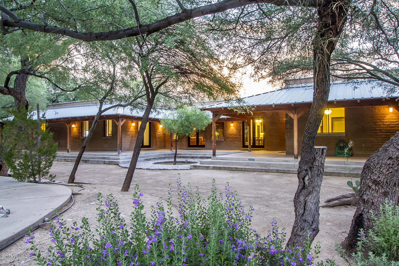The richness of the building materials, 16-inch thick exposed adobe walls, open beam ceiling, polished concrete floors & counter tops and a fireplace built of hand quarried volcanic rock. All set under the canopy of a mesquite bosque in the Tanque Verde Valley. The territorial adobe home custom built in 2001 backs up the the 5th fairway of Forty Niners Country Club. The wrap around post and beam porch with metal roof opens out to the backyard and Pebble Tec pool & spa.
