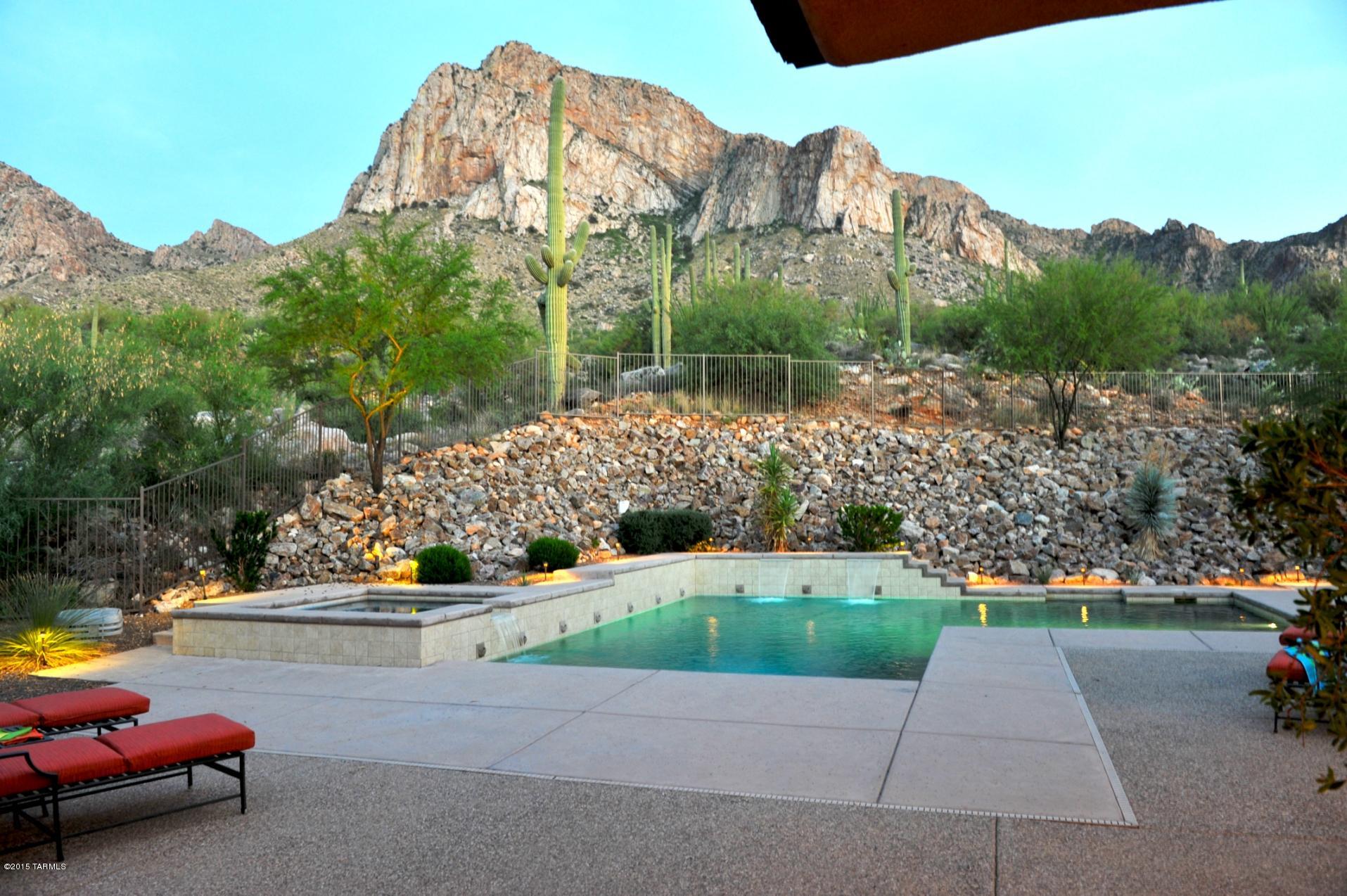 Classic modern design by renowned international architect Charles Stinson. Unique modular & private layout with an owner's 3,402 SF main home (great room, master suite, den/office) connected by a covered breezeway to a 1015 SF guest house with 2 suites and large rec room. Main house with chef's kitchen (Viking appls) and great room with fireplace has soaring windows to showcase valley lights below and the majestic Catalina Mountains/Pusch Ridge behind the tranquil pool & spa area. Your adult family or guests will appreciate the separation and en-suite amenities of the guest house's easy connection to the main house's kitchen and great room. Nestled on under 9 acres of rugged high desert terrain at the top of the prestigious guard-gated community of La Reserve in Oro Valley.