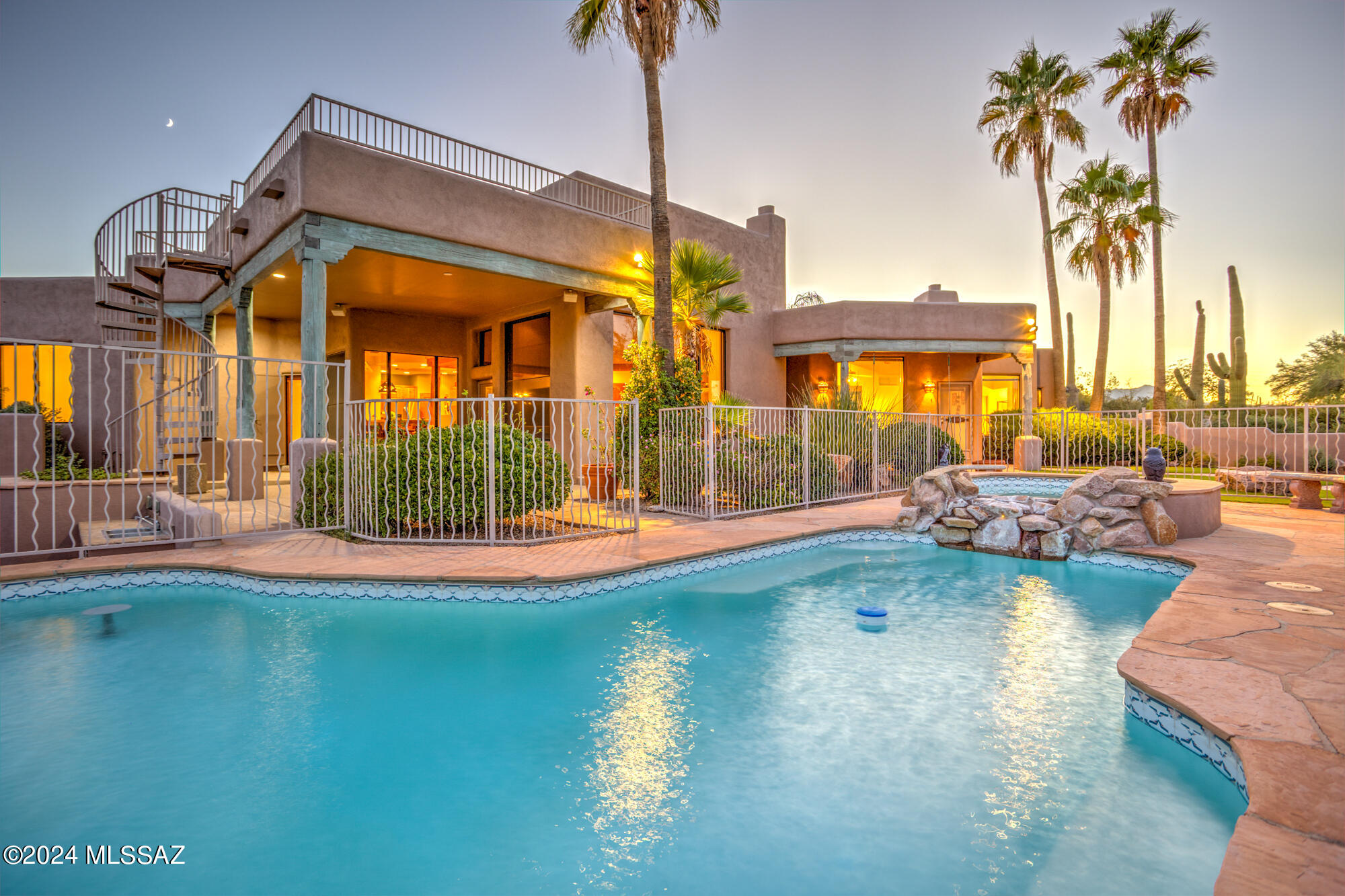 Experience unparalleled tranquility and breathtaking views in this exquisite Santa Fe-style residence, nestled on a 1.76 acre view lot within the prestigious Los Arroyos Del Oeste gated community. Perfect for multi-generational living, this stunning home features an attached guest house that embodies luxury and privacy.  Step into the grand great room, where soaring scraped Viga wood beam ceilings rise over 14 feet high, accentuated by a charming beehive fireplace and expansive windows that frame the captivating vistas. The elegant dining areas blend seamlessly with a chef-inspired kitchen, equipped with modern appliances, a corner pantry, and inviting breakfast bar seating.  Each generously sized bedroom boasts walk-in closets, while the primary suite is a private retreat complete with it's own fireplace, a cozy sitting area or office/den, and a spa-like bathroom featuring a soaking tub, separate shower, and dual vanities.
The guest house offers a private entrance, a full kitchen with an island, and a spacious living area, perfect for hosting visitors or providing an independent living space. Functional elegance continues with a powder room that doubles as a pool bath, while a wrap-around patio enhances the outdoor living experience, showcasing a stunning pool and spa with a waterfall feature and swim-up bar.
Indulge in al fresco dining with an outdoor BBQ and kitchen area, complete with a fireplace, and enjoy the lush new turf that complements the serene landscape. A spiral staircase leads to a rooftop deck, offering panoramic views that elevate this home's charm. This exceptional residence truly epitomizes the best of Tucson living. Discover your dream home today!