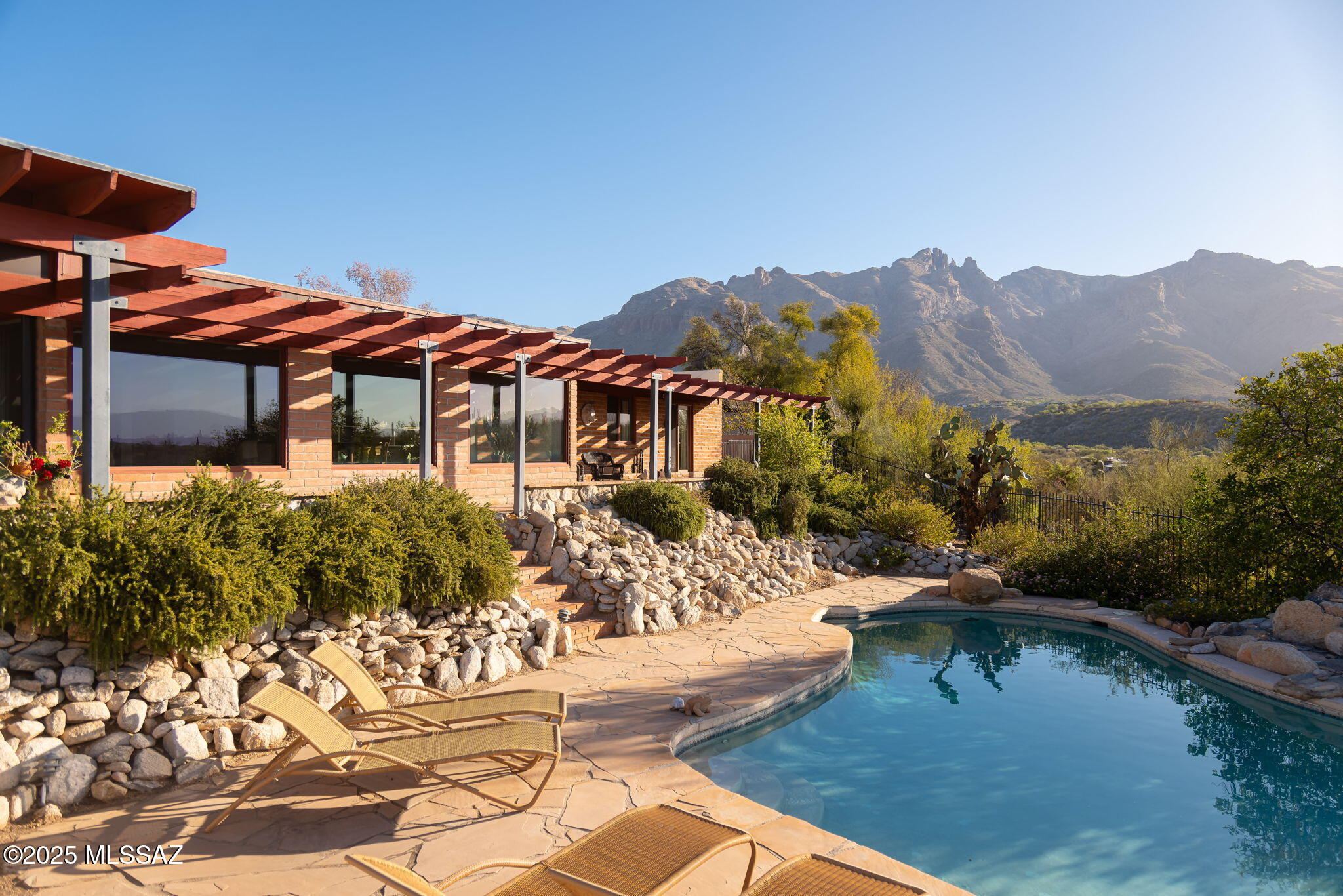 Set high on an elevated lot within the Catalina Foothills, this 1974 burnt adobe home offers sweeping 180 degree views that extend from the rugged peaks of the Catalinas to the glow of the city lights below. Tucked at the end of a quiet cul-de-sac, this property feels both grounded and expansive - its architecture rooted in the desert, its spirit shaped by decades of memory, ritual, and the cadence of Sonoran life. Once inside, generous natural light and thoughtfully framed views define the living spaces - whether it's the mountains illuminated by afternoon sun from the formal living room, or the mesquite filtered light that drifts into the office each day. The open kitchen connects seamlessly to the family room and sunroom, inviting conversation across spaces. A split bedroom plan offers flexibility and privacy, well-suited for multigenerational living, guests, or households with varied rhythms & schedules. With four bedrooms and three baths, the home accommodates both quiet retreat and shared gathering with ease. Saltillo tile floors, thick adobe walls, and warm, lived-in interiors speak to the home's enduring character and tactile honesty.

Outdoors, a covered patio and trellis offer front-row seats to Tucson's elemental beauty: sunrises over morning coffee, the arc of monsoon storms rolling in from the south, vivid rainbows stretching across the horizon, and the hush of twilight as the city lights begin to shimmer below. The pool is both refuge and vantage - whether floating beneath a towering saguaro, sharing a meal beside the water, or watching bobcats and quail pass along the edge of the patio. The golden hour, when the sunset transitions into evening lights is spectacular and must be experienced.

The home is located within the highly regarded Catalina Foothills School District, consistently ranked among the top districts in both Tucson and the state- an appealing consideration for families seeking strong public education in a beautiful, well-connected setting.

With immediate access to nearby trails for hiking, climbing, horseback riding, and mountain biking, and just minutes from La Encantada, St. Philip's Plaza, and the restaurants and galleries of the Foothillsthis home offers a rare balance of privacy, beauty, and proximity. 

Showings are available by appointment, don't miss this incredible opportunity in the coveted Foothills.