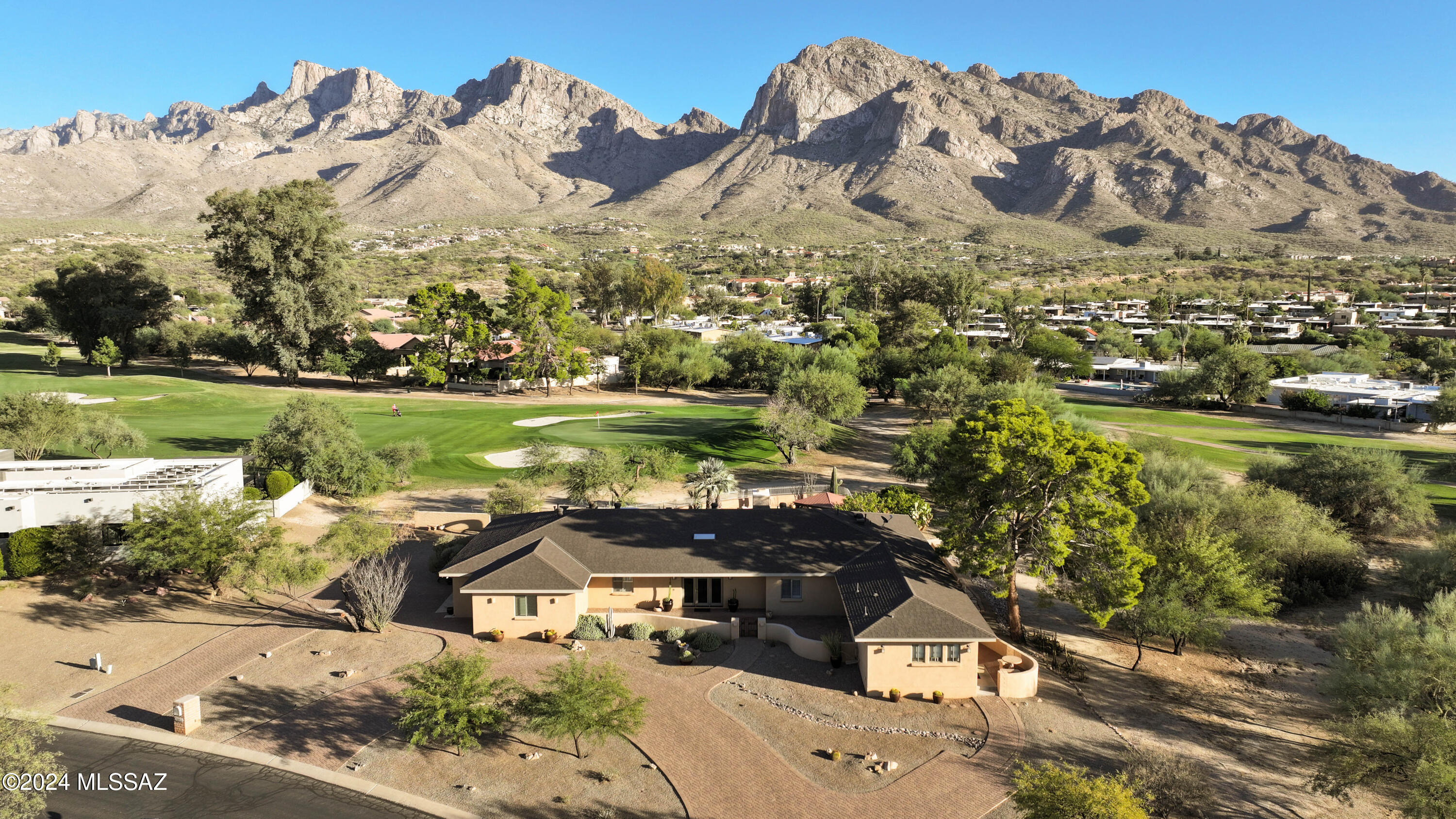 Welcome to a hidden gem nestled in the prestigious Oro Valley Country Club community with unobstructed views of Pusch Ridge. This delightful home situated on a private acre greets you with a circular brick-paver driveway leading to a front courtyard, complete with a fountain. The foyer directs you to the captivating living room with exposed beam ceilings, a gas fireplace, built-in bookshelves, & windows framing spectacular mountain & golf course views. The 3,046 sq. ft. main residence exudes warmth & character, offering 4 spacious bedrooms, 3 baths, and both a two-car garage & golf cart garage. For guests or multi-generational living, the separate guest house provides a private retreat with a comfortable living area, kitchenette, bedroom, and full bath.
Outdoors, immerse yourself in tranquility, overlooking the lush fairways & green with the Catalina Mtn backdrop. Enjoy sunny days relaxing by the pebble tec pool or dine al fresco under the pergola surrounded by fruit trees & mature landscaping that add to the serene ambiance. The kitchen boasts alder cabinetry, granite countertops, Sub-Zero refrigerator, double ovens and a cozy breakfast nook. Entertain with ease in the adjacent Formal dining room.  Additional features include new roof (2023), tile flooring, soft water system, 2 AC systems replaced 2018 & 2022, outside access to basement ideal for a wine cellar or additional storage.  This home is designed for comfortable living, offering style, functionality, and stunning views in every corner. Don't miss this exceptional opportunity in Oro Valley Country Club!