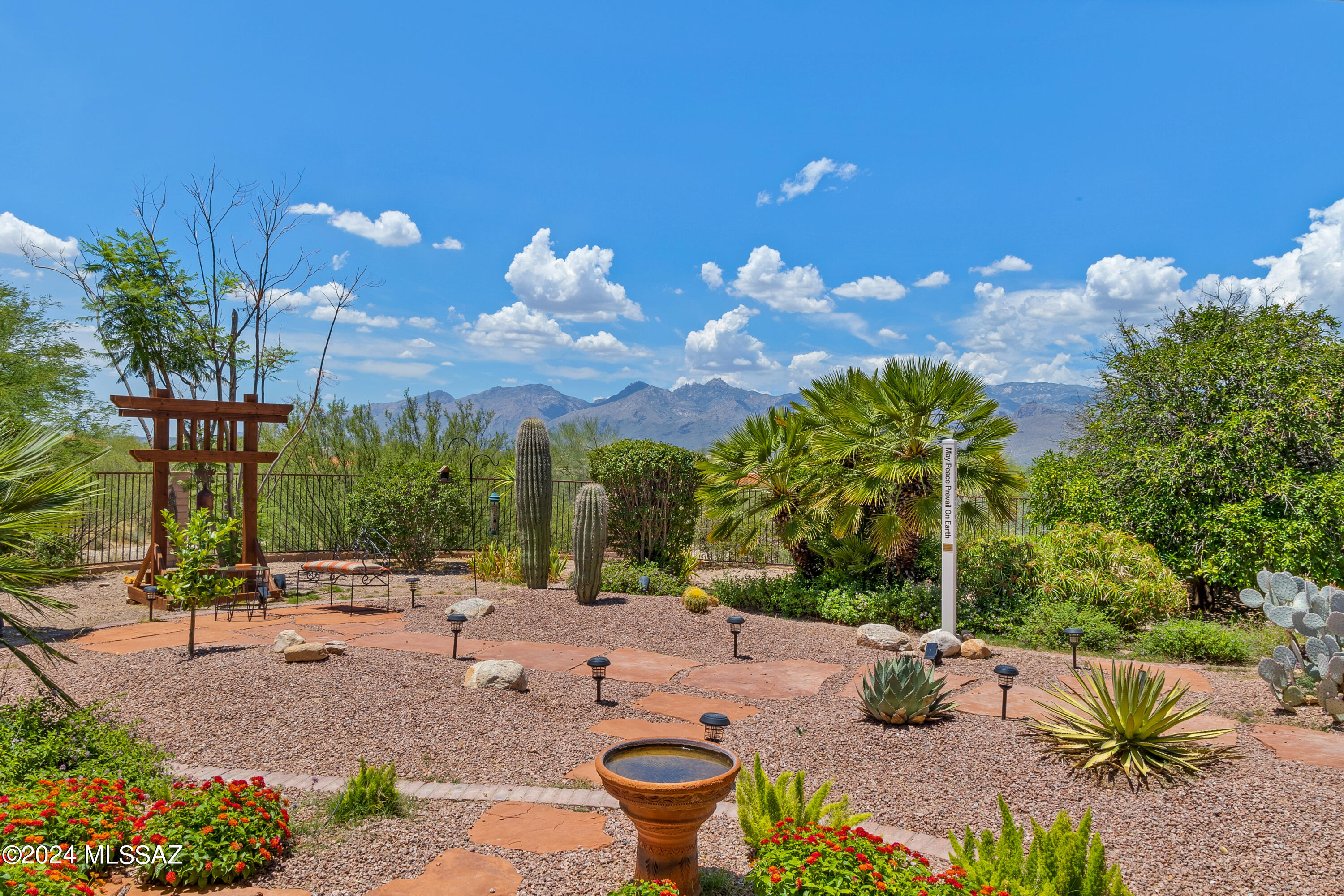 Located on over an acre within the private gated community of Arizona Estates, sits a turn-key home that offers the best in Arizona desert living. The gentle sounds of flowing water and stunning mature landscaping gives you a sense of calm as you approach the grand entryway. After you enter through the large double front doors you are in the formal foyer with soaring ceilings and an abundance of natural light. Straight ahead is the living room with a custom media center and wood burning fireplace. Mountain views can be seen through the large picture window. To the right is the tastefully designed kitchen where you can enjoy natural desert views from the breakfast nook. Continuing through the kitchen you will find a convenient hall bath and large laundry room with ample storage. The 3 car garage, with an epoxied floor, offers space for a workshop. To the left of the foyer is the formal dining room adorned with wood flooring. A large picture window provides you with a front row seat to the beautiful outdoor fountain and mature landscaping. Watch a profusion of birds come and go right from the comfort of your dining room. Through the dining room you will find the primary suite. The large primary bedroom also offers views of the fountain and opportunities to enjoy the wildlife. The primary bathroom has separate vanities, a walk in-shower, jetted-tub, and a sizable walk-in closet. Included in the primary suite is a large room that currently accommodates an office and  large gym equipment. Two guest bedrooms, one with an en-suite bath, are ideal for guest accommodations or office space. The additional full bathroom offers flexibility for when you are entertaining or have overnight guests. Make your way to the backyard where breathtaking mountain views await. This tranquil zen-like backyard design is a rare find in Tucson. The newer irrigation system nourishes the citrus trees and natural desert plantings. Expansive verandas create an ideal environment to enjoy the outdoors. These sweeping verandas wrap around nearly the entirety of the house exterior, cooling the interior home during the summer months. Come see this welcoming home that offers an abundance of peaceful outdoor living spaces nestled within the idyllic community of Arizona Estates.
