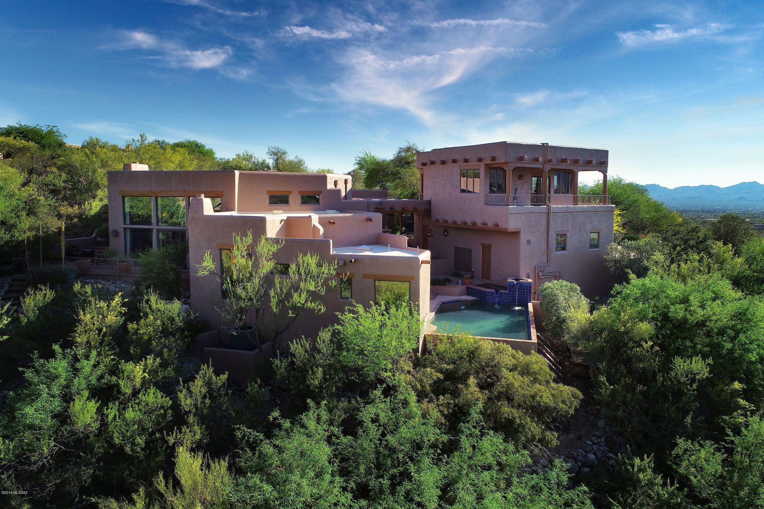 Imagine coming home to a magnificent piece of pure Santa Fe style architectural and cultural living history! This unique home in the guard-gated community of Sin Vacas in the Catalina Foothills offers a rustic, yet regal lifestyle. The premium hill-side lot allows for breathtaking picturesque views of the ancient desert, and its mountain ranges are easily visible from the home's many over-sized windows and outdoor living spaces. The Old-World appeal of this property begins with its entry into a walled Courtyard, featuring a multi-tiered fountain. The wrap-around covered patio invites you down to a spa with a cascading water feature spilling into the negative edge heated pool, all over-looking the endless natural desert landscape generously dotted with mature healthy saguaros, desert acacia and palo verde trees. The spacious Great Room boasts a soaring 16-foot high wood viga beamed ceiling. The corbels, log pole accents, and brick flooring provide a natural relationship to the outdoor terrain. The massive wood-burning fireplace is situated near the window-wall, offering incredible views of the majestic mountains and ancient desert flora and fauna. A second, private, kiva fireplace is located on the opposite end of this huge space, in an intimate sunken banco sitting area making it a perfect spot for gentle conversation. A Library Loft overlooks the massive Great Room, and offers a cozy space for reading, re-energizing, or just a fun place for kids to hang out. A Formal Dining Room is linked to the Great Room, with another kiva fireplace and a round dining table lit by a grand antler chandelier. A Farm-to-Table Kitchen is represented in this authentic Arizona kitchen, offering plenty of space for the chef along with a protected trellised atrium to grow herbs and vegetables. The kitchen features a Sub Zero refrigerator, Wolf 48" dual fuel range with 6 gas burners, Bosch dishwasher, 182 bottle wine cellar, and doors leading to the inner courtyard with its natural floral fragrances. The Master Suite is the epitome of the Southwestern lifestyle, emanating serene, natural energy. It includes a corner beehive fireplace, wooden viga ceiling, window wall with unobstructed views of the ancient Catalina Mountains, and glass doors leading to the pool, spa, and courtyard. A double-sized Guest Bedroom Suite includes a living area opening to the atrium. The large Casita is equipped with its own kitchenette, and features an awe inspiring wraparound deck with 360 degree mountain and city views. Perhaps these pristine scenes will inspire you. Nature at it's finest. By day, night or anytime in between, this one-of-a-kind home is at one with the great outdoors! You'll love the four verandas with their flower and cactus gardens, along with a large three car garage. If wildlife viewing is your thing, or you enjoy stargazing Tucson's "dark skies," this is the perfect setting for relaxing in the spa or enjoying your telescope's personal light show.