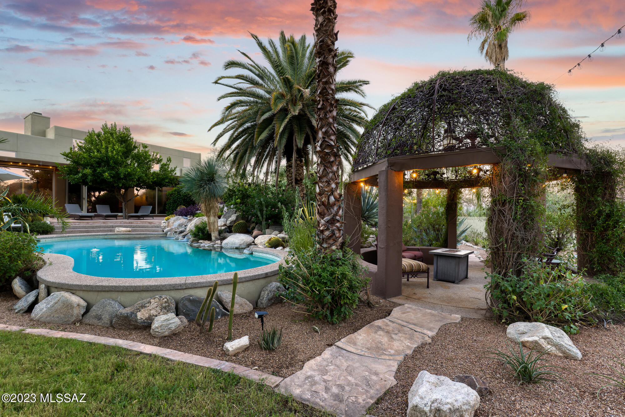 A tranquil desert sanctuary, boasts a stunning 4,178 sqft main house and a separate 1,095 sqft guest house nestled on a 5-acre estate. The thoughtful design featuring a split floor plan, providing privacy and convenience. The heart of the home shows beautiful wood ceilings, and floor to ceiling glass showcasing panoramic views of the Catalina Mountains on one side, and a resort-style backyard with lush landscaping completed by a pool featuring a soothing waterfall and spa. The backyard is fully walled adding to the feeling of security to this well designed outdoor space, creating a true sense of tranquility. The guest house is fully equipped with living room, bedroom, and a full kitchen. The home is located centrally in Oro Vally, close to trails, schools, restaurants and shopping.