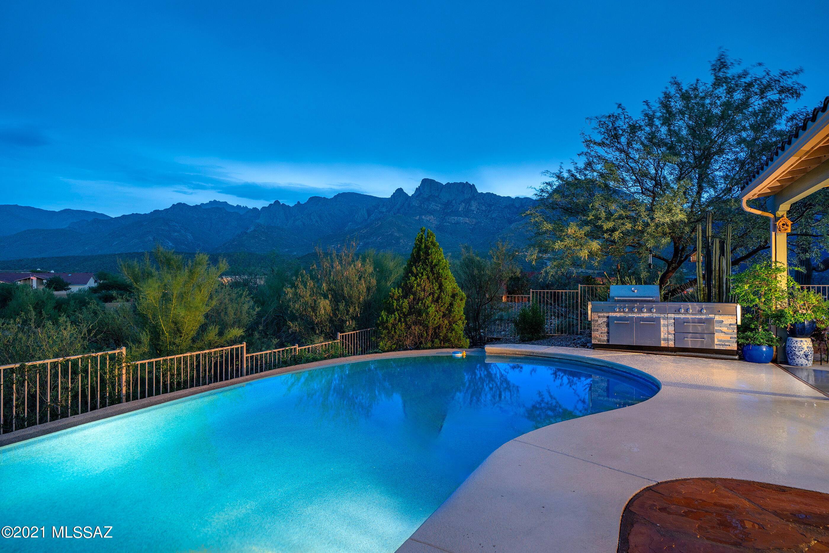 Enjoy some of the most dramatic Catalina Mountain and expansive city views from this privately situated hilltop residence. Sited on 1.03 pristine acres, offering spectacular sunset and city lights, easily accessible throughout the various patios, as well as through picture windows strategically placed to enhance the many surrounding view corridors. A gated breezeway acts as the main point of entry, opening onto the home's primary public spaces, with the owner's suite sequestered on the primary level, offering a combination of luxury fit and finish, complete with a patio walkout, sumptuous bath with dual vanities, large soaking tub with fireplace, walk-in shower and an oversized custom built-out dressing closet. Two secondary suites are featured on the West end of the home, privately situated and perfect for family, or guests alike. The upper level offers a fourth bedroom/flex room allowing homeowners to customize their living space to fit individual interests (i.e. office, gym, guest suite), with a walk-out deck overlooking Pusch Ridge and the Catalina Mountains beyond.

Subtle contrasts are found in the Chef's kitchen, designed by Katrina Mullinax of Homeworks. Custom Alder wood cabinetry by Columbia Cabinets, with built-in wine/beverage storage, open bookshelves and under-cabinet task lighting, set against the tastefully selected travertine tile backsplash, leather finished, chiseled edge granite countertops and pro series stainless appliance package. The breakfast nook flanks the dining, living and family rooms, with vaulting ceilings adding to the dramatic scale and space. 

The exterior provides enhanced natural landscapes with views stretching out over the various mountain ranges in every direction. Enveloping the residence are numerous outdoor living spaces that seamlessly connect, each having been thoughtfully positioned for entertaining, while overlooking the resort-like pool and spa, both elegantly and effortlessly nestled within space.

Walkways meander through the vibrant desert landscapes into a private lower level entertaining area, which includes a 550 sq ft ancillary building, perfect for a workshop, or additional overflow storage. A fully equipped greenhouse supports the mature vegetable gardens,  with the picturesque covered Pergola, fire-pit and activity points, offering the perfect environment for watching the evening sunsets frame the distant skyline.