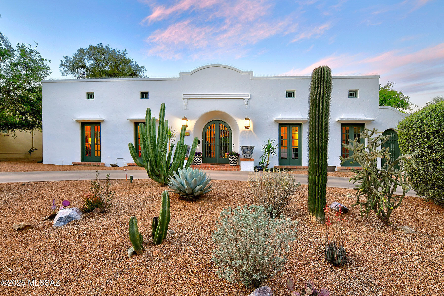 In the highly coveted enclave of Sam Hughes, within the storied University Manor, stands a singular gem — a 1932 Spanish Revival residence of exceptional character and presence, a short walk to the UofA campus and sports complex. With its commanding street appeal and timeless architecture, this home is a rare confluence of history, elegance, and artistry.  Enter through a dramatic zaguan to discover interiors graced with 10' to 12' ceilings, original scored integral-colored concrete, rich brick, warm wood, and timeless flagstone floors. French doors, along with arched windows and doorways, cast dappled light throughout the home, enhancing its romantic charm.
The beautifully renovated kitchen is both functional and full of soul, featuring a 6-burner stove, double ovens, cozy eat-in nook, and clerestory windows that bathe the space in natural light.
An expansive living room boasts a stately fireplace and custom built-in library, while the formal dining room offers refined entertaining with a distinctive hanging buffet. Beyond an arcaded breezeway, a separate family room with soaring beamed ceilings stands at the center of the home. Enhanced by a renowned Tucson Architect, Ned Nelson, it showcases the Artisan's dramatic fireplace and hearth, facing a terrarium.
The primary suite offers a serene retreat with a vintage ensuite bath. A second bedroom enjoys access to a hall bathroom, while a third bedroom suite features its own private, recently renovated bath, ideal for guests or multi-generational living.
Freshly painted inside and out, the home is surrounded by lush, mature landscaping. Adobe walls and ocotillo fencing lend privacy to a backyard sanctuary featuring fruit trees, a tranquil water feature with pond, a covered patio with new concrete overlay, and a glistening pool with a brand-new pump. A separate above-ground hot tub spa completes the outdoor oasis.
This home is on the National Historic Registrar offers lower property taxes for owner occupants. This is not just a home, it is a rare architectural treasure in one of Tucson's most beloved neighborhoods .