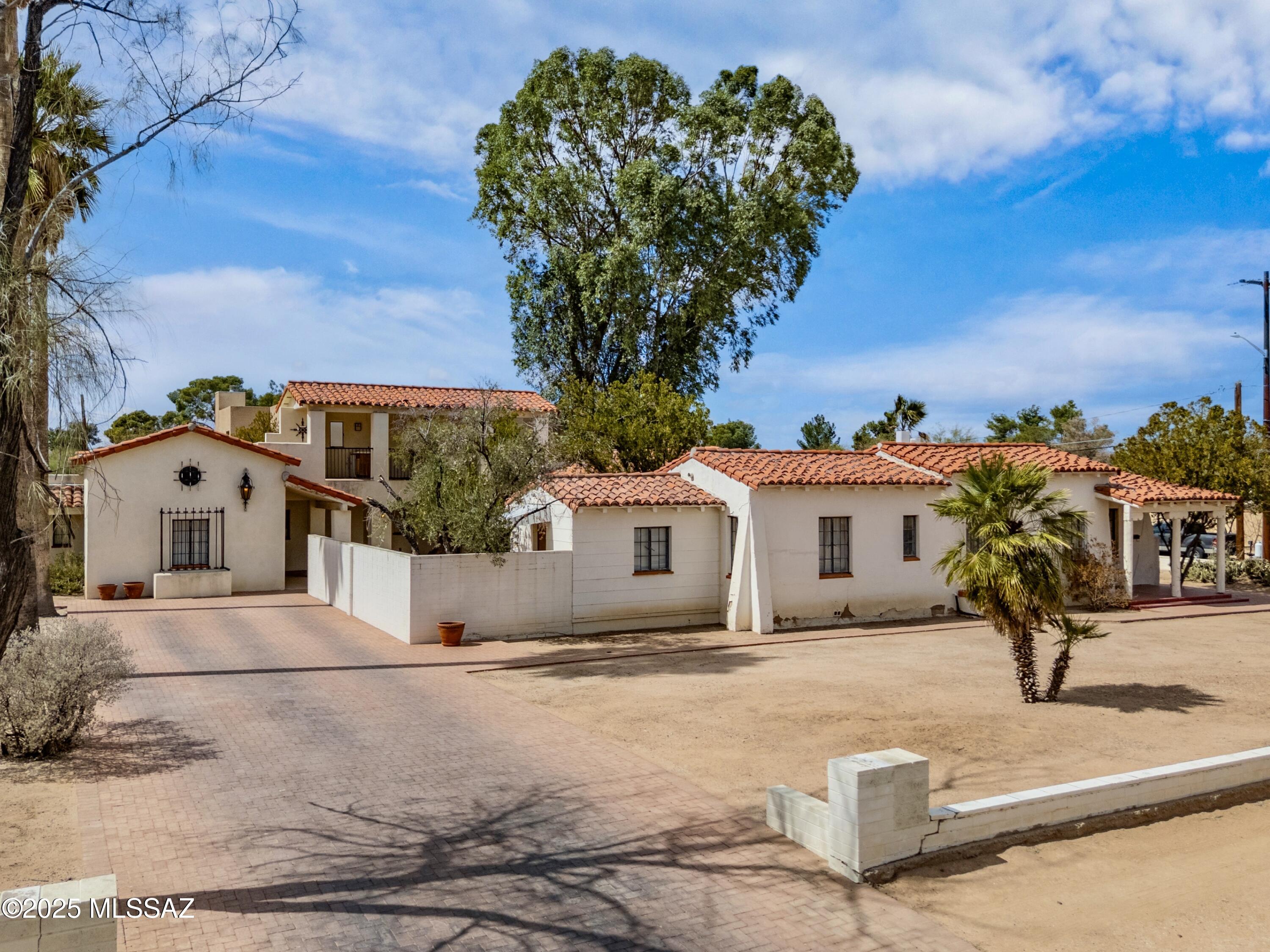 This stunning Spanish Colonial home, designed by Joesler in 1924, is located in the heart of Tucson and features a full guest house addition from 2003. It is a renovator's dream and offers an excellent opportunity to restore the original masterpiece. The property is designed around a large central courtyard with garden beds, covered patios, arched walkways, elaborate ironwork, clay-tiled roofs, and a covered rooftop deck with mountain views. Inside, you'll find gorgeous features including high ceilings with exposed wood beams, hardwood floors, hand-troweled walls, and iron chandeliers and light fixtures. The stately wood-burning fireplace and built-in library cabinets contribute to the charm, while the intriguing layout seamlessly merges intimate spaces with areas perfect for gatherings, both indoors and outdoors. Refer to the floor plan for flexible use of space, as the layout offers multiple office, studio, or storage options, and a conveniently located laundry room for shared access of the residences. Take note of the ample parking in the elongated level paved driveway and along the city curb of the large corner lot. Do not enter the outdoor stairwell leading to the covered rooftop deck. It is blocked off as the tread is unstable. Viewing of the rooftop deck is only available via aerial photography at this time.