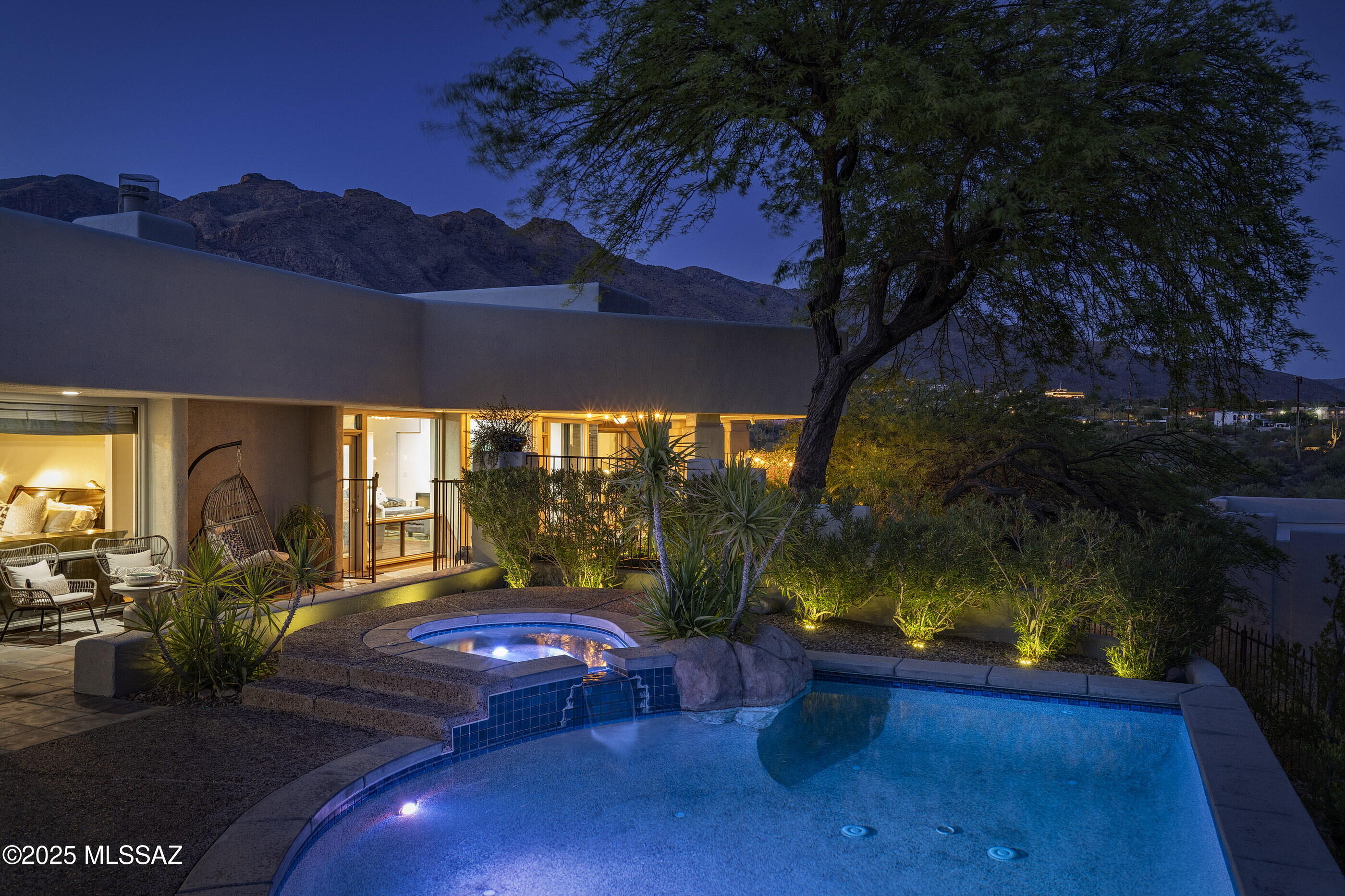 Privately positioned behind the gates of La Paloma Estates, one of Tucson's most established enclaves, this quintessential custom Desert Contemporary by architect David Tyson offers a rare alignment of intentional design, natural context, and enduring quality. 
Framed by the Catalina Mountains, with sweeping city and skyline views, this 3,712-square-foot residence is defined by architectural clarity and spatial efficiency. Clean lines, curated materials, and a restrained palette underscore the home's commitment to design integrity, while its orientation and expansive glazing maximize light, views, and privacy. Four bedrooms and four bathrooms are arranged in a split bedroom plan to support both everyday functionality and separation of space. A 385-square-foot guest suite, complete with a private entrance, offers full autonomy for long-term guests, or separate office quarters, without compromising the flow of the primary residence.

Main living areas are organized around a central kitchen appointed with custom and contrasting millwork, Sub-Zero and Thermador appliances, and streamlined surfaces. Adjoining living and dining spaces connect seamlessly to the outdoors through oversized glass walls and French doors, supporting fluid transitions between the indoor experience and exterior environment. The primary suite is deliberately private, with plank wood flooring and a spa-inspired bath clad in honed travertine. The secondary bedrooms are thoughtfully positioned within the floor plan, ensuring privacy and functionality for family members, or guests alike. Each room is proportioned for comfort and includes well-appointed finishes consistent with the home's overall design ethos. The lower level expands the home's programming with a highly considered flex space, currently being utilized as a separate family room. Windows frame unobstructed Catalina mountain views, a glass-enclosed wine installation serves both aesthetic and functional roles, while integrated ceiling speakers and an east-facing private patio support use cases ranging from theater to studio to wellness. 

Where this home truly shines is in its outdoor living experience, a seamless extension of the architecture and a reflection of the true Tucson lifestyle. Multiple covered patios wrap around the home, each capturing a different angle of light, shade, and view corridor depending on the time of day or season. The southern terrace is a showpiece, with deep covered overhangs offering generous shade while framing the private pool, elevated spa, and outdoor kitchen with built-in barbecue, ample prep space, and bar seating. Perched above it all, a rooftop deck offers a rarefied vantage, complete with a cozy fireplace and sweeping north-facing views of the iconic "Finger Rock" and the full expanse of the Catalina Mountain range. Whether hosting a sunset dinner party, lounging poolside, or enjoying a quiet morning with a coffee and mountain views, the outdoor spaces were designed to elevate every moment. 

Offered within one of Tucson's most desirable and exclusive communities, residents enjoy walking-distance access to a Jack Nicklaus designed 27-hole championship golf course, eight hard and two clay tennis courts, seven pickleball courts, both a Junior Olympic-sized lap pool and a resort-style swimming pool, as well as state-of-the-art fitness facilities, offering a seamless balance of luxury living and active lifestyle.