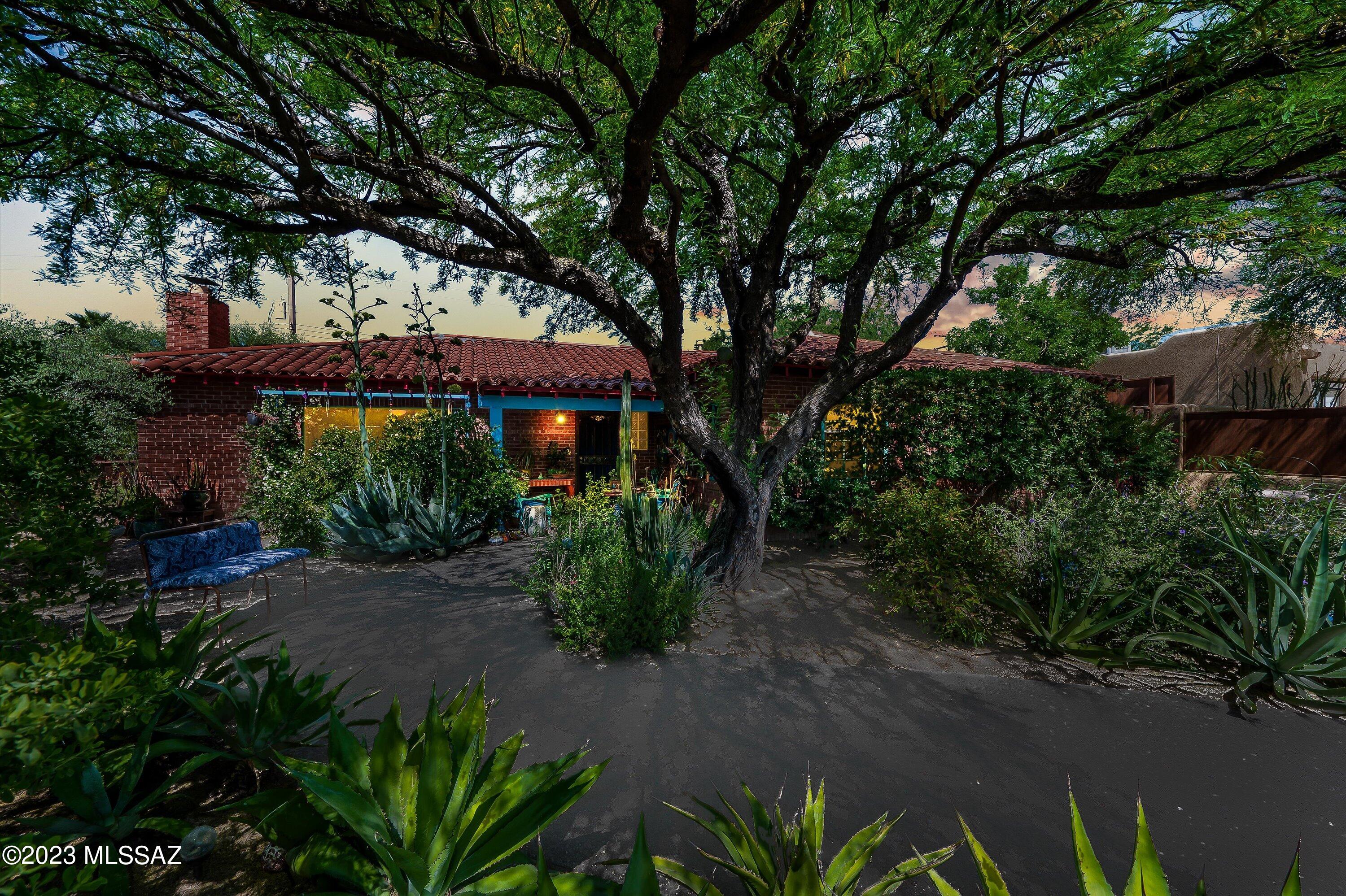 This stunning, 2234 sqft Sonoran Ranch Bungalow is a showpiece in the much-coveted Sam Hughes neighborhood, close to U of A and downtown. Boasting 3 generously sized bedrooms and 2 charming original tiled bathrooms, this home is the epitome of character and elegance. The home features colored concrete tile and scored colored concrete floors, with custom luminary light fixtures and thoughtful custom accents throughout. The large living room and separate family room and dining room areas are anchored by a central built-in bookcase/entertainment center and wood burning fireplace with a custom wrought iron screen. Gorgeous picture windows abound. The foyer leads to a 300 sqft gourmet kitchen with prep sink, tons of cabinetry, a center island with breakfast bar, and an eat-in area surrounded by walls of windows with views of the beautifully landscaped backyard and dining courtyard. The primary suite has a totally private courtyard/patio.  A tandem garage with beautiful metalwork doors accommodates one car, with parking available for more. The lush desert flora on the corner lot, and the many private courtyards and desert flowerbeds on drip irrigation add to the natural ambiance of the home. The custom mural painted by a local artist, beautifully detailed gate/fence work with colored glass accents surrounding the home, and a wonderful color palette give this home all the charm and ambience you've been looking for. With a place on the National Historic Registry, this home has been impeccably cared for and lovingly remodeled, ensuring that it will continue to charm for generations to come.