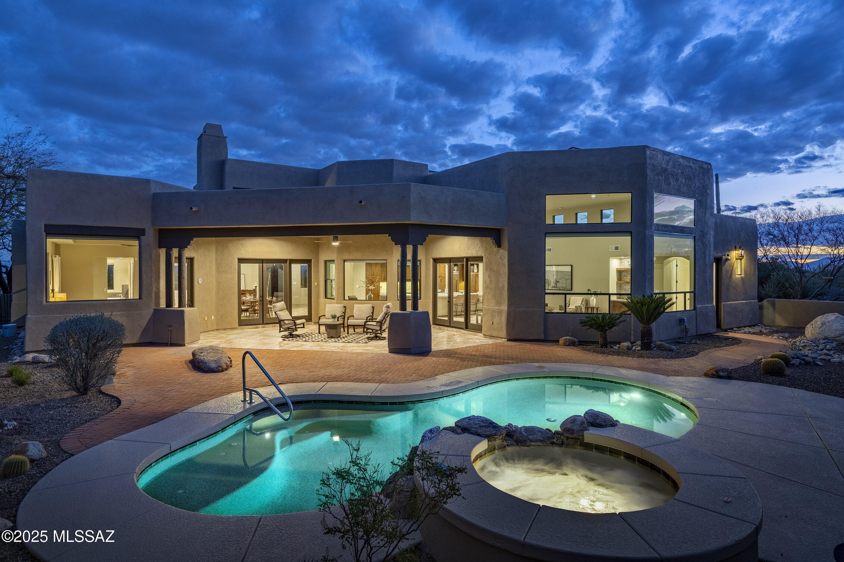 Nestled within the prestigious, cobblestone-lined streets of The Enclave at Pima Canyon in the exclusive guard-gated community of Sin Vacas, this privately situated residence offers an unparalleled connection to the vast and rugged beauty of the Catalina Mountains. Thoughtfully crafted with a refined sense of design, proportion, and materiality, this timeless property embodies classic detailing with modern elegance. The flexible floor plan, featuring four bedrooms and four bathrooms, seamlessly balances form and function, creating an inviting living environment where every detail has been carefully considered. At the core of the residence, the chef's kitchen is a study in material contrast and precision craftsmanship. Custom millwork defines the space, where knotty alder natural wood cabinets meet a striking sage green center island. Expanses of white quartz surfaces establish a serene, monolithic quality, reinforcing a sense of clarity and restraint. Flowing seamlessly into the adjoining dining and formal living areas, the kitchen fosters an atmosphere that encourages both gathering and quiet reflection. From the great room, large glazed openings frame the surrounding landscape, allowing natural light to animate the interiors throughout the day. Multiple points of egress dissolve the threshold between indoors and out, cultivating a continuous spatial dialogue between the architecture and the rugged desert terrain beyond.

The primary suite is privately positioned on the Northeast end of the residence, featuring large dual walk-in dressing closets and a spa-like bathroom. The bathroom includes a walk-in shower with body sprays and a separate soaking tub. Adjacent to the suite, the den/office offers south-facing city views and overlooks the cozy front courtyard. Thoughtfully designed with a split bedroom floor plan, the residence includes two additional ensuite bedrooms, as well as a fourth bedroom which could be utilized as a flex space, with its bathroom also serving as the pool bath.

Adding to the home's energy efficiency and sustainability, a Tesla solar system provides an alternative power source to reduce energy costs. The 13.78 kW DC photovoltaic system consists of PV modules, an inverter, and a mounting system designed for long-term operation. This system is designed to increase energy efficiency harnessing Arizona's natural resources and supporting sustainable living.

Encircling the home, a series of thoughtfully positioned outdoor living spaces create an effortless flow between shelter and landscape. Here, one is fully immersed in the tranquility of the natural surroundings. The sun-drenched terrace, designed for seamless indoor-outdoor living, offers al fresco dining with breathtaking views of the Catalina Mountains. Overlooking a resort-like pool, this space serves as an extension of the home, a place where lifestyle and nature exist in perfect harmony.