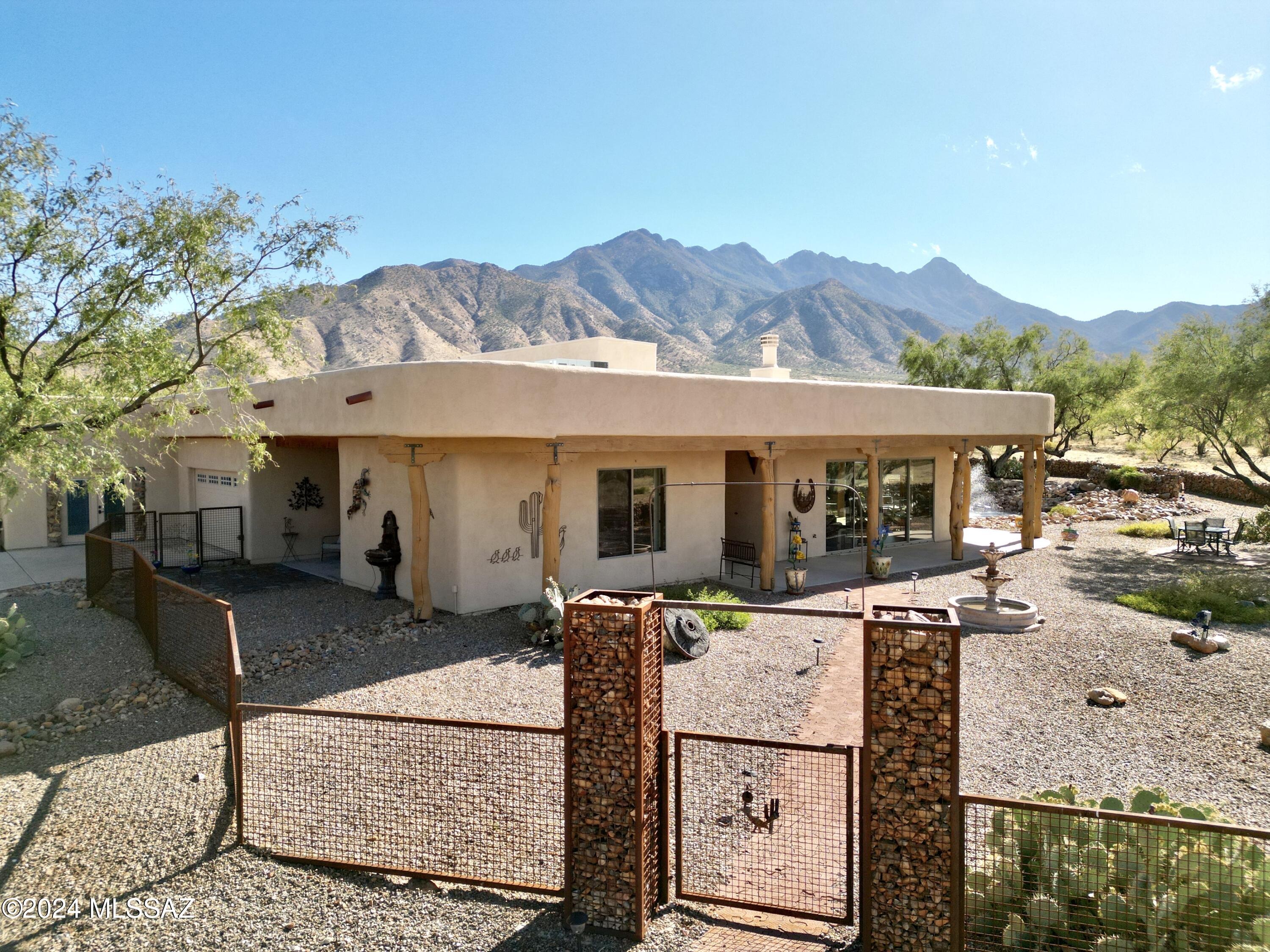 Amazing property at the foot of the Santa Rita's on 4.14 acres of fenced flat ground. Home exudes 3,162 sq. ft. of elegant tranquility. All tile flooring, 10 foot + high ceilings, granite countertops, glass everywhere with unbelievable views of the mountains, valley and pond. Stone walled compound area, registered well, outbuildings and a vegetable garden. Originally designed as a 2 bedroom plus a 3rd bedroom suite with separate entrance, it is presently configured as a 2 bedroom split with a primary bedroom, office and guest suite. High end kitchen cabinets, two islands, great room fireplace with incredible views bring the main living area together. Covered deep patio wraps ¾ around with built in BBQ and granite countertops.  Secluded lifestyle close to I19, shopping and 5 golf courses.