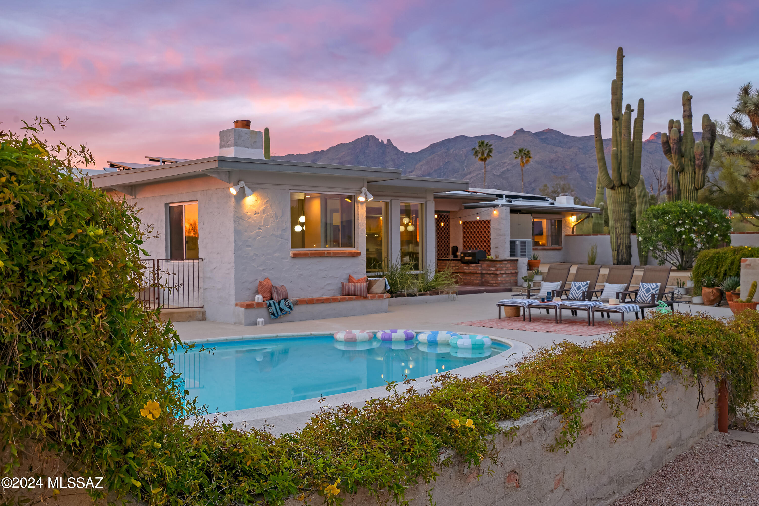 Sited on over an acre, this Midcentury Adobe home was designed by architect Dave Fraker. Abundant windows and a sprawling open plan position this home for premium views of our Tucson mountains and city lights. Floor to ceiling glass and modern design details make this home one of the finest in the Catalina Foothills. Quartz countertops, stainless steel appliances, and custom pantry complete the well appointed kitchen. The primary suite offers two walk-in closets, kiva fireplace (one of four fireplaces in the home), and spacious updated bathroom. Two additional bedrooms and a den/office overlooking the pool and skyline. The grounds include a pool, sport court, saguaro studded veranda, and ample parking. Just a short drive to hospitals, schools, and The Loop (rillito bike path). Owned solar, blown-in insulation, energy efficient tankless water heater, commercial grade exterior doors, roll down shutter and a whole house generator. This home offers superb energy efficiency.