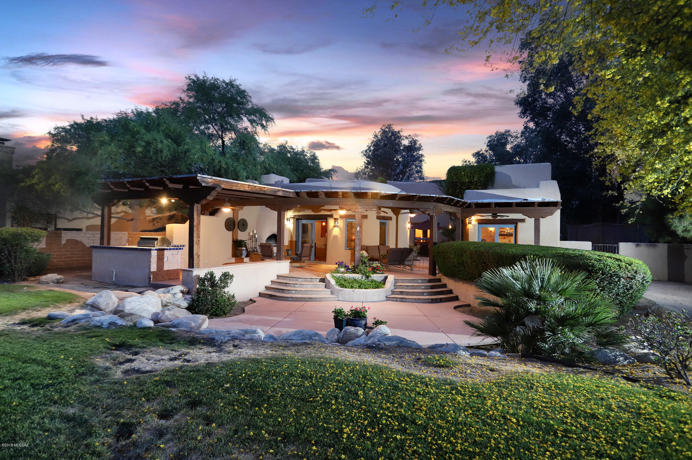 Nestled in a private cul-de-sac in lovely Tucson Country Club Estates is a hidden treasure, a stunningly gorgeous and truly unique mud adobe home reflecting the best of Tucson's gracious Southwestern lifestyle. Enter this magical space via a cobblestone drive and walkway leading into a gated courtyard graced by huge and gracefully gnarled mesquite trees and a charming little seating area. Stop to admire the rich dark wood corbels and vegas, and the rich tongue-and-groove ceiling, of the 3 car carport accented by handsome iron light fixtures and a wooden bench. Notice the antique iron chandelier lighting the front entry area. Step inside to a home of rounded pueblo brick walls and exquisite natural materials that create an organic feeling throughout the home. The salon features a fabulous ceiling of viga beams radiating from a corner of the room out to the curved exterior walls, and completed by a rich tongue-and-groove ceiling known in Southwestern architecture as latillas, a common theme in the home. It's a very cozy space, with another fabulous antique chandelier. Across the entry hallway is an equally dramatic dining room, with openings through the thick pueblo walls into the hallway and graced by an even more spectacular chandelier...don't forget to look up at the high ceiling for more viga beams and latillas radiating from a corner out to the entire room. 
The kitchen is a dream, with stunning thick chiseled edge granite counters rounding into a circular  seating/dining/gathering area softly accented by pendant lights. Appliances, all by Viking, include a commercial grade stove with six burners plus a griddle and two ovens, massive side-by-side refrigerator and freezer. microwave, warming drawer and dishwasher, all with the classic Viking stainless steel exteriors. Once again, very high ceilings feature radiating vigas over latillas, a very artisan-created look. Custom mesquite cabinets are a deep mahogany shade with a rich sheen.  A walk-in pantry, spice shelf and glass-fronted cabinet are also featured. An adjacent cozy family room is also cradled by curving pueblo brick walls and another rich vigas-and-latillas ceiling. A beehive fireplace adds to the warmth of the room. Just off the kitchen and family room is a delightful interior courtyard graced by delightful gardens, a large fountain and draping vines. Beyond is a long covered portal (covered terrace) featuring a kiva fireplace and an outdoor kitchen with large grill and separate cooktop burner set in a traditional tile counter. The rear yard is spectacular, with huge ancient palos verdes and mesquite trees, views of the TCC golf course and, over the lush green desert, sweeping mountain views providing fabulous sunsets, fully enclosed with handsome metal screen fences. 
Back inside, an office/study/project space leads to the media room with another counter of thick chiseled granite topping cabinets and a Viking bar refrigerator, and with a stainless steel sink. Lots of space to sprawl and relax! An exterior door leads to another private courtyard. (Contemporary Southwestern architecture breaks down the barriers between inside and out.)  Beyond the media room are two smaller bedrooms, both with saguaro-ribbed cabinets and built-in desks...homework time! A bath between these bedrooms provides two gorgeous dark metallic glass sinks set in a handsome dark counter that will disguise the results of being used by small children, and a shower lined with rich dark slate tiles and beautiful mesquite cabinets. Back on the other side of the walk-though office is another small bedroom with the same saguaro-ribbed cabinets and built in desk, and featuring a globe crystal chandelier fit for a princess. The nearby bathroom enjoys a copper sink and fittings, with a Jacuzzi bubbler tub and shower in a stone tile surround accented with copper glass insets and mesquite cabinets. The Master bedroom is a gem, a graceful romantic space with high ceilings over the bed area, lovely wall sconces and another gorgeous chandelier, and a cozy sitting area next to another adobe beehive fireplace with a lower ceiling making the space warm and inviting. The bath has a jacuzzi feature and room for two, set in a handsome surround, an attractive mosaic tile design encircling the room, a shower with a chiseled stone surround, and rich metallic sinks set in a chiseled stone counter, with more rich dark mesquite wood cabinetry underneath. A large walk-in closet has another "Princess Chandelier" and lots of beautiful wood shelving. A comfortable casita with its own full bath provides space for visitors. It's a short walk to the Tucson Country Club with many amenities for everyone. 
Throughout the home, enjoy archway room separation, custom doors with a "barn door" look, tan colored polished cement flooring, art niches, unique wall sconces, dark wood fans, skylights and rich natural materials. The home provides a glorious setting for entertaining, elegant yet relaxed living, and raising a family. It's a quiet safe neighborhood where neighbors know each other and kids can ride bikes in the cul-de-sac. It's not pretentious, nothing gaudy, just gracious living in a fabulous one-of-a-kind setting. Inquire about a viewing appointment at your earliest convenience.