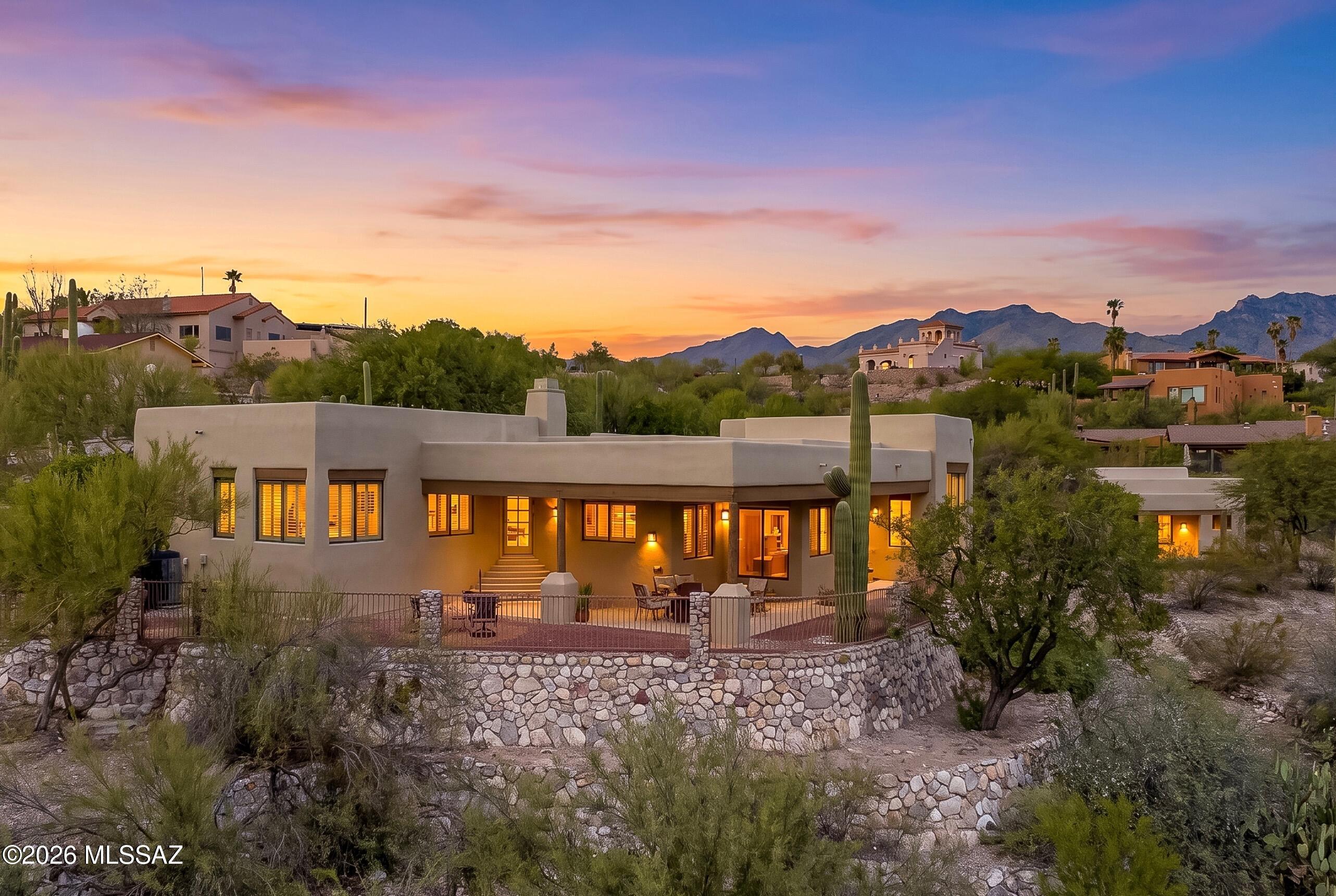 Set on nearly an acre in the Catalina Foothills, this Santa Fe-style home combines generous living spaces, city and mountain views, and a setting that embraces the surrounding Sonoran Desert. Custom wrought iron fencing, native vegetation, and mature saguaros frame the property and create a sense of privacy from the moment you enter the courtyard.
The four-bedroom, three-bath home features a thoughtfully designed floor plan with bright spaces, neutral selections, and Saltillo and concrete floors throughout. Delicately balanced rustic notes and crisp modern finishes offer the best of our Tucson aesthetic. Wood-accented ceilings define the living and family rooms, where a focal kiva fireplace adds warmth and Southwestern character. The open and spacious kitchen centers around an island and takes advantage of views toward the city lights.
Each bedroom offers a walk-in closet, while recent improvements throughout the main home include new plumbing fixtures, faucets, toilets, updated light fixtures, and new door hardware and hinges. These details complement the home's established architectural character while providing a fresh, cohesive feel. 
The outdoor spaces offer several ways to enjoy the desert setting, including an entry courtyard and large covered patio with views toward the surrounding landscape. Enjoy immersion in nature by day, and city lights by night.
The property also includes an attached two-car garage and a separate two-car garage with RV accommodation and a half bath, providing exceptional flexibility for storage, vehicles, hobbies, or the potential conversion to a guest house, subject to applicable approvals.
With its combination of acreage, distinctive Southwestern architecture, flexible ancillary space, and sweeping Tucson views, this property offers a rare opportunity to create a foothills retreat with room to make it your own.