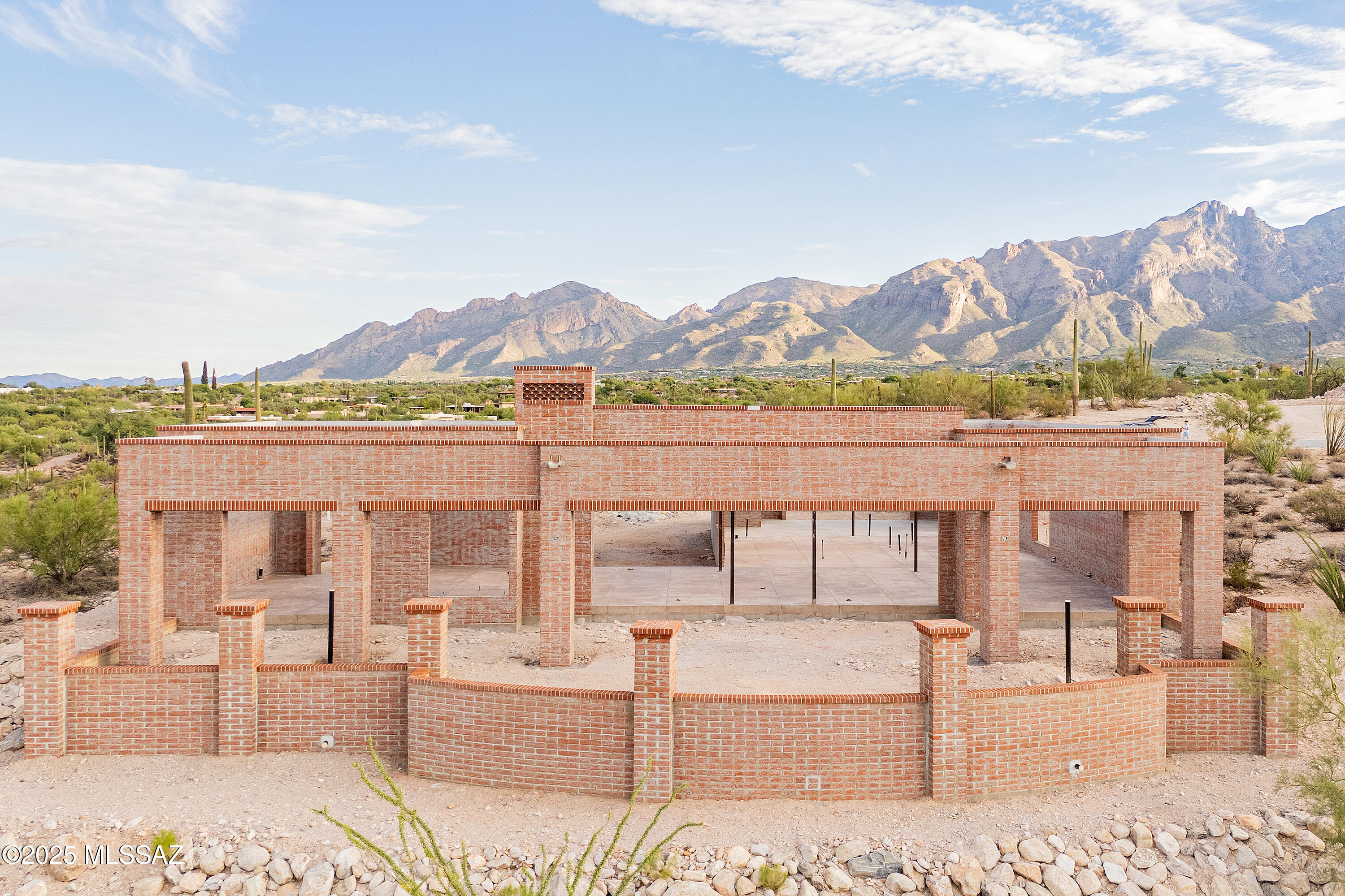 This new construction 2,516 sq. ft. home is more than a style. Contemporary desert vernacular is an architectural language grounded in place, according to local architectural historian R. Brooks Jeffery, respecting the delicate Sonoran Desert environment, and incorporating time-honored design principles with contemporary interpretations that reflect the cultural characteristics unique to Tucson. Situated on .83 acres in the gated Quintana in the Catalina Foothills, this residence offers unmatched city and mountain views and a level of construction quality rarely seen in today's new builds.

Designed by renowned architect Michael Franks and brought to life by La Quinta Building Company, this 2-bedroom, 2 ½-bath is being built to endure, featuring masonry construction with mortar-washed brick details and will be completed with steel casement windows and doors with dual-glazed high-efficiency glass.

Inside, the finished home's spacious great room will showcase walls of glass, a beamed ceiling, and a carved limestone fireplace, seamlessly blending indoor living with the surrounding desert landscape. Scored, integral-color concrete floors flow throughout the home, complemented by custom alder wood and glass cabinetry and 8-foot solid wood interior doors, every detail carefully chosen to elevate the home beyond standard finishes.

The gourmet kitchen will feature a generous center island, natural quartzite countertops, and a premium appliance suite including Sub-Zero, Wolf, and Cove.

This home offers two primary suites, each with spa-like en-suites, which will feature quartzite tub decks, custom limestone tile and glass shower enclosures, and custom-designed walk-in closets with built-in organization.

Additional features will include a fully integrated audio, visual, and security system, state-of-the-art mechanical systems and motorized shades in private areas.

Outdoors, a brick driveway and courtyard entry, hand-forged wrought iron gates and railings, and professionally designed hardscape and landscape will create a striking first impression. The expansive rear porch captures panoramic city and mountain views.  

This single-level home exemplifies architectural integrity and enduring quality, designed as an extension of its natural surroundings creating harmony between architecture and nature. Located just minutes from premier golf courses, country clubs, and world-class dining and shopping. Scheduled for completion in 2026.