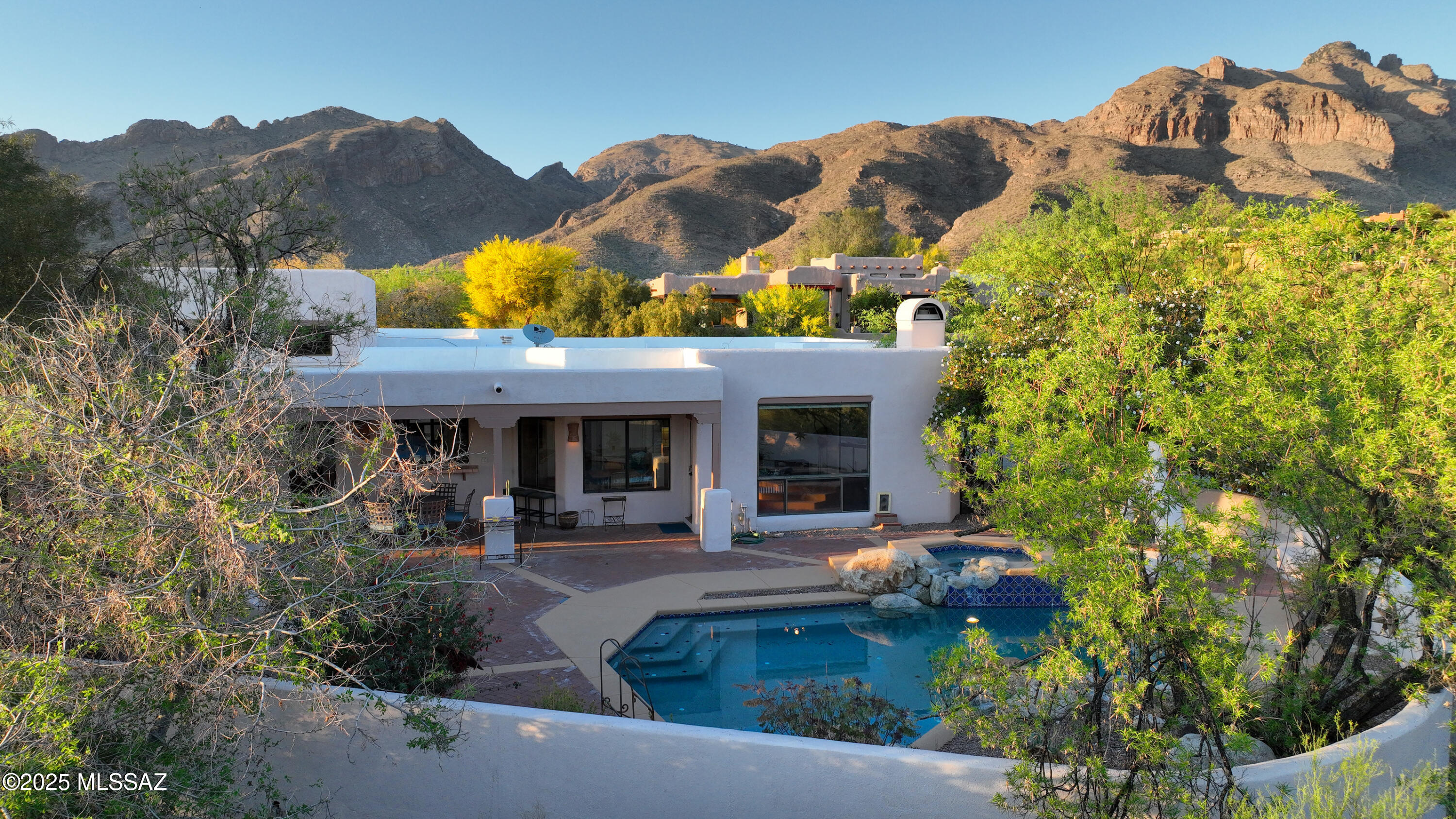 Discover timeless Santa Fe charm in this custom Michael Almli-built home nestled on an elevated .80 acre cul-de-sac lot w/lovely city light and mountain views. Welcoming courtyard entry w/custom wrought iron gate leads you into the home featuring soaring exposed beam ceilings & rich architectural details. Enjoy outdoor living with sparkling pool, spa, Kiva FP and lg cov'd patio w/extended pavers. Inside, the generous kitchen features a terrific island, SS appliances,  abundant cabinet & counter space and opens to a cozy breakfast nook & greatroom w/dramatic FP & wet bar. Spacious primary offers a sitting area, 3-way FP & spa-like ensuite. Formal dining and living room w/south facing French doors. This exceptional foothills  property is just minutes from Tucson's best dining & shopping!