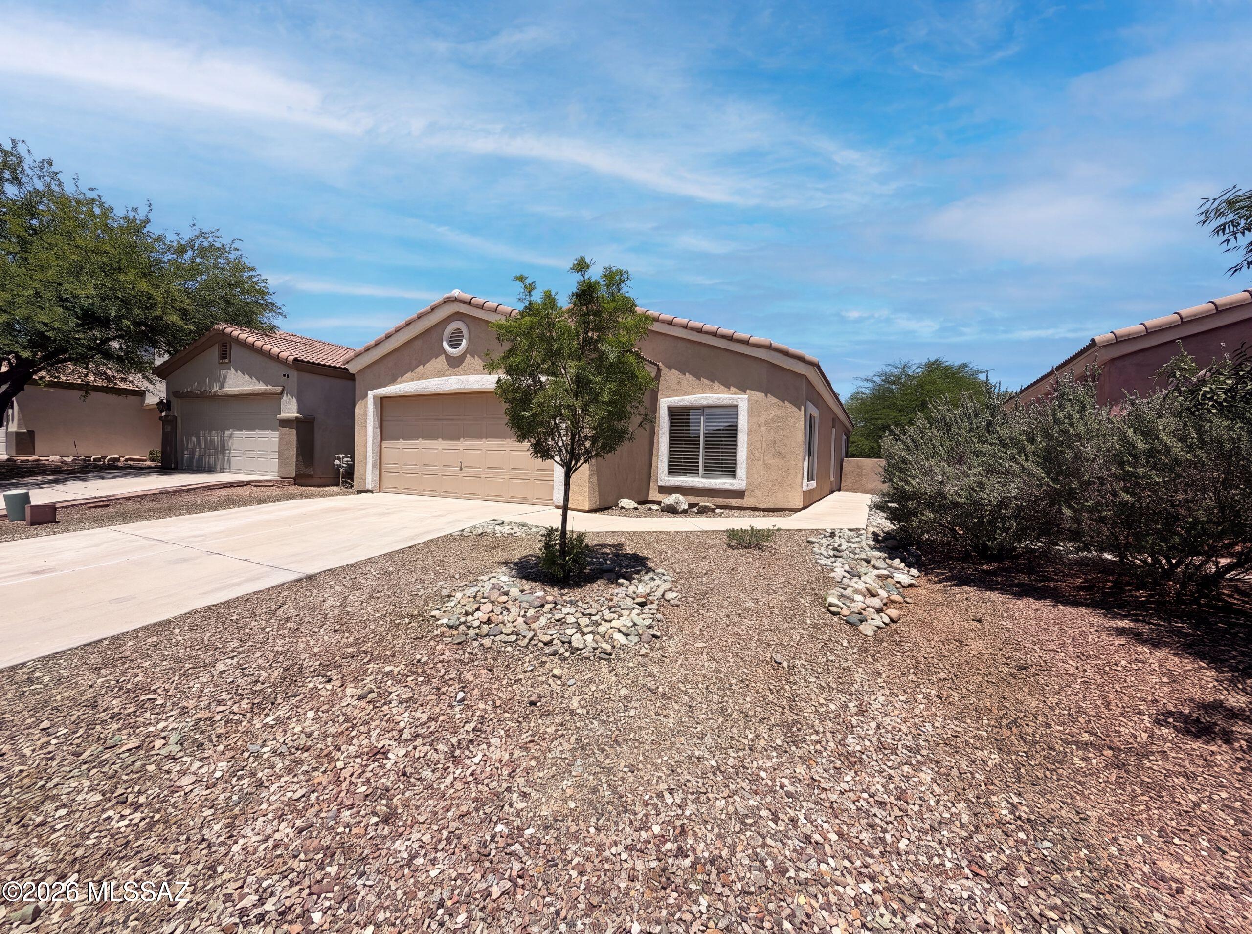 171 E Calle Puente Azul is a single-story Sahuarita home built in 2003. The kitchen includes a peninsula with breakfast bar seating, wood cabinetry, and an adjacent dining area. The main living room is finished with tile flooring and opens to the backyard through sliding glass doors. The primary bedroom is carpeted and connects to a bathroom with a double vanity and a separate tub and shower. Two additional bedrooms and a second full bathroom provide added space, and ceiling fans are installed throughout. Out back, a covered patio overlooks a fully fenced backyard with low-maintenance desert landscaping. A two-car garage completes the layout of this Rancho Sahuarita home.. Included 100-Day Home Warranty with buyer activation