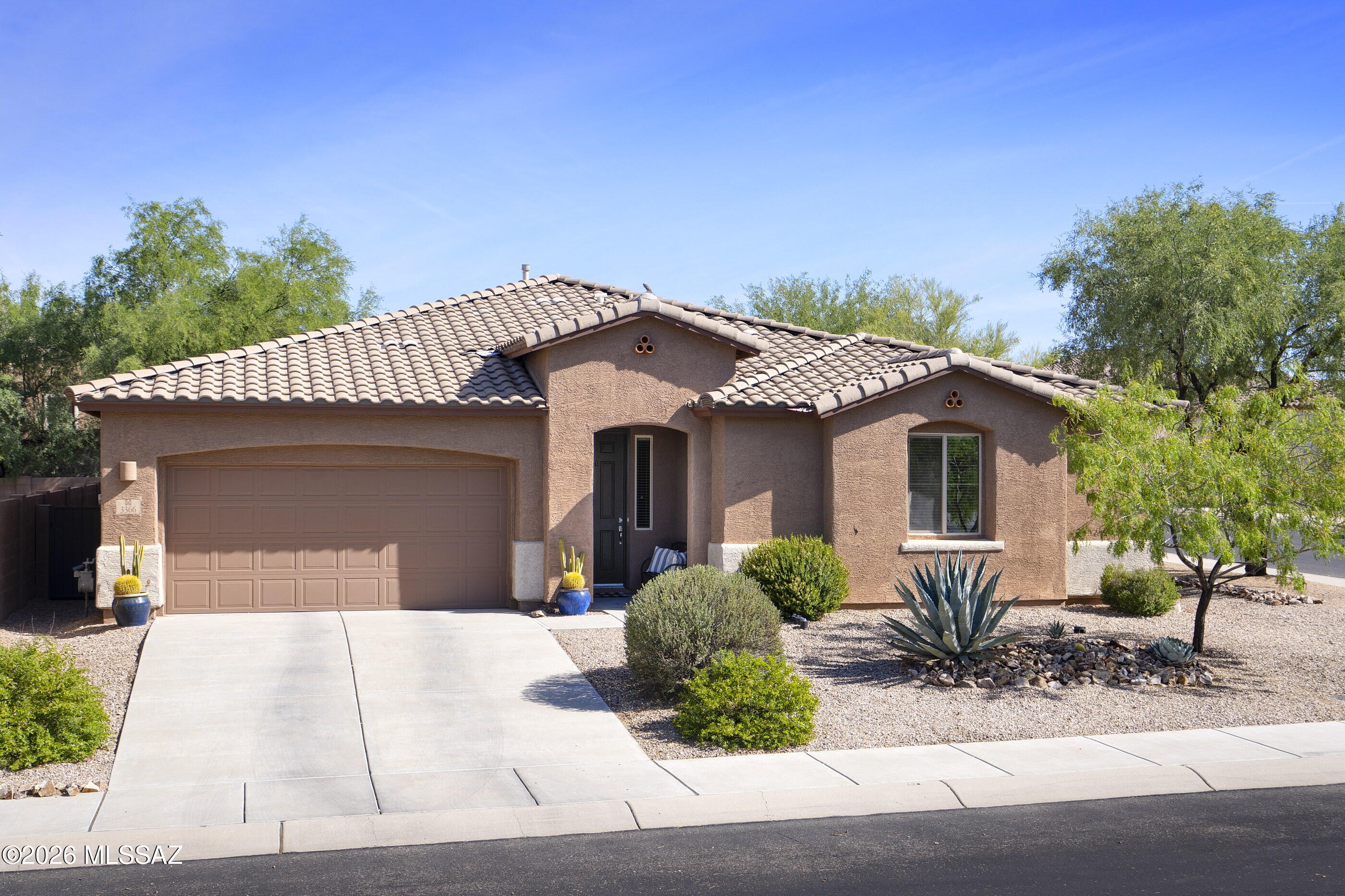 Beautiful 4 bedroom, 3 bath, one story home in gated Tangerine Crossing also boasts a 3 car tandem garage. Guests are greeted in an elegant entry hall with wainscoting and plenty of room for art. This home has an excellent split bedroom floorplan with three ''branches'' that allow the primary suite and one oversize guest bedroom compete privacy, while two additional generously sized bedrooms share a Jack and Jill bath off a separate hall. The light-filled open concept living space boasts a sleek built-in entertainment center from California Closets, a stylish ceiling fan and access to the fully landscaped green backyard. The adjacent dining area has ample space for a 6 to 8-seat table and chic bronze chandelier with a mesh drum shade.  All living spaces and ''wet'' areas feature neutral easy-care tile, and the home has a soft gray paint palette accented by white 8' doors and trim. Home cooks, rejoice! The open kitchen offers an abundance of dramatic dark cabinetry, gray and creamy white granite counters, pantry closet and a full stainless steel appliance package including a 5-burner gas range, double wall ovens, dishwasher, microwave and a French door fridge. Rustic open sphere pendants with Edison bulbs highlight the massive granite-topped kitchen island/breakfast bar--there is room for more than one cook at a time in here!
The private primary suite has a large walk-in closet and its own ensuite bath with an oval soaking tub, walk-in shower, dual sinks and separate toilet room. Down the main hall, a guest bedroom with a walk-in closet is serviced by a full hall guest bath. Another set of guest bedrooms share a Jack and Jill bath with dual sinks and a beautifully tiled walk-in shower. 
There is plenty of room for household supplies in the well-equipped laundry room, complete with cabinets and a sink. A tandem garage currently has the 3rd bay outfitted as a storage and workshop, but you could easily restore it to accommodate another vehicle, if needed. 
The outdoor space is gorgeous and was thoughtfully crafted to give it a lush feel. Mature plantings and faux grass complement the artful design of the covered patio and its sunny extension. There are "peek-a-boo views" of the Catalina and the Tortolita mountains from the backyard. Your new home is located in popular, gated Tangerine Crossing in Marana with easy access to the adjacent Town of Oro Valley to the east and I-10 to the west. This neighborhood has mature trees and two parks for residents to enjoy.