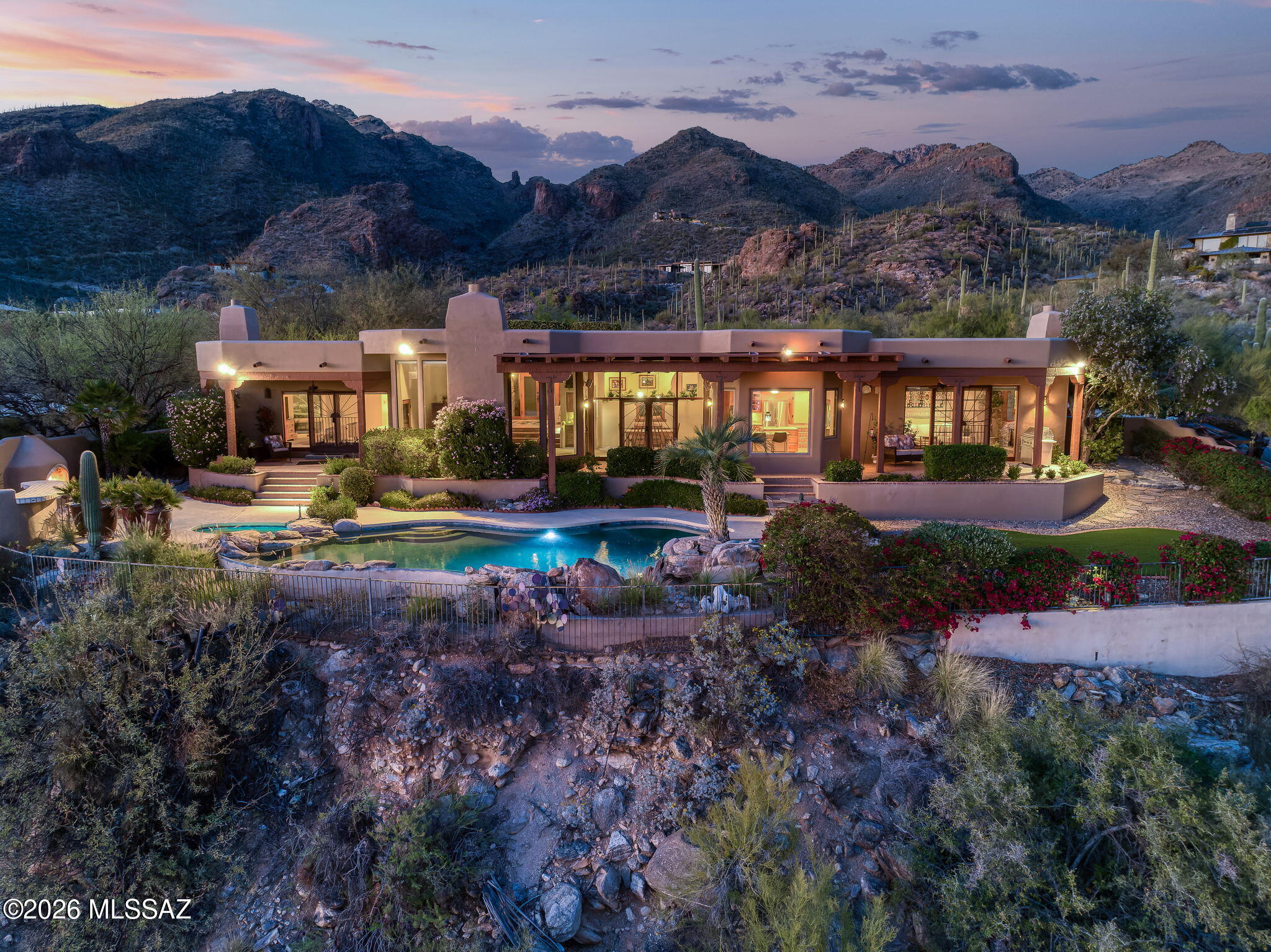 For those who value views and privacy above all, this custom home in gated Canyon View Estates delivers. Set on an elevated 1.38-acre homesite--one of only three on the street with a north/south exposure--at approximately 2,700 feet above sea level, this Catalina Foothills residence captures truly spectacular views of the city, mountains, Tucson's iconic sunsets, & the Ventana Canyon golf course.
Canyon View Estates is located in the highly sought-after Catalina Foothills School District #16 and is within walking distance of Canyon View Elementary & Esperero Canyon Middle School. This location provides a remarkable combination of natural beauty, views, privacy, and proximity to Tucson's finest amenities. A circular driveway laid with one-of-a-kind native stone leads to a charming gated... courtyard with lush landscaping and a tranquil water feature. Upon entry, a dramatic wall of windows frames a stunning elevated view overlooking the city, creating an unforgettable first impression.
The home features a desirable split-bedroom floor plan with four bedrooms, three bathrooms, and a den/office, offering comfortable separation between the owner's suite and the guest bedrooms. Throughout the home, warm architectural details--including stacked stone accents, wood-beamed ceilings, skylights, custom wood doors, wood-encased windows, and four fireplaces--create an atmosphere that exudes warmth, charm, and quality. The remodeled kitchen is positioned to capture views and features granite counters, a butcher-block center island beneath a large skylight, two sinks, stainless steel appliances, custom cabinetry to the ceiling with lit glass-front display cabinets, a custom copper hood vent, and a built-in breakfast bar. A bright breakfast nook just off the kitchen provides the perfect setting for casual dining with a view. The kitchen opens seamlessly to the family room, where a stacked-stone fireplace creates a warm focal point and french doors provide direct access to the backyard.Living spaces are designed for both everyday living and entertaining. The living room includes a wet bar with custom cabinetry and a generous dining area ideal for large gatherings.
The spacious owner's suite enjoys mountain views, a gas fireplace, a skylight above the bed for star-filled nights, and a private covered patio with spectacular city, mountain, and sunset views. The owner's bathroom features wood-look tile flooring, dual vanities, a jetted soaking tub with a corner window framing remarkable views, a separate shower, and a large walk-in closet with custom built-ins.
A separate bedroom wing includes three additional bedrooms and two bathrooms, including a remodeled Jack-and-Jill bath with dual sinks and a custom tile shower.
The resort-style backyard features a PebbleTec pool and spa, water feature, expansive covered patio, artificial turf, and lush landscaping throughout. From its elevated vantage point, the outdoor living spaces enjoy sensational city, mountain, and sunset views. Designed for both everyday enjoyment and entertaining, the backyard includes a built-in bar area near the wood-burning outdoor fireplace--perfect for gatherings large and small.
The additional land provides a natural privacy buffer and potential future expansion. The adjacent seasonal creek also enhances the sense of space and privacy.
Additional highlights include custom wrought iron screen doors throughout, an oversized three-car garage with epoxy floors, built-in cabinetry and workshop area, a laundry room with sink and storage, and HVAC replaced in 2024 with smart thermostats.
Ideally located just minutes from Sabino Canyon Recreation Area, Canyon Ranch Wellness Resort, Ventana Canyon Country Club, and everyday conveniences, including Whole Foods, Bashas', restaurants, cafés, and shops. Canyon View Elementary and Esperero Canyon Middle School are within walking distance.