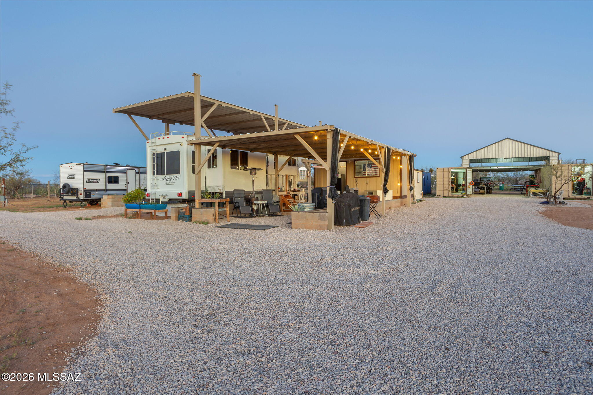 Welcome to a one-of-a-kind 1.25-acre ''Destination RV'' retreat that redefines what rural living with full amenities truly looks like. This remarkable property has been thoughtfully developed from the ground up, featuring a fully upgraded 2014 36' Arctic Fox 5th wheel with dual-zone mini split heating and cooling, a wood-burning stove, electronic keypad entry, 4-stage reverse osmosis water system with remineralization, residential-sized refrigerator, projector with drop-down screen, custom built-ins, pull-out desk, and a Cannon Landmark safe - all designed for comfortable, full-time living. The grounds are equally impressive, boasting over 100 tons of manicured gravel, 60 preserved mesquites, and an array of industrial-grade steel shade structures on concrete foundations including a 36x15 RV/tiny home cover, a 36x18 ramada with draw shades, a 22x20 automotive shop, and an 18x20 rear storage structure. Two 320 sq. ft. climate-controlled workshop/storage units, an 18x12 wellness studio with A/C, a dedicated laundry room with on-demand water heater, and a plumbed supply shack add incredible functionality to every corner of the property. Livestock lovers will appreciate the dual pens with no-climb and electric fencing, a chicken coop with covered yard, a steel cattle panel yard with farrowing area, and field fencing with barbed wire on three sides. Two full RV hookups - a 50-amp primary and a 30-amp guest - are complemented by Thim utility water service, a 3-bedroom septic system, and five water spigots spanning over 200 feet of trenched plumbing, making this property as practical as it is extraordinary. Whether you're seeking a private homestead, an income-producing RV destination, or a versatile multi-use compound, this property delivers an unmatched lifestyle opportunity in the heart of the Sonoran Desert.