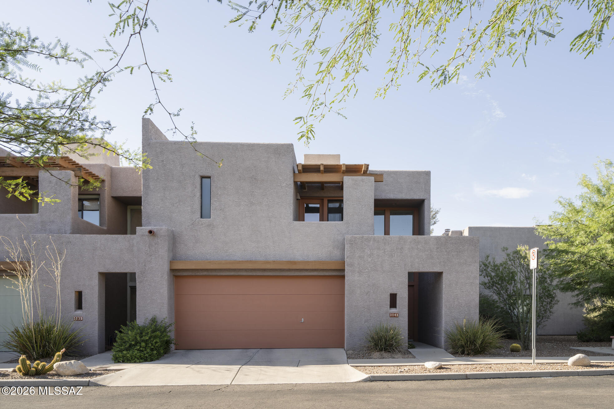 Designed by Tucson architect David Tyson, this Southwest modern end-unit townhome is defined by strong horizontal lines, layered massing, soaring ceilings and carefully framed views. Tyson's characteristic recessed-square motif gives rhythm and depth to the broad roofline, creating a distinctive architectural presence within this intimate enclave.
Inside, the two-story plan is open and light-filled, with tall ceilings that create a generous sense of space. Living and dining spaces flow easily together, while large openings draw the eye outward and connect the interior to the desert light. Upstairs, two bedrooms and two baths provide a comfortable, efficient layout, complemented by an attached two-car garage. Set within this small community of homes, the property offers both retreat and connection. The Loop and Tucson Racquet & Fitness Club are just moments away, with convenient access to restaurants and shopping. A thoughtful expression of regional modernism, designed for an active and uncomplicated Tucson life.