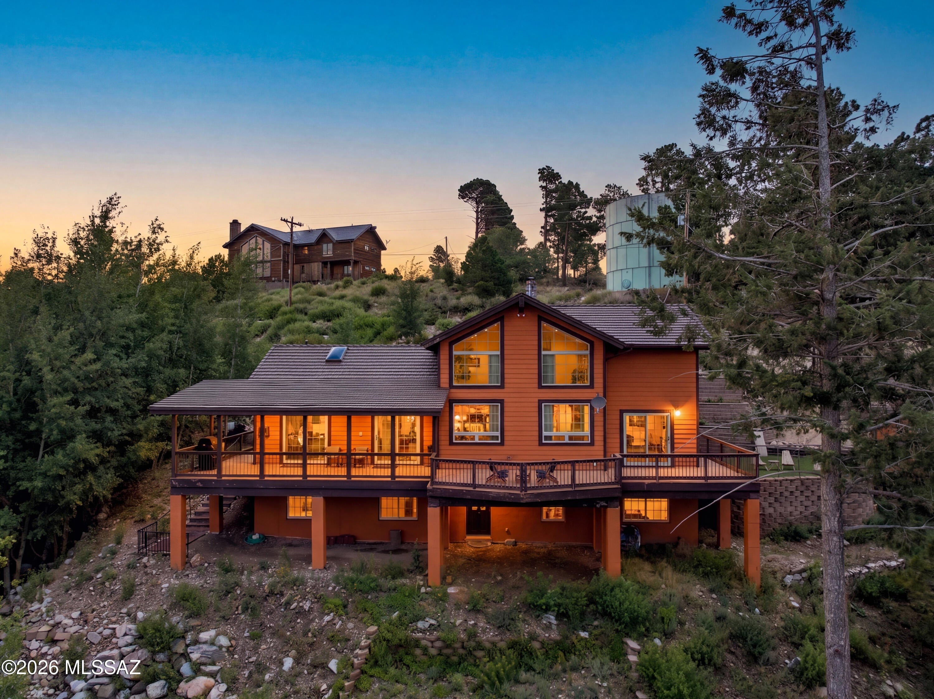 At 8,200 feet -- an hour from Tucson -- the air changes. When the city is sitting in the triple digits, it's in the 70s here: windows open, no AC, cool nights and quiet mornings.

Tucked at the end of a private dead-end lane, this fully furnished custom mountain home is one of Mt. Lemmon's signature properties. The lane closes in a circular turnaround, and a colored concrete driveway gives family and guests plenty of room to pull in.

Inside, 3,581 sq. ft. rises under soaring vaulted ceilings, with walls of windows framing panoramic views and wraparound decks that carry the living space outdoors. The chef's kitchen with granite counters is built for a crowd. A pellet stove and gas fireplace warm the winters, and the primary suite's jetted spa tub is exactly where you want to land... after a day on the ski hill. Modern furnishings throughout convey -- walk in and it's done.

Five bedrooms and three baths, plus a loft with a queen Murphy bed and its own closet for a sixth sleeping space. The lower level adds a kitchenette and lives as a separate wing -- ideal for teenagers and their friends, or for visiting family who want their own space. That flexibility, paired with the bedroom count and oversized kitchen, also makes this an unusually strong candidate for vacation rental or Airbnb income between stays.

Outside, lush natural landscape and terraced gardens thrive on the mountain's own terms, supported by large water storage fed by the gutter system. Built to live up here year-round: steel shingle roof and whole-house generator.

At $321 per square foot -- fully furnished and turnkey -- it's priced well under anything comparable currently offered on the mountain and without an HOA. A primary residence, a summer escape, or a legacy property for generations to come.