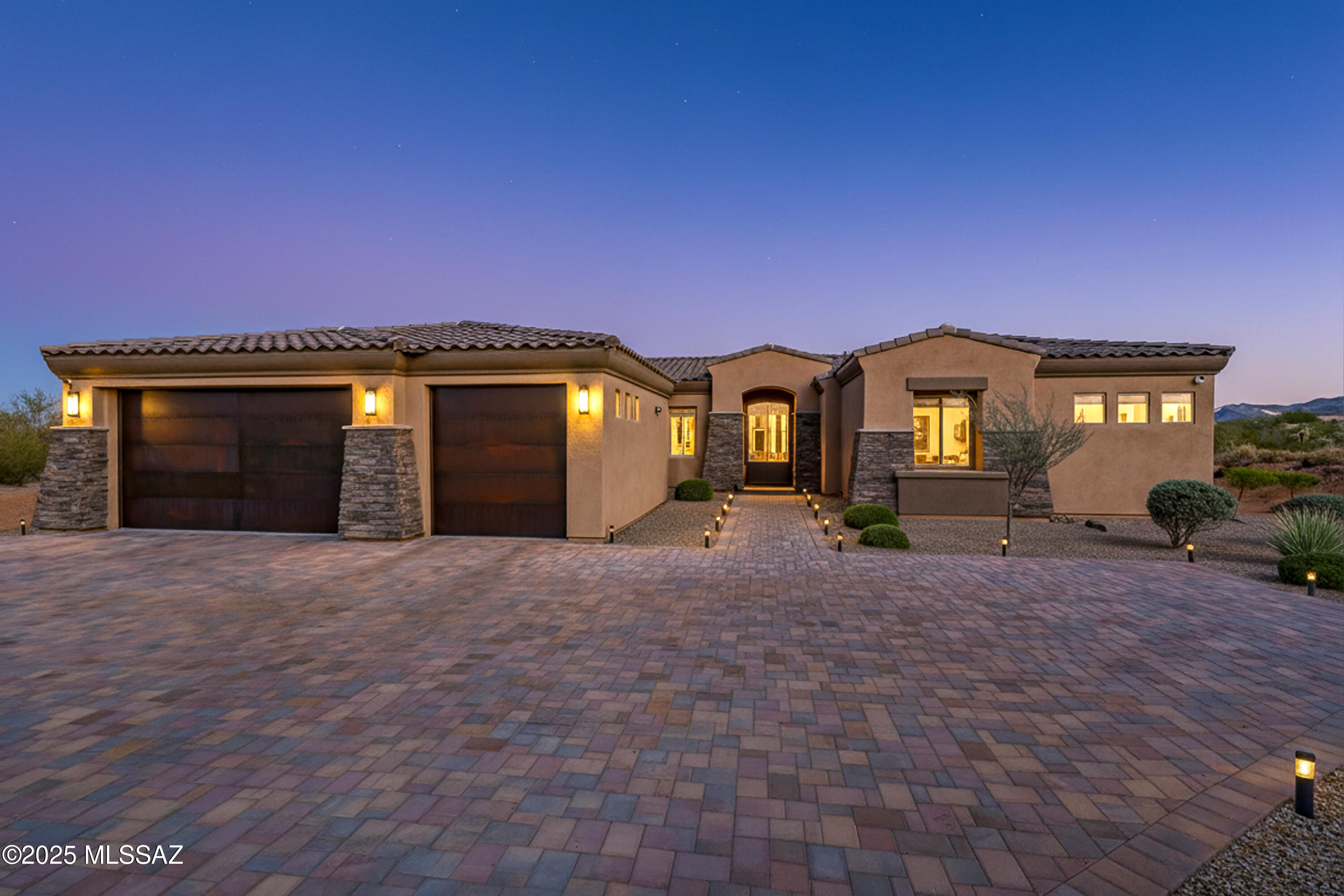 From the moment you pull up, this home makes a statement. Set on over an acre in Stone House, the curb appeal is refined, custom-level luxury with a wide paver driveway, stacked stone accents, and oversized modern metal garage doors. The elevation creates a true estate feel, with privacy, separation, and space that is rarely found in newer Southern Arizona builds.

Inside the modern luxury continues. With 13' ceilings, wide hallways, and unobstructed flow from entry to great room, this home lives BIG. Every space feels open, light-filled, and visually connected, just like a high-end custom build should. 

Wood-plank porcelain tile runs throughout, creating a continuous flow from room to room. In the main living areas the modern brushed brass light fixtures, sleek black fans - and clean architectural lines give the great room and dining room a designer, high-end look.

The kitchen is a true showpiece of quartz counters, white cabinetry, a full glass-face upper cabinet wall, wine fridge, walk-in pantry, and professional KitchenAid appliances all tied together with a contemporary mosaic backsplash. Even the everyday details feel elevated, small appliance "stations," modern lighting, and extra cabinetry give you the functionality unexpected.

The powder bathroom even has a full-textured accent wall, giving it a boutique hotel feel and memorable style.

The primary suite is spacious, peaceful, and perfectly placed with private patio access, dual walk-in closets, and a luxury tiled shower. Both additional bedrooms are ensuite perfect for guests, seasonal residents, or multi-gen living.

The laundry room is oversized and upgraded with storage and upper cabinetry. And the 3-car garage is extended, with ceiling storage racks already installed.

From the backyard and covered patio you'll enjoy true Southern Arizona evenings glowing sunsets washing over the desert landscape and mountain views that feel like a moving piece of artwork right outside your door.

Outside, this is the Arizona lifestyle people move here for quiet desert surroundings, mountain views, that make evening outings feel like an all inclusive resort community.

Move-In Ready, Impeccably Designed, Built and Maintained to Impress all who Live and Visit this Stone House Residence. A truly One of a Kind.