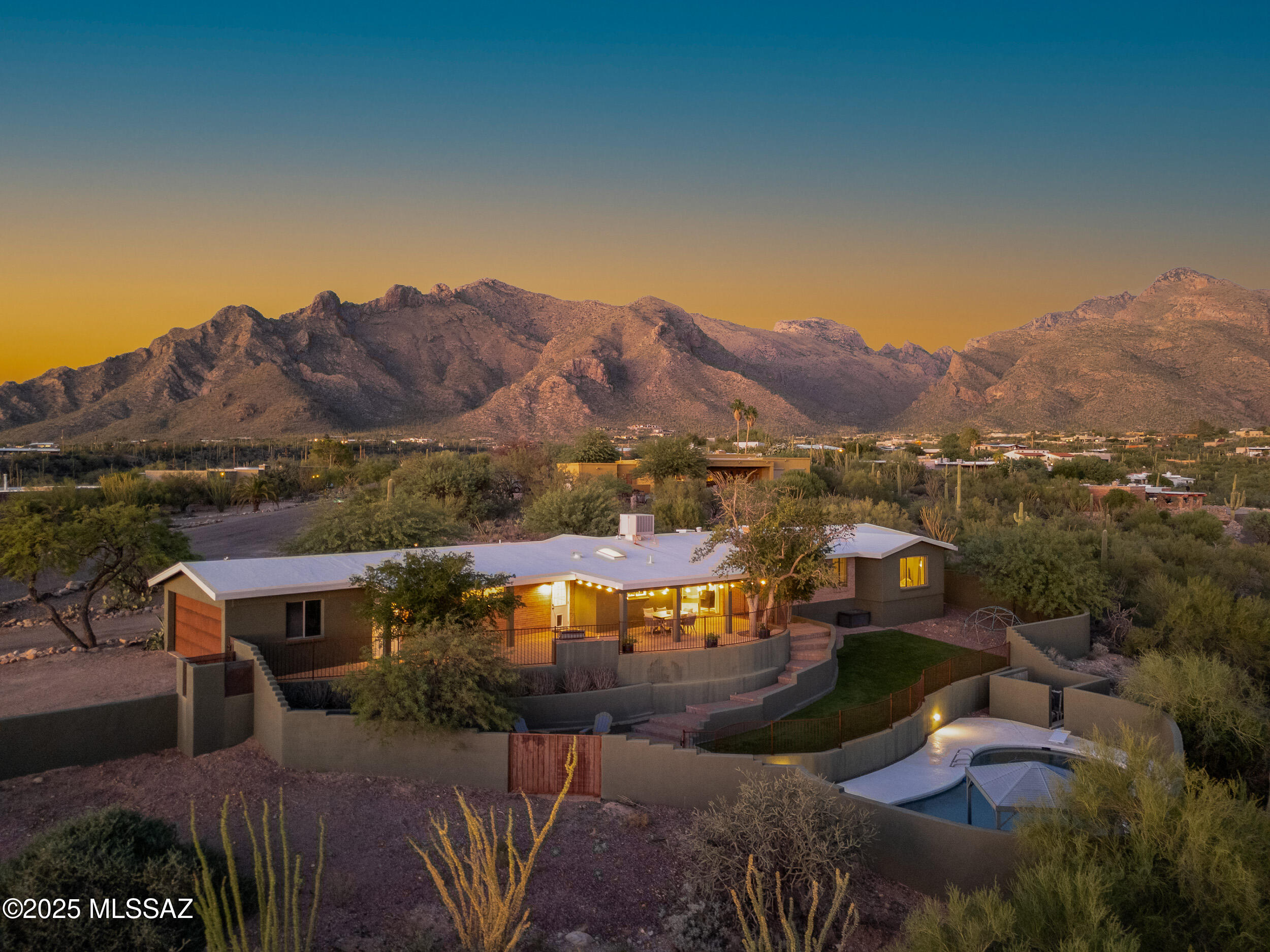 Perched on an elevated 1.29-acre lot with sweeping desertscape, mountain and twinkling city lights views, this ranch-style brick home offers single-level living with no interior steps and an airy, light-filled ambiance. The 2,733-square-foot plan includes four bedrooms (dual primaries and two guest bedrooms), three baths and open living spaces. Two open but delineated living spaces (one with a fireplace) are complemented by an adjacent dining room and offer desert vistas through the windows. The open kitchen has classy, creamy white granite counters with soft veining, white cabinetry complete with a charming plate rack and a full stainless appliance package. Just off the kitchen, a practical laundry closet and a mudroom with storage keep daily life running smoothly. The main primary suite is a true retreat generous in scale with a dramatic high ceiling and broad windows that capture mountains by day and city lights by night. Its new spa-like bath features a large walk-in shower clad in marble-look tile with a hexagon basketweave floor, a freestanding vessel tub, and a dual-sink vanity. Two closets include a large walk-in with a barn door, and dual mini-split units allow tailored climate control. The second primary suite, ideal for guests or multi-generational living, sits privately at the opposite end of the home and offers a vaulted ceiling, dual vanities, a walk-in shower with a separate makeup/vanity counter, a lockable walk-in closet, and an additional linen closet. Two additional comfortable guest bedrooms share a full hall bath. Out front, a minimalist desert-landscaped courtyard sets a serene tone. There is plenty of parking/driveway space and an attached two-car garage. The private backyard unfolds across multiple terraced levels designed for effortless entertaining and everyday enjoyment. The upper level, accessed by sliding doors and enclosed by a view fence, provides a covered paver patio and an extended terrace with flagstone-topped banquette seating and a built-in barbecue. The middle terrace offers broad stretches of low-maintenance faux grass, a firepit gathering area, and a versatile gravel area ready for a play structure or garden. At the lowest level, the pool area (with a diving board and shaded pergola) invites leisurely afternoons and sunset swims. The location places the best of North Tucson within easy reach  approximately four minutes to La Encantada, five minutes to Whole Foods and favorite dining spots such as Wildflower, Truland, Teaspoon, and El Charro Steakhouse, seven minutes to Tohono Chul, and ten minutes to Trader Joe's. Don't miss seeing this wonderfully livable home with a very welcoming vibe!