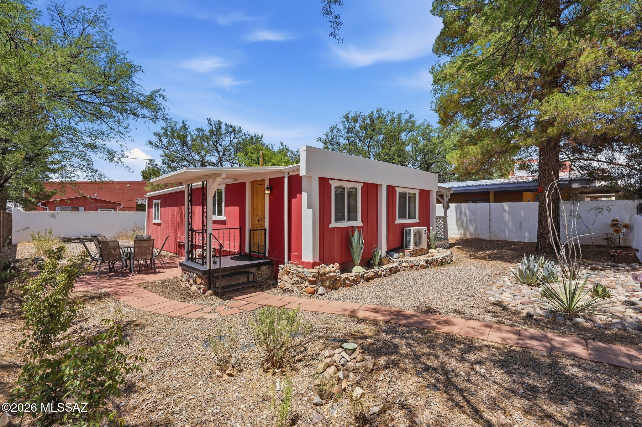 Welcome to the Little Red Cabin, located in the center of Patagonia just steps away from the town's restaurants, gifts shops, and markets! This home is central to all that this beautiful nature haven has to offer, such as the Arizona Trail, Patagonia Lake State Park, the Nature Conservancy, and the Patton Center for Hummingbirds, and is located just 25 minutes to Nogales and an hour to Tucson. This lovingly cared for 2-bedroom, 1-bath home boasts a beautiful yard with a privacy wall surrounding all sides, a large, covered deck running the full length of the house on the east side, an outdoor patio on the west side, and a beautiful shade tree in the front yard. The kitchen has a newer stainless-steel refrigerator and a 5-burner stainless gas stove. The current owners have updated the home to create an open concept between the kitchen and living room. The living room is filled with wonderful sitting areas and has plenty of room for a great workspace in front of a picture window overlooking the patio. The main bedroom is large, with a king-size bed and plenty of closet and storage space; the second bedroom haa served as a music and art room with a futon that converts into a full bed for any guests you may have. The living room has a newer 2-ton mini-split heat/air conditioning unit, and each bedroom has a dedicated a/c unit, keeping the home cool and comfortable.
The backyard has a separate shed with full washer, dryer, and utility sink, plus extra storage space with a gardening bench. The recently added corrugated metal wall adds character and increased privacy. Recently installed restorative landscaping features rainwater catchment systems and basins, a grey water diversion valve from the laundry, and native desert plantings including a beautiful rock and succulent garden in the front yard. Enjoy the magnificent butterflies and hummingbirds that now frequent the yard! The home is centrally located in this vibrant town, steps away from the library and town park, and close to the school and community pool. Ideal for full time living, rental, or vacation rental income. If you want to enjoy a private setting while also being right in the heart of the village, you will love the quaint and beautiful Little Red Cabin!
