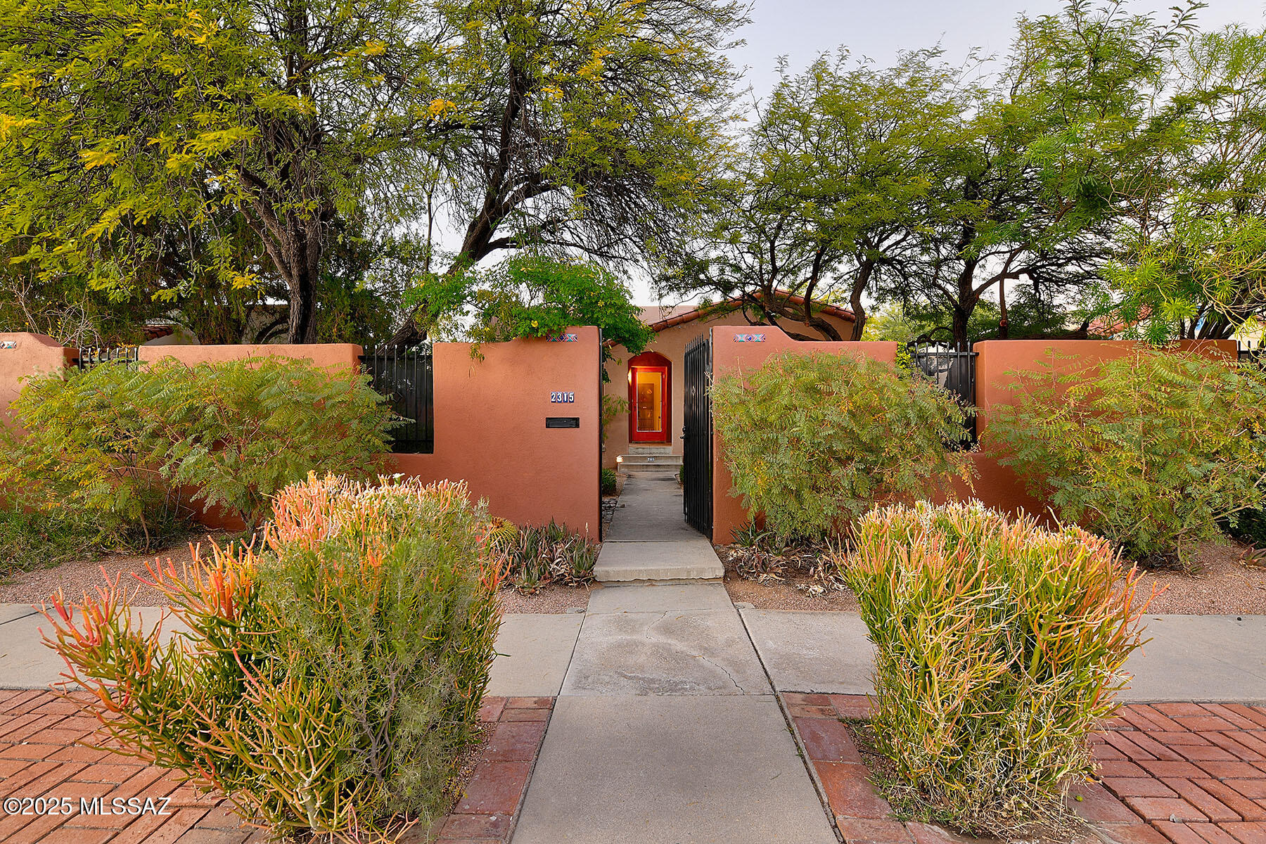 Sam Hughes 1937 Spanish/Moorish Bungalow. This beautiful 2-bedroom, 2-bath home blends timeless character with thoughtful modern updates. Features include original restored hardwood floors, a wood-burning fireplace, large windows, living room & formal dining room. The well-appointed, remodeled cook's kitchen offers ample storage, granite countertops, and stainless steel appliances. A butler's pantry includes a convenient laundry area & extra storage. The spacious primary bedroom boasts and ensuite bath with double vanities, a walk-in closet, and a large walk-in shower. Additional spaces include a den/office and a second full bathroom. Stunning mature mesquite trees create a lush canopy over the walled, private grounds. A separate workshop/storage room adds versatility, and a rare 4-car carport is accessible from the alley. Walking distance to The U of A., the ModerStreet car, Himmel Park, Restaurants and more!