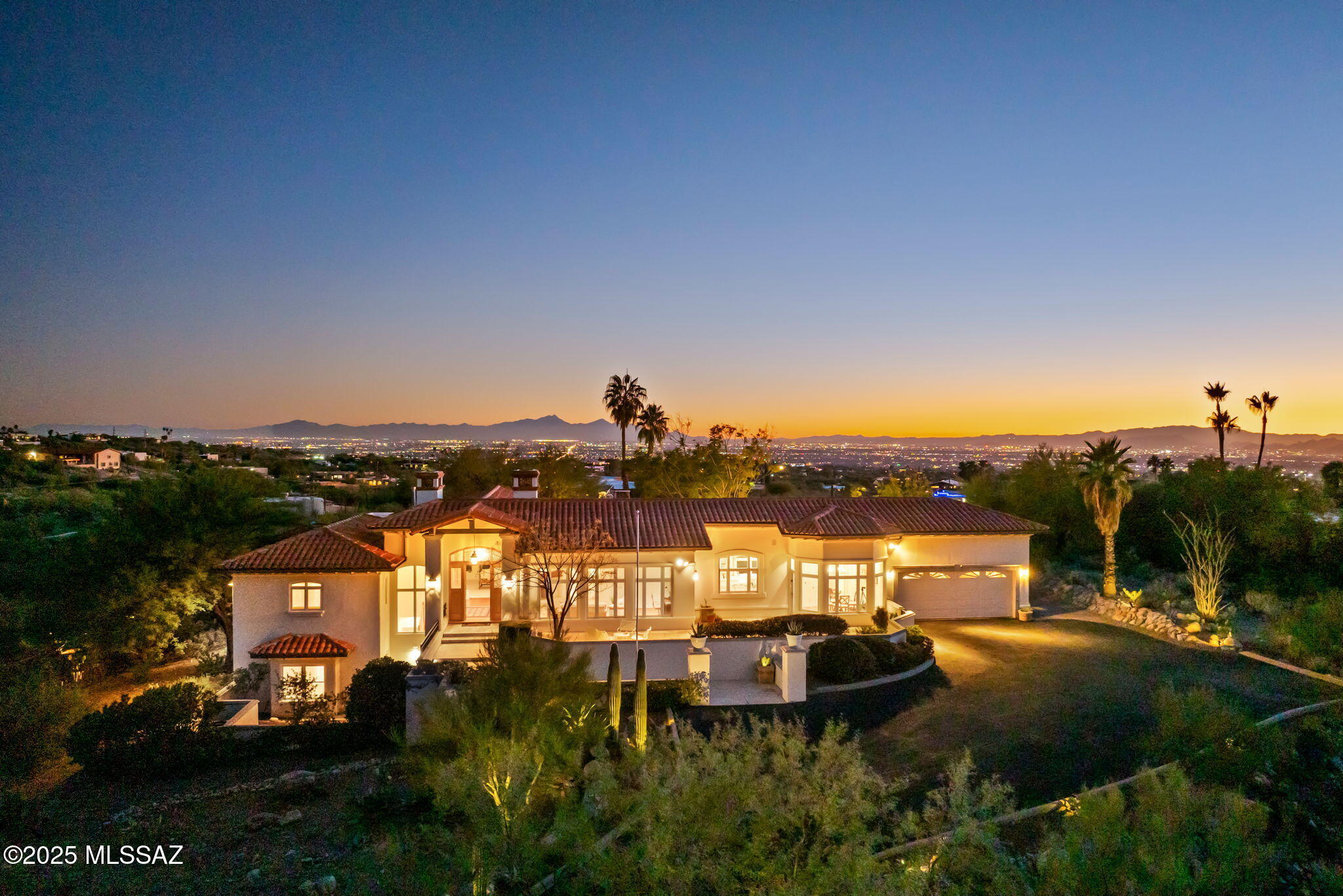 For the First Time Ever Offered for Sale- The Ballmer Estate in prestigious Skyline Country Club Estates! Born in Europe, refined in California, and shaped by a life well lived across some of the world's most extraordinary locations, the original owner of this residence possessed an intuitive sense of design and a vision far ahead of her time. On one of Skyline's premier hilltop parcels, she created her dream home—now known as The Ballmer Estate—and entrusted architect Bill Gansline to bring it to life. The result is a masterwork of refined, understated luxury designed for effortless entertaining and casual daily life. Positioned on a rare elevated hill-top lot, the home delivers commanding views in every direction—dramatic Catalina Mountain vistas from the front and sweeping, twinkling city lights from the rear captured through expansive walls of glass. The main level features a flawless, highly functional floorplan. Upon entering, white-washed beamed ceilings, rich wood floors, and floor-to-ceiling picture windows establish an immediate sense of calm and refined elegance. A custom wall of built-ins and a gas fireplace anchor the living room, while French doors open onto the grand covered terrace. Adjacent you will find an exceptional dining room with coffered ceilings and panoramic city and garden views. The gourmet kitchen is bright, spacious, and genuinely inspiring, even for those who rarely cook, offering abundant storage, a large center island with gas cooktop, double ovens, Sub-Zero refrigerator/freezer, a walk-in pantry, extensive prep space, and a breakfast nook framed by floor-to-ceiling windows and a private patio for morning coffee with the towering Catalina Mountains above. A warm, inviting family room adjoins the kitchen, complete with a gas fireplace, custom millwork, oak floors, and an ideal workspace for the at home professional or just paying the bills. The primary suite is a private sanctuary with city-light views, its own patio, dual walk-in closets, and a spa-like bathroom with steam shower and soaking tub. On the lower level, guests will feel truly spoiled. Two generously sized bedrooms share a Jack-and-Jill bath and enjoy a private patio with striking mountain views and their own separate entrance. A large bonus room currently used as a wine cellar and storage could serve as a man cave, studio, mother-in-law suite or a large safe room. 
Outdoor living is exceptional in every way. All main rooms in the house open to the expansive covered terrace overlooking the twinkling city lights below and the sparkling pool and spa area. Off the kitchen is a covered grill area for the few days a year you might get wet grilling outside here.  Mature landscaping, peaceful fountains, and unmatched views complete a setting that feels both timeless and magical and instantly transports you to Santa Barbara or the Amalfi coast. The oversized workshop and adjacent storage room off the garage present a straightforward opportunity to create an attached guest casita with private entrance and side parking-easily converting this into a 4-bedroom, 4-bathroom home without disrupting the existing floorplan. Perfect as a primary residence or a low-maintenance lock-and-leave retreat, the home benefits from Skyline Country Club's 24/7 manned gate and active patrol, providing added peace of mind. Lovingly maintained by its original owner until the age of 98, this residence stands as a rare fusion of European design & class, California casual elegance, and desert Southwest architecture & influence decades ahead of its time and only improving with age.