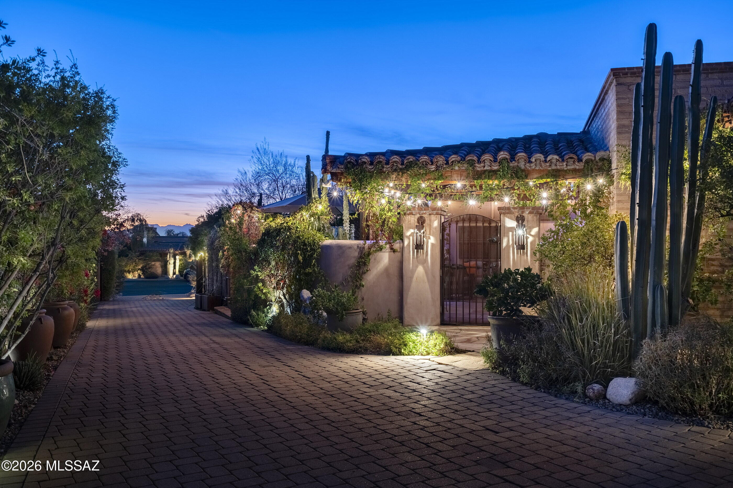 Conceived as an intimate dialogue between land, craft, and time, this authentic mud adobe residence is a quiet manifesto of place. Designed and built by James Gray of Stellar Gray Fine Homes, the home rests behind private gates within Adobes De La Vista, a rare enclave of 7 Adobe residences set in the heart of the Catalina Foothills. At 2,639 square feet with 3 bedrooms and 3 baths, the property unfolds as a composed sequence of spaces where architecture feels shaped rather than imposed, emerging naturally from the desert floor. The walls, formed from 16 inch thick stabilized mud adobe, give the home its unmistakable presence and deep sense of permanence. Their mass tempers light and heat, creating interiors that feel calm, grounded, and protective. Plaster surfaces soften the geometry, while stone walls built from rocks gathered on site root the architecture firmly in its surroundings. Antique columns sourced from India introduce a subtle global patina, standing as quiet witnesses to centuries of craftsmanship and lending the home a sense of lived history.

At the heart of the residence, the great room gathers living room, dining room, and kitchen into a single, fluid volume. This space feels generous yet restrained, where proportion and material guide the experience rather than ornament. Knotty alder cabinetry brings warmth and texture to the kitchen, its natural grain echoing the organic character of the adobe walls and concrete countertops, providing tactile surfaces reinforcing the honesty of the architecture. Light moves gently across the room throughout the day, reinforcing the feeling that time itself is an essential design element.

To the north, the great room opens seamlessly into a sunroom that acts as a luminous threshold between inside and out. Beyond, the north patio reveals an atmosphere reminiscent of San Miguel De Allende - intimate, layered, and quietly celebratory. Here, the architecture encourages pause and reflection, with framed views and shaded edges that invite long afternoons and unhurried evenings.

The south facing front courtyard offers a contrasting yet complementary experience. A covered veranda defines the space, creating a sheltered outdoor room that opens directly onto a built-in therapeutic spa. This courtyard serves as both arrival and retreat, a place where water, shade, and adobe walls converge to create a deeply personal sanctuary. Gardens weave throughout the property, offering paths to meander and moments of discovery, reinforcing the idea that this home is not simply occupied, but experienced.

Completing the narrative is an owned EnPhase solar system that works in quiet harmony with the thermal mass of the adobe construction. The thick earthen walls naturally moderate interior temperatures, absorbing warmth during the day and releasing it slowly as evening falls, while solar energy supports efficient and sustainable living. Together, these elements create a residence that feels timeless yet forward thinking, where comfort, responsibility, and beauty exist in effortless balance.