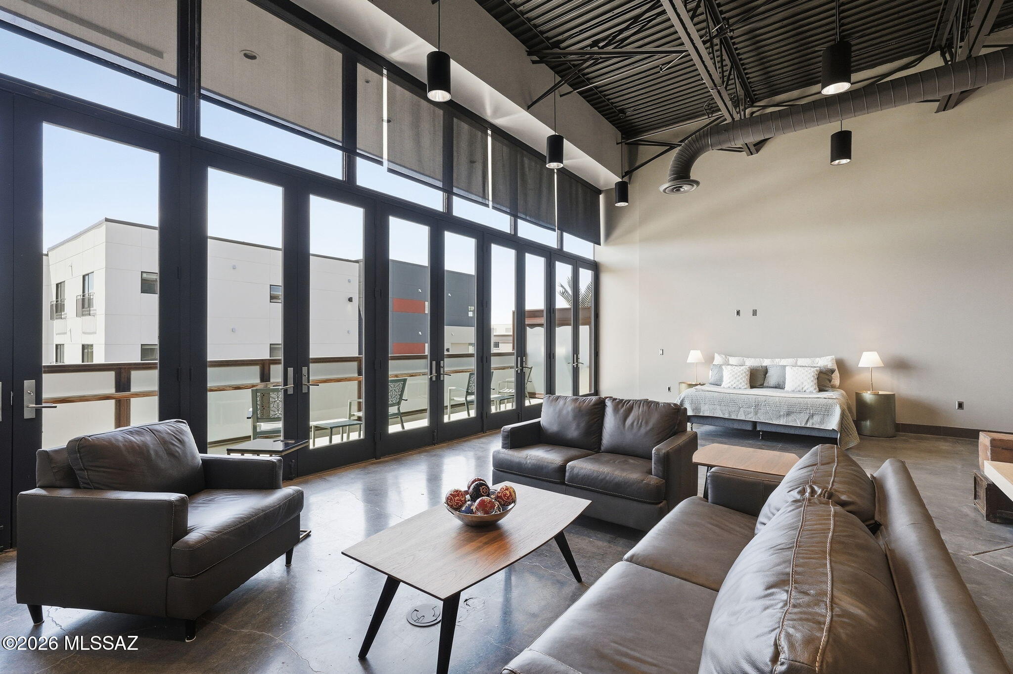 Seize a rare opportunity to own a gorgeous modern loft in desirable downtown Tucson. This distinctive residence blends contemporary sophistication with industrial refinement, featuring open-truss double-height ceilings and polished concrete floors. The architecture and open concept design make the space feel grand and expansive. 
Floor-to-ceiling windows bathe the open-concept layout in natural light, leading to a custom gourmet kitchen.  Defined by rift-sawn white oak cabinetry and professional-grade appliances, this thoughtfully designed space is perfect for culinary enthusiasts who appreciate both form and function. Beyond the versatile mezzanine level, a massive 30-foot private balcony offers front-row views of the Santa Rita Mountains, Armory Park, and ''A'' Mountain. Complete with restricted elevator access and a secure,
