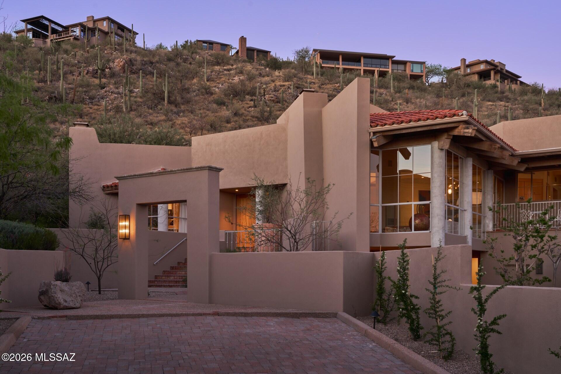 A thoughtfully reimagined residence by designer Casey W. Smith, this bold architectural home is set into the hillside and defined by material, light, and a sense of casual grandness. Brick floors add warmth and texture, while soaring steel-framed windows draw the landscape inward, filling the interiors with natural light. Warm wood tones create continuity throughout.

The home unfolds through an intuitive sequence of spaces designed for gathering and connection, balanced by more intimate moments — a moody powder room, discreet bar, and a skylit library — allowing the residence to shift seamlessly between entertaining and quiet retreat. Natural stone, raw brass accents, and artisan plaster fireplaces lend confident sophistication, while generous ceiling heights enhance scale and presence.

Completely renovated with systems, appliances, fixtures, and finishes thoughtfully upgraded, the home delivers modern performance while honoring the integrity of the architecture. Terraces, courtyards, garden rooms, and the pool extend daily living outdoors, reinforcing a seamless indoor-outdoor relationship. A four-car garage and a flexible layout support multigenerational living, anchored by an expansive primary suite, three additional ensuite bedrooms, and a separate pool suite with spa bath and kitchenette  ideal for guests or extended stays.

Balancing contemporary restraint with classical elegance, this is a perfectly livable home  bold, warm, and entirely its own  set within one of Tucson's most coveted guard-gated communities in the Catalina Foothills, Ventana Canyon Estates. Situated at the quiet, private end of Ventana Canyon Drive.

Nestled in the prestigious Catalina Foothills, residents enjoy proximity to world-class golf, hiking in Sabino Canyon, top rated schools, luxury shopping and dining  all just minutes away.