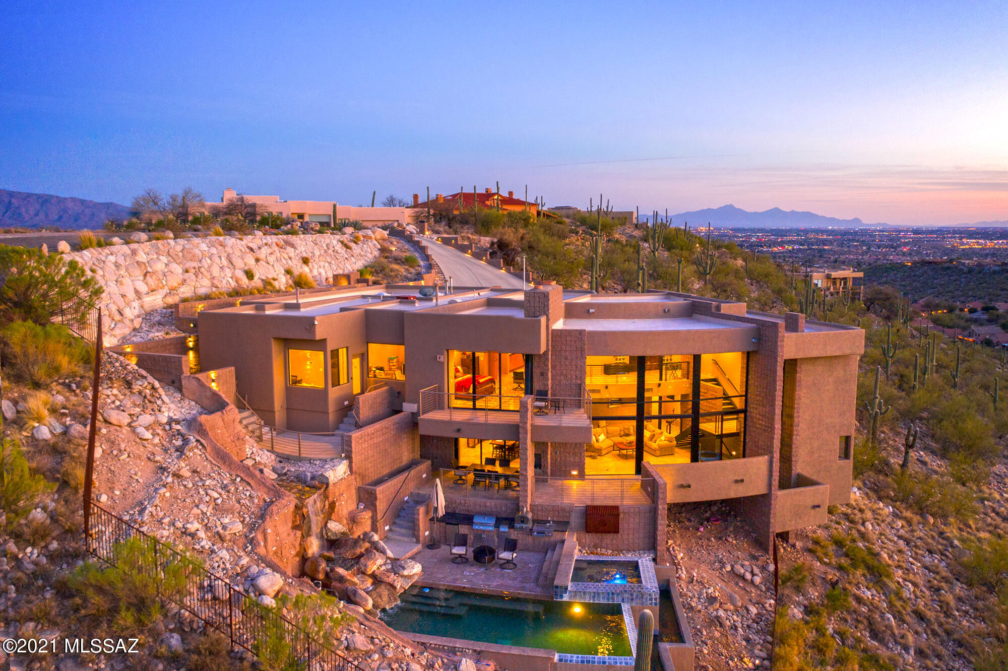 Hill Top Modern Architecture In North Tucson Foothills, a timeless contemporary situated on a lofty hillside, maximizes elevated and panoramic city and majestic mountain from every window; surrounding mountain views by day and mountain silhouettes by night. The most discriminating individual will appreciate the dramatic drive through the private hidden gated community. The utilization of outdoor spaces begins with the dramatic drive toward home, split-faced concrete architecture, cantilevered overhangs, and verandas. As you walk thru the weathered iron entry door you are greeted with a terraced design, floor-ceiling glass with sweeping views, an extraordinary abundance of natural light and magnificent views, yet is warm and comfortable. On the main level is a spacious open great room that provides a massive gathering space; sweeping vista views, over looking the pool and veranda, stone walls and travertine floors through-out, custom cabinetry, solid wood interior doors, modern light fixtures. A streamlined and comprehensive chef's kitchen, dining space, living room with double sided gas rock fireplace, zoom room, office, commercial elevator & guest bath, along with two spacious bedrooms. Built-in security system for main home & casita that features cameras, air temp control, indoor sensors, and garage door controls, all managed from one app. The separate entrance Casita charms every guest with the private patio and unstoppable views. 

A streamlined chef's kitchen, natural wood custom cabinets, granite slab, stainless steel appliances, prep sink in island with raised eat-in bar, adjacent to dining room.

 
The luxury master wing includes gas glass rock fireplace, master bath, walk-in closets, separate office and private view balcony all overlooking the North Tucson Foothills with forever views of 365 dramatic sunsets and city lights. 

This showpiece offers an oversized three-car garage, elevator leads to other levels of home, storage space and mechanical rooms.

 
Multi-leveled patio views from entire house from the floor to ceiling windows with glass doors to the outdoor living space with native cacti, saguaros, wrap-around patio with fire place, boulder waterfall cascading into the pool, sunning patios, outdoor cooking with BBQ, pizza oven, small fridge, and offering unimaginable vistas in every direction. The fanciful LED pool lights change color. The 2-sided negative edge heated Pebble Tec Pool/spa also features jets, lights, music and fun finishes that will make you smile.  A showplace with Tucson seasons: be the first to view rare snow fall, double rainbows, and championship games poolside. Only 3 minute drive to the area's best hiking at Sabino Canyon, fine dining, shopping, and entertainment. Arrange for a private showing, a face-time tour, or visit the video included here.