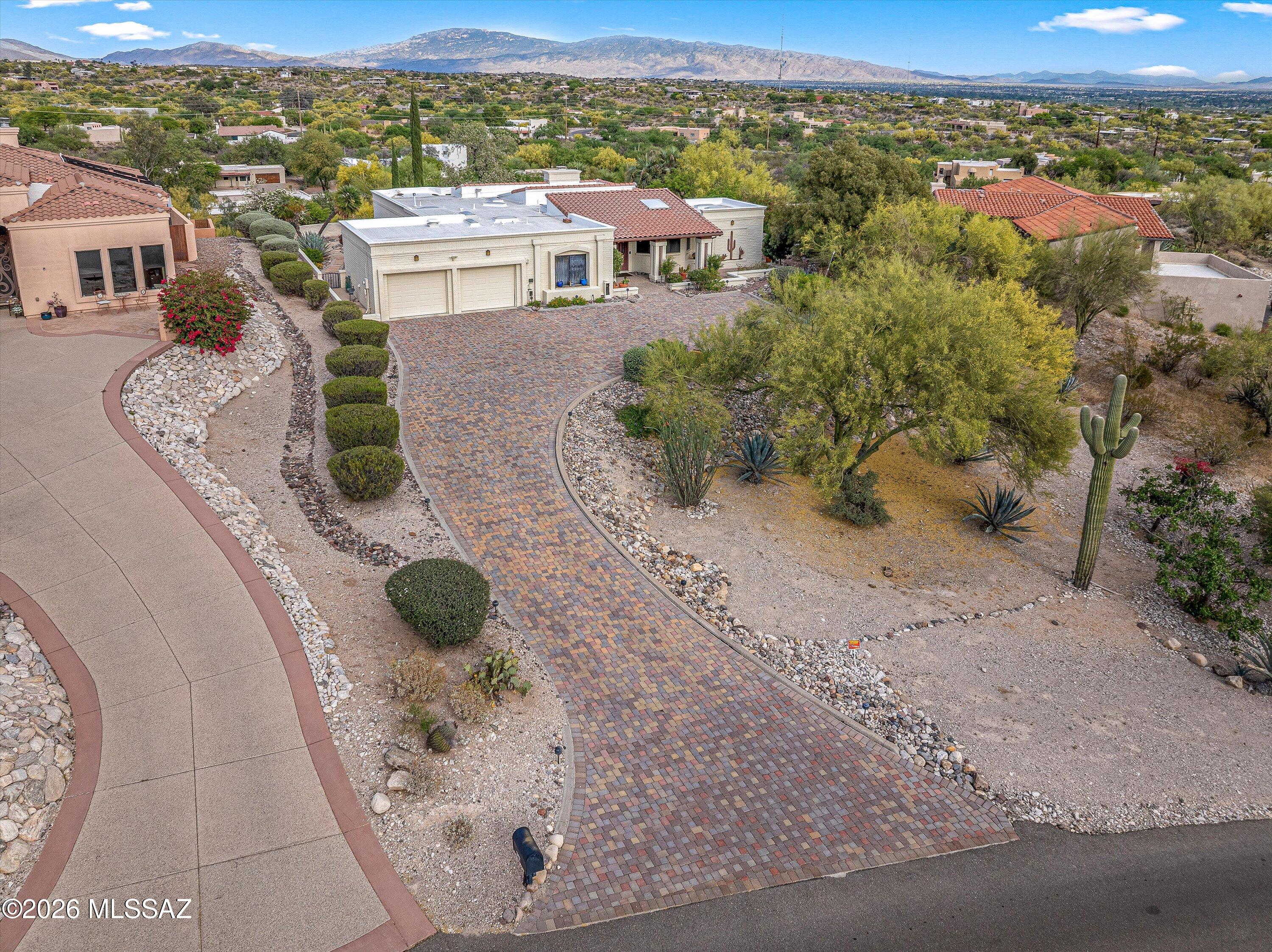 Poised against a breathtaking Catalina Foothills backdrop, this desert sanctuary epitomizes refined Southwestern living. Vaulted ceilings and arched alcoves highlight the spacious home, and expansive skylights bathe it in soft, natural light. A striking hooded fireplace and walls of glass frame the panoramic mountain views. The entertainer's kitchen flows effortlessly to a sprawling enclosed side patio terrace for easy extended entertaining. The enormous primary suite offers an enviable walk-in closet. The connected den/office can be closed off for a private guest room. This house has abundant clever storage, and feels like home the moment you walk in. From the terracotta roof to the lighted xeriscape, every detail celebrates Tucson's serene beauty and effortless indoor-outdoor living.