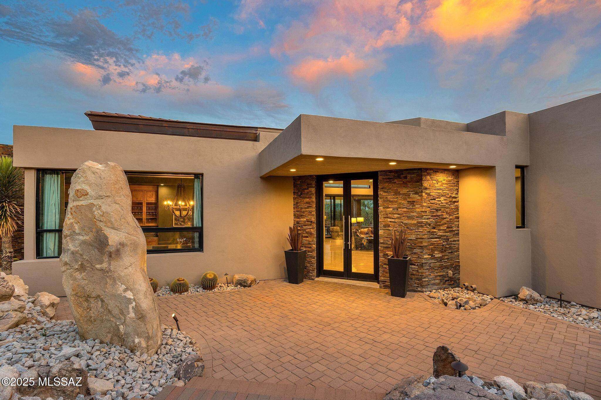 A Modern Desert Space Of Your Own In Stone Canyon | Set alongside the 13th Fairway and seamlessly carved into the ancient rock outcroppings of Stone Canyon, this contemporary residence is a celebration of design, landscape, and luxury. Surrounded by saguaros and sculptural boulders, the home offers a blend of serenity, privacy, and panoramic views. Daylight brings sweeping vistas of the Catalina Mountains, while nightfall reveals the city lights of Tucson. The home is being offered fully furnished with pieces from Restoration Hardware, Arhaus, American Leather, and LCM custom designs, allowing for a seamless transition into luxury living. Mechanical systems have been recently replaced, ensuring peace of mind and comfort. Inside, you'll find an expansive great room designed for effortless entertaining and daily living. Tall ceilings, walls of glass, and multi-panel sliding doors dissolve the boundaries between indoors and out, allowing the desert to become part of the architecture.
The spacious gourmet kitchen is a wonderful space to cook and gather which features dual islands, Wolf and Sub Zero appliances, and breakfast room with mountain views. An elegant dining room framed by large picture windows creates a dramatic yet intimate setting with views and privacy.

Designed for both grand entertaining and quiet moments, the home features multiple outdoor living areas. A sprawling covered patio includes a full outdoor kitchen and fireplace, while an infinity-edge pool and spa stretch out toward the desert horizon. The rooftop deck with glass walls to preserve every view around you, complete with its own fireplace, invites you to take in the stars and city lights. The flagstone path leads to a bocce court and a secluded viewing patio raised high on the hill  an ideal setting for morning coffee or evening cocktails, surrounded by the breathtaking beauty of downtown Tucson, the Santa Catalina Mountains, and Arizona's vibrant sunsets.

With its blend of timeless elegance, modern design, and unparalleled views, this desert sanctuary is a rare and remarkable offering in one of Southern Arizona's most prestigious communities. Note: Small list of furniture/art pieces to be excluded.