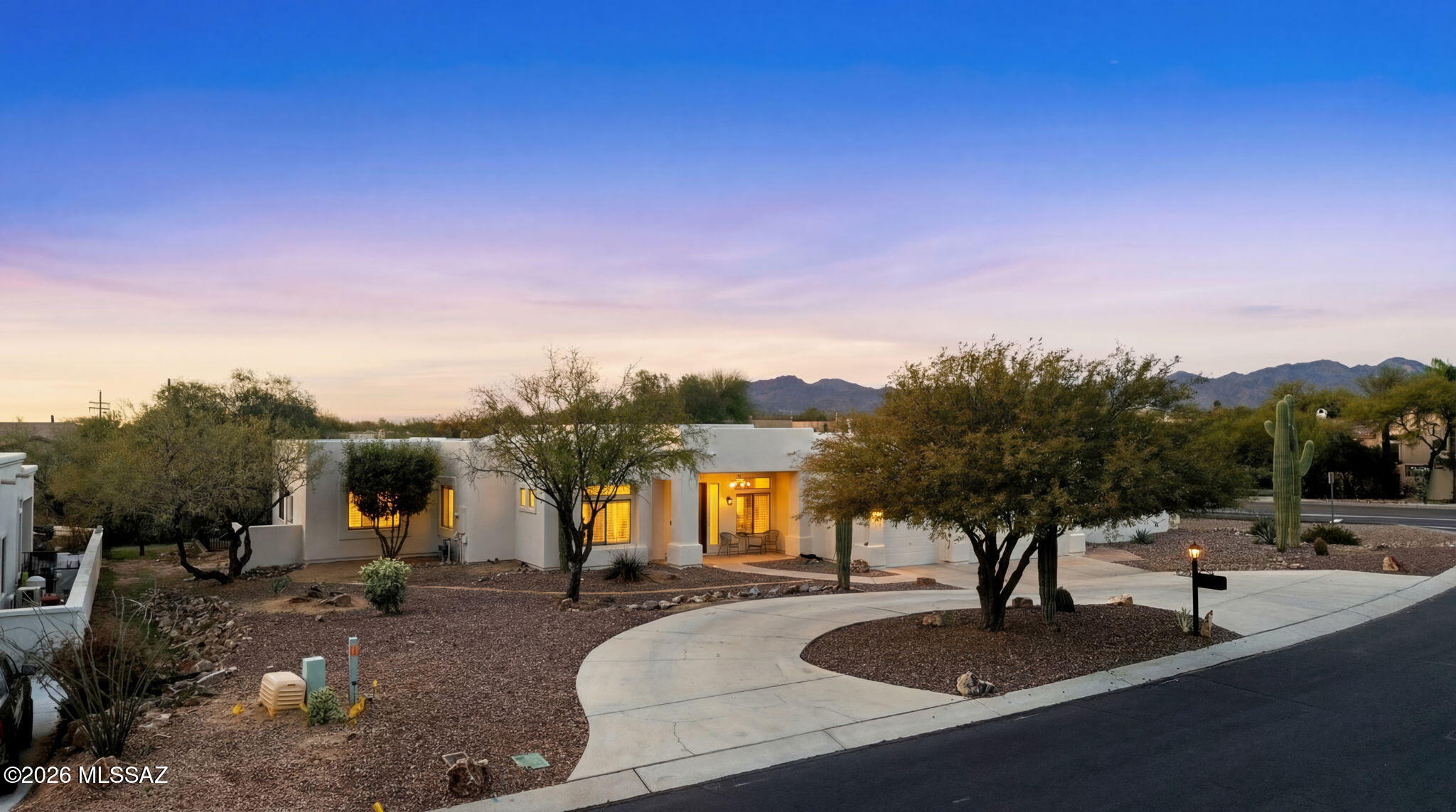 Nestled in the heart of Oro Valley's scenic desert landscape, this beautifully maintained single-story residence offers a seamless blend of modern comfort and Southwestern charm. Set on a spacious lot with mature desert landscaping, this home provides both privacy and breathtaking mountain views.
A long, gently curved driveway leads to an inviting contemporary stucco façade with a three-car garage and a welcoming front entry. Inside, the open and airy floor plan features soaring ceilings, warm wood flooring, and abundant natural light throughout. The spacious great room flows effortlessly into the chef's kitchen, which boasts white cabinetry, granite countertops, a large center island, stainless steel appliances, and ample storage—perfect for both everyday living and entertaining.