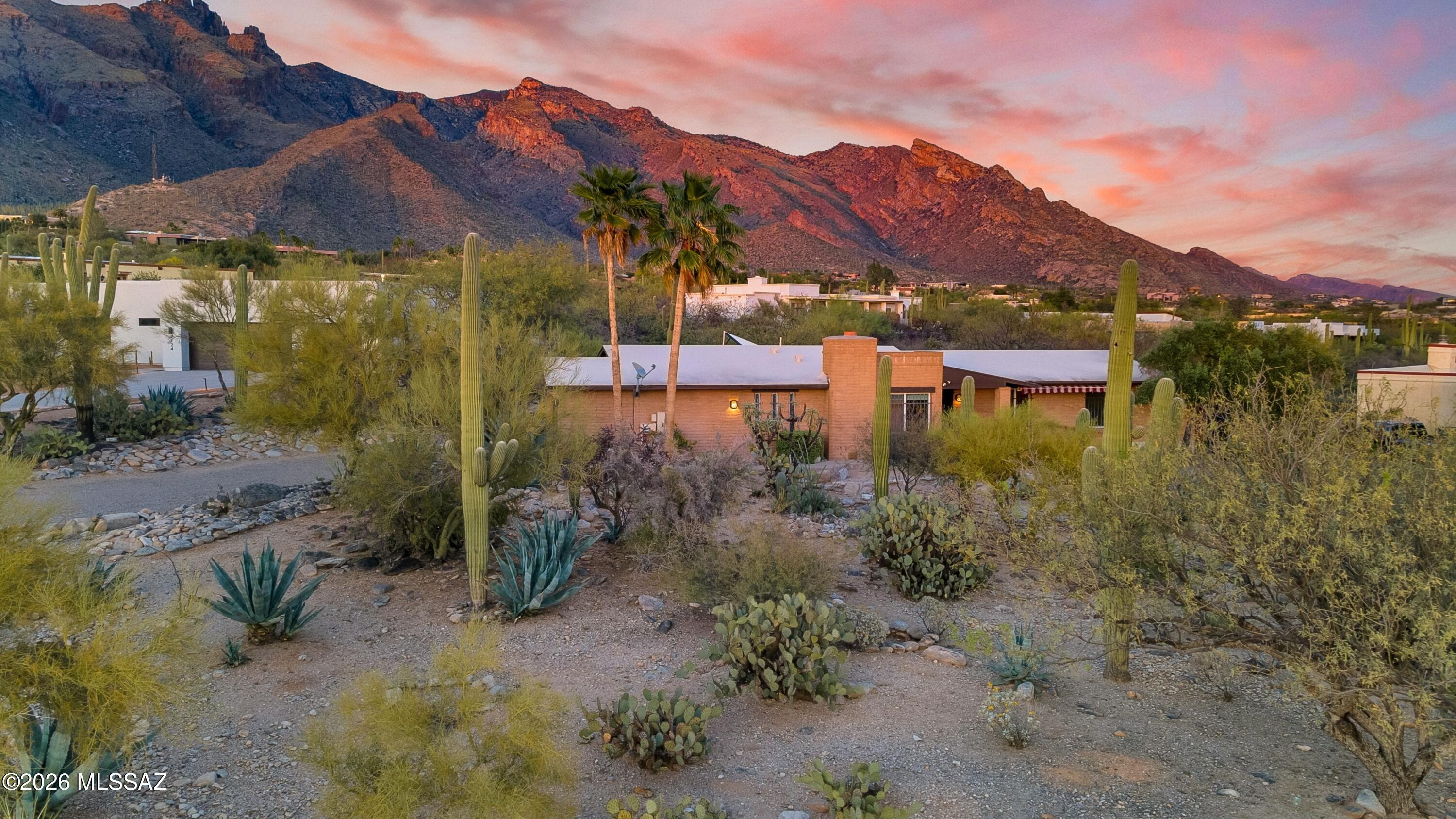 Set high in the Catalina Foothills near the crest of Campbell Avenue, just moments north of La Encantada, this thoughtfully expanded residence captures sweeping city lights and dramatic mountain views from an elevated, over ¾-acre homesite. With permitted additions enhancing both livability and flow, the home offers a rare combination of privacy, efficiency, and move-in-ready comfort, featuring a newer HVAC system, solar water heating, and a recently recoated roof. The updated kitchen is both functional and refined, appointed with rich cherry cabinetry with rollout shelving, granite countertops, and upgraded appliances including an induction cooktop. It opens seamlessly to a generous dining area and an expansive living room, where an electric fireplace creates a warm focal point(continued against a backdrop of glittering Tucson city views. The primary suite is a true retreat, oriented to capture both Catalina Mountain and city vistas. The spa-inspired bath features dual vanities, a spacious walk-in closet, and a walk-in shower framed by picture windows that elevate everyday routines into a scenic experience. A well-positioned guest bedroom enjoys easy access to a full hall bath, while the privately situated third bedroom functions as a secondary suite, complete with its own ensuite bath, ample closet space, and direct access to a charming sunroom, ideal as a light-filled studio, lounge, or "catio," all with stunning mountain views. A pantry/laundry room just off the kitchen provides additional storage and utility, leading to a full-size two-car garage. Outdoors, natural desert landscaping in both the front and rear yards creates a low-maintenance environment that complements the surrounding Sonoran landscape. Ideally located near premier hiking trails, upscale shopping, and dining, this property offers the perfect balance of serenity and convenience, equally suited as a full-time residence or an elegant seasonal retreat.