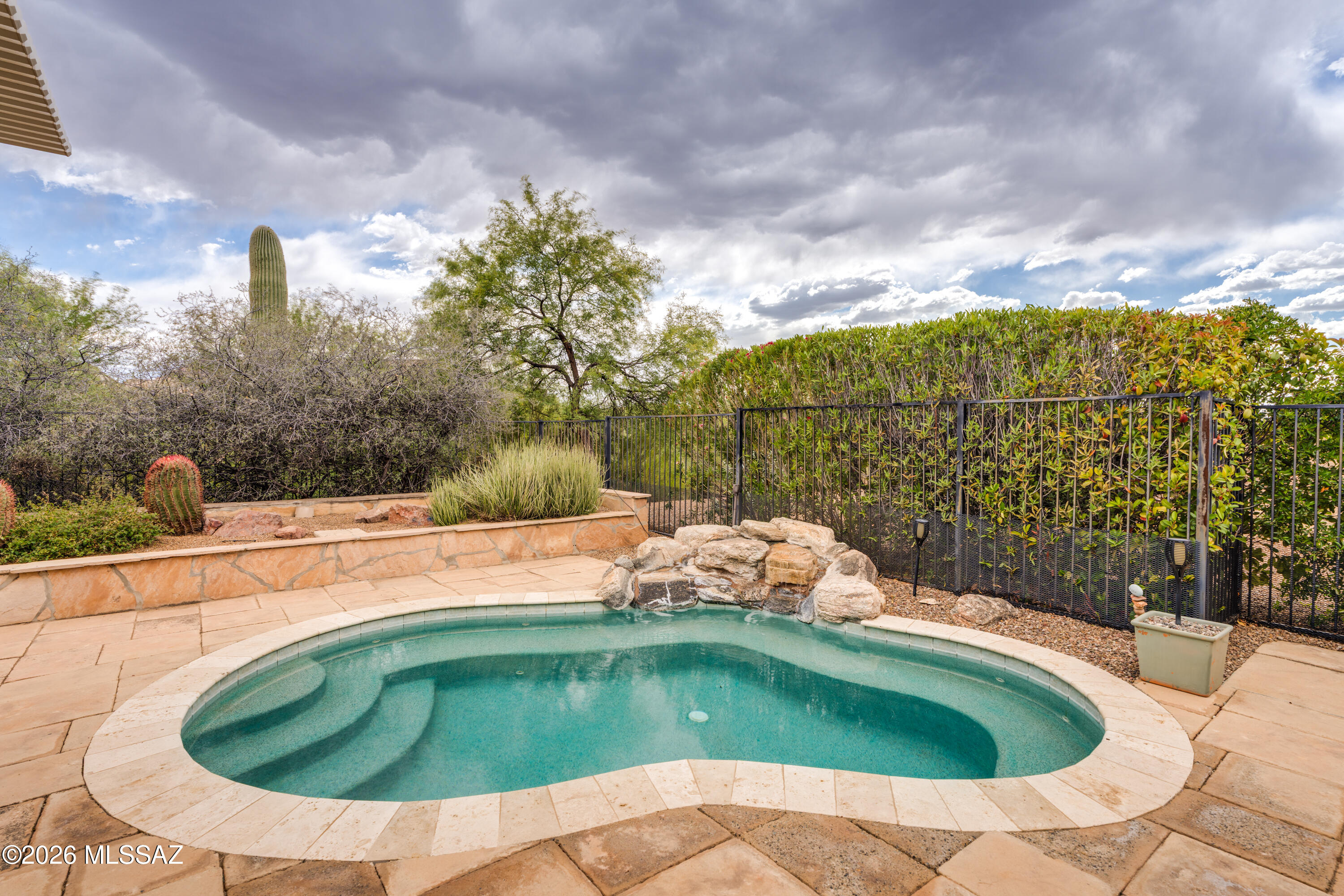 Situated on a premium homesite backing to lush common area, this 1,589 sq.ft. Oakmont model in Quail Creek features a spacious backyard retreat designed for year-round Arizona outdoor living, complete with a refreshing spool and tranquil waterfall feature. This home offers 2 BR, 2 BA, and a versatile den ideal as a formal dining room, home office, or hobby space. A welcoming front paver courtyard leads to the entry foyer and into a spacious great room designed for comfortable everyday living and entertaining. Hard-surface flooring extends throughout the living areas, while both bedrooms feature new carpet for added comfort. The upgraded kitchen showcases granite countertops, pot drawers, pantry closet, electric range, dining nook, and a built-in buffet providing additional storage and serving space. The extended owner's suite features a bay window overlooking the spool and includes a well-appointed bath with dual vanity, tile shower, and walk-in closet with custom built-ins. A split bedroom plan offers privacy for guests, with the guest bedroom featuring a built-in armoire and adjacent bath with tub/shower combination. The backyard is designed for relaxed resort-style living with an extended paver patio, oversized pergola, and the versatile spool and tranquil waterfall feature combine the best elements of a spa and pool. Ideal for cooling off on warm Arizona days, enjoying soothing hydrotherapy, or simply unwinding outdoors, this inviting space is perfectly suited for both quiet relaxation and entertaining family and friends.
